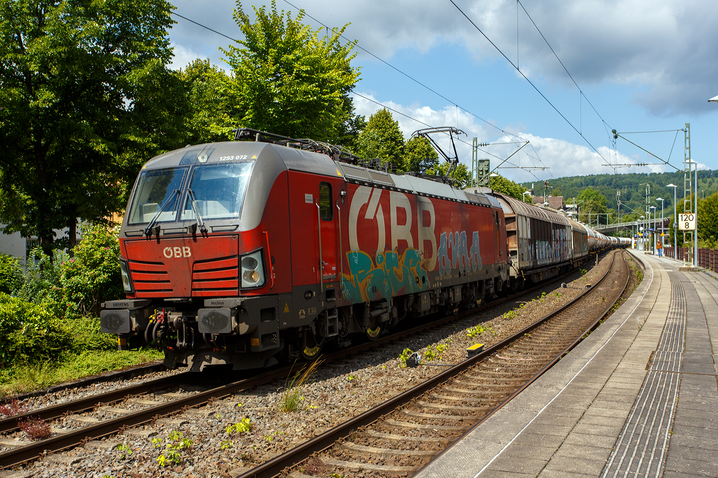Die leider beschmierte ÖBB 1293 072 (91 81 1293 072-5 A-ÖBB), eine Siemens Vectron MS (X4E) in der Variante A35-1a (Länderpaket) der ÖBB-Produktion GmbH, fährt am 17 Juli 2025 mit einem sehr langen gemischten Güterzug durch den Bahnhof Kirchen (Sieg) in Richtung Köln.

Die SIEMENS Vectron MS / X4E wurde 2020 von Siemens in München-Allach unter der Fabriknummer 22759 und an die ÖBB - Österreichische Bundesbahnen (ÖBB-Produktion GmbH) geliefert. Sie ist in der Variante A35-1a ausgeführt und hat so die Zulassungen für A, D, I, SLO, CZ, SK, H, PL und HR. Von der Variante A35 hat die ÖBB insgesamt 123 Loks (1293 001-123).

Ende Januar 2017 unterzeichneten die Österreichischen Bundesbahnen und Siemens Mobility einen Rahmenvertrag über bis zu 200 Lokomotiven, wovon die ersten 30 Mehrsystem-Vectron direkt zum Gesamtpreis von 120 Mio. Euro abgerufen wurden.

Die Siemens Vectron weisen im Betrieb mit Wechselspannung eine Leistung von 6.400 kW, mit Gleichspannung 6.000 kW, auf und haben eine Masse von bis zu 90 Tonnen, die auf vier Achsen verteilt eine Achslast von 22,5 Tonnen ergibt. Aufgrund der überwiegenden Verwendung im Güterverkehr sind die Lokomotiven zunächst für 160 km/h zugelassen. Zur Verbesserung der Laufeigenschaften auf kurvenreichen Strecken wurden die Lokomotiven mit aktiven Drehdämpfern ausgerüstet

TECHNISCHE DATEN:
Spurweite: 1.435 mm (Normalspur)
Achsformel: Bo’Bo’
Länge über Puffer: 18.980 mm
Breite (über Handstangen): 3.012 mm
Höhe (Panto abgesenkt): 4.248 mm
Begrenzungslinie: UIC 505-1
Drehzapfenabstand:  9.500 mm
Achsabstand in Drehgestell:  3.000 mm
Raddurchmesser:  1.250 mm (neu) / 1.160 mm (abgenutzt)
Dienstgewicht: 90 t
Max. Radsatzlast: 22,5 t
Meterlast: 4.742 kg
Höchstgeschwindigkeit: 160 km/h  (Lok 1293.047-051 200 km/h)
Antriebsleistung: 6.400 kW (AC) / 6.000 kW (DC)
Anfahrzugkraft: 340 kN
Kleinster bef. Halbmesser: 80 m
Stromsysteme: 15kV/16,7Hz; 25kV/50Hz; 3kV DC (1,5kV DC)
Antriebsart: IGBT Stromrichter und Drehstrom Fahrmotore mit
Antrieb: Ritzelhohlwellenantrieb
Bremsbauart: KE-GPR-E m Z, (D), ep. Dynamisches Bremssystem Elektrodynamische Hochleistungs-Rückspeisebremse, für DC Netze zusätzlich Widerstandsbremse
Leistung der dynamischen Bremse: 6.400 kW (AC) / 6.000 kW (DC), Leistung der Widerstandsbremse: 2.600 kW (DC)
E-Bremskraft der dynamischen Bremse: 150 / 240 kN
Federspeicherbremse 45 / 50: 60 kN
Zugheizung: 900 kVA
Betriebliche Daten:
Zugbeeinflussungssysteme: Alstom IVC ETCS L1-2 + SCMT; LZB 80/E, PZB 90; MIREL VZ1; SHP
Sicherheitsfahrschaltung: Zeit-Zeit Impuls-SiFa
Zugfunk: GSM-R Dual Mesa 23 SW 4.9.3, Analogbetrieb 450 MHz gemäß UIC 751-3, GSM-R gemäß EIRENE FRS 7, SRS 15
Fern- und Vielfachsteuerung: UIC-WTB nach ÖBB Fernsteuerkonzept, ZMS-ZDS-ZWS

Quellen: ÖBB-Produktion GmbH, Siemens und wikipedia
