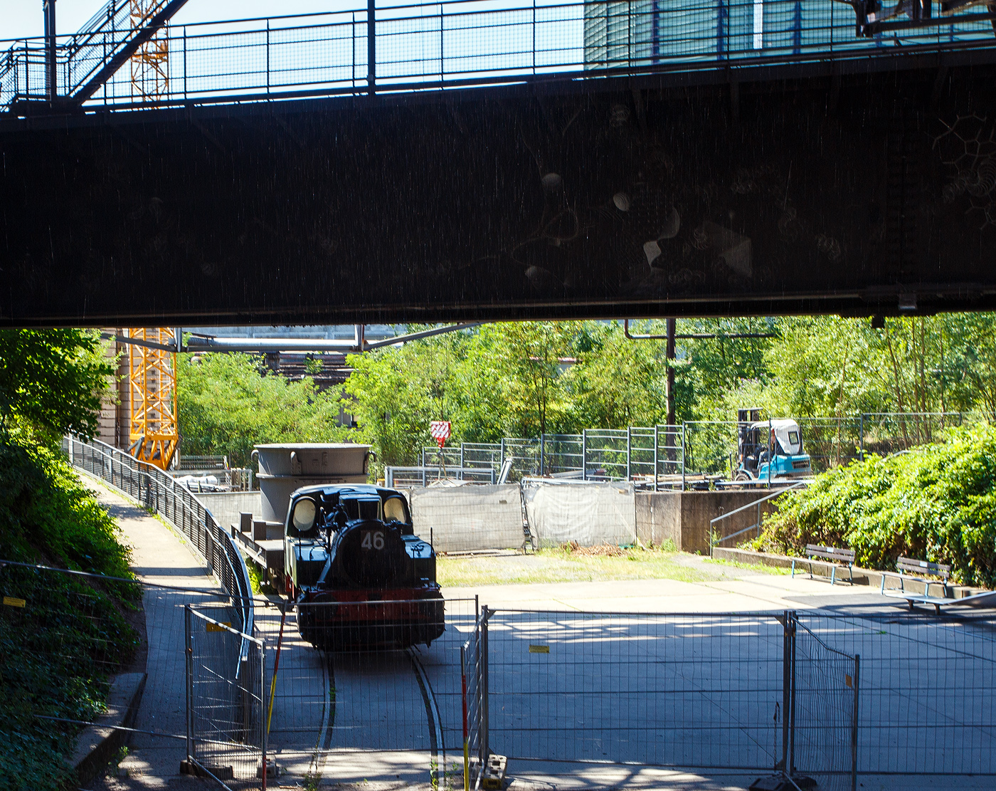 Die Normalspur-Dampflokomotive 46 der V�lklinger H�tte (ehem. R�chling'schen Eisen- und Stahlwerke GmbH in V�lklingen/Saar, ab 1982 ARBED-Saarstahl GmbH, ab 1986 Saarstahl V�lklingen GmbH), eine Jung Hochofenlok niedriger Bauart, abgestellt mit einem offenen Roheisenpfannenwagen der Burbacher H�tte, hier am 01 Juli 2025 am Gel�nde V�lklinger H�tte als Denkmal. Heutiger Eigent�mer ist die Initiative V�lklinger H�tte e.V..

1964 wurde die Lok Nr. 46 mit der Fabriknummer 13835 im Auftrag der R�chling'schen Eisen- und Stahlwerke als letzte rostgefeuerte Dampflok der Firma Arnold Jung, Lokomotivfabrik GmbH, in Jungenthal bei Kirchen an der Sieg gebaut und am 09.12.1964 geliefert. Einsatzgebiet war der Roheisentransport von den sechs Hoch�fen zum Thomasstahlwerk, wobei die besonders beengten Verh�ltnisse auf der V�lklinger H�tte eine besondere Bauform erforderten. Die Verbindung zwischen Eisenwerk und Stahlwerk war nur durch einen Tunnel m�glich, da die Deutsche Bahn durch ihre Gleisanlagen die H�tte in zwei Bereiche teilt. Dieser Tunnel, der Roheisenkanal, ist so niedrig, dass die zweiachsige Lok nur eine H�he von 2.640 mm �ber der Schienenoberkante und eine Breite von 2.450 mm aufweist. Die Loks 44 (11945/Baujahr 1953) und 45 (13240/Baujahr 1959), die nach vorliegenden Unterlagen technisch baugleich sind, wurden schon vorher (von der Arnold Jung GmbH an die V�lklinger H�tte geliefert. 