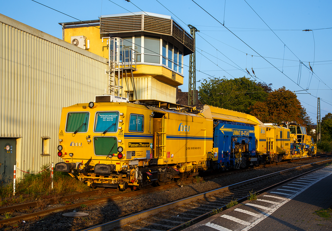 Die Plasser & Theurer Universalstopfmaschine UNIMAT 09-475/4S, Schweres Nebenfahrzeug Nr. D-DGU 99 80 9424 001-2 und die Plasser & Theurer Schnellschotterplaniermaschine SSP 110 SW, Schweres Nebenfahrzeug Nr. 99 80 9425 068-0 D-DGU, sind am 05.09.2021 im Bahnhof Haiger vor dem Stellwerk Fahrdienstleiter (Hf) abgestellt.

Die UNIMAT 09-475/4S eine Kombinierte Gleis- und Weichenstopfmaschine wurde 2011 von Plasser & Theurer unter der Fabriknummer 1358 gebaut und an die DGU geliefert.

TECHNISCHE DATEN der Unimat 09-475/4S:
Spurweite: 1.435 mm
Länge über Puffer: 31.540 mm
Drehzapfenabstände: 6.400 mm / 3.500 mm / 14.000 mm
Achsabstände im Drehgestell: 1.800 mm
Lauf- und Triebraddurchmesser: 920 mm (neu)
Anzahl der Achsen: 8
Gesamtwicht: 122,6 t
Anhängelast: 50 t
Höchstgeschwindigkeit: 100 km/h
Bremse: KE-GP mZ K
kleinster befahrbarer Radius: R 150
zul. Streckenklasse: D4 und höher
zur Mitfahrt zugelassene Personen: 5
