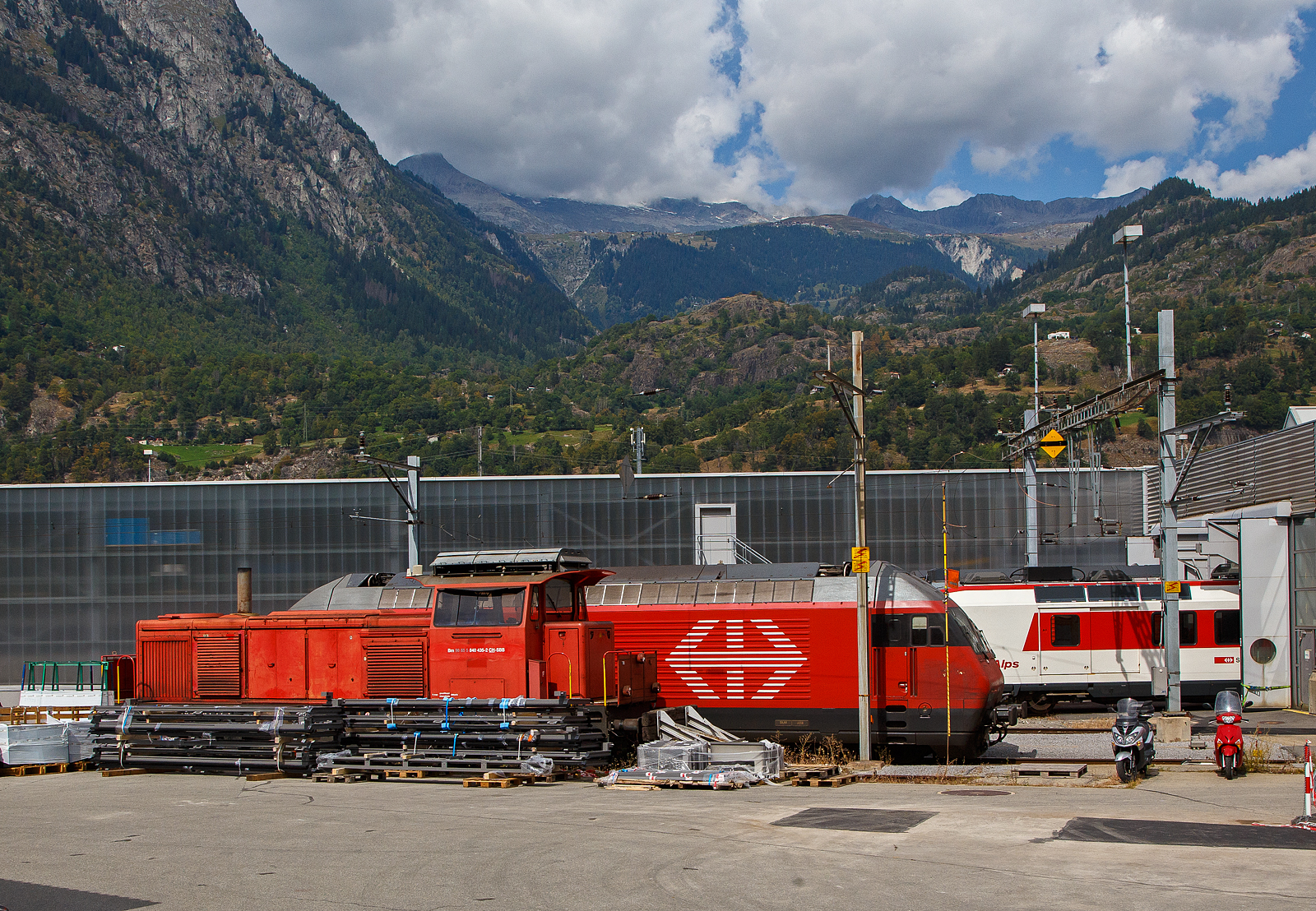 Die SBB Bm 840 435-2 (98 85 5 840 435-2 CH-SBB) der SBB, ex SBB Bm 4/4 18435, leider mit verdecktem Fahrwerk, abgestellt am 07 September 2021 beim SBB Depot in Brig, aufgenommen aus einem MGB-Zug heraus.

Ab und zu trifft man noch auf die SBB Bm 4/4/ SBB Bm 840 eine schwere Rangierlokomotive der Schweizerischen Bundesbahnen SBB. Sie wird/wurde durch die SBB Am 843 von Vossloh abgelöst. Die Normlast der Bm 4/4 beträgt 365 Tonnen bei 15 km/h.

Für den mittelschweren Rangierdienst auf größeren Bahnhöfen beschafften die SBB von 1960-1970 als Ersatz für die letzten Dampflokomotiven die diesel-elektrischen Bm 4/4. Sie bedienten hierbei häufig die nicht elektrifizierten Anschlussgleise und Rangieranlagen. Daneben oblag den Bm 4/4 aber auch die Traktion von LRZ und Hilfswagen bei Entgleisungen und anderen Störungen auf dem Streckennetz. Bei einer Studenleistung von 620 kW erreicht sie eine Streckenhöchstgeschwindigkeit von 75 km/h.

Geschichte:
Die Schweizerische Bundesbahnen (SBB / CFF / FFS) musste sich Mitte der 1950er-Jahre nach neuen Lokomotiven umschauen, um die veralteten, in Betrieb und im Unterhalt teuer gewordenen Dampflokomotiven, bis Mitte der 1960er-Jahre, durch moderne elektrische und thermische Triebfahrzeuge zu ersetzen. Es bestand auch von Seiten des damaligen Eidgenössischen Volkswirtschaftsdepartementes (EVD) und des damaligen Militärdepartementes (EMD) ein Interesse, die fahrdrahtunabhängige Traktionsreserve auszubauen.

So entstanden im Beschaffungsprogramm folgende Typen von thermischen Triebfahrzeugen:
1. Eine schwere Diesellokomotive vom Typ Bm 6/6 für den schweren Rangierdienst in großen Rangierbahnhöfen, zur Führung von Güterzügen auf nicht elektrifizierten Strecken, sowie als Ersatz der Hilfslokomotiven in größeren Depots.
2. Eine mittelschwere Diesellokomotive vom Typ Bm 4/4 geeignet für den mittelschweren Rangierdienst als Ersatz der Dampflokomotiven vom Typ E 4/4 sowie zur Verwendung als Hilfslokomotive in kleineren Lokomotivdepots.
3. Eine Dieselrangierlokomotive vom Typ Em 3/3 für den mittelschweren bis leichten Rangierdienst als Ersatz der Dampflokomotiven vom Typ E 3/3 und E 4/4.

Zusammen mit der Wahl der Diesellokomotivtypen wurde im Sinne einer spezifisch schweizerischen Lösung für alle Lokomotiven die elektrische Leistungsübertragung gewählt. Vorteil war u.a. des Einbaues einer wirksamen
elektrischen Bremse sowie die Kombination des Unterhalts der Diesellokomotiven und der rein elektrischen Triebfahrzeuge.

Aber bereits damals entstanden auch Zweikrafttraktoren welche als elektrische, vom Fahrdraht gespeiste Triebfahrzeuge verkehren konnten und zusätzlich mit einem Dieselmotor für vom Fahrdraht unabhängigen Betrieb ausgerüstet sind. Diese Fahrzeuge, von welchen ein leichter und ein schwerer Typ gebaut wurden, ersetzen leichte Dampflokomotiven und überalterte Benzin und Akkumulatorentraktoren beim Einsatz in nicht voll elektrifizierten Rangieranlagen auf sehr wirtschaftliche Weise.

Die SBB Bm 4/4 (heute Bm 840):
Die 46 Lokomotiven (Bm 4/4 18401-18446) wurden von der Schweizerische Lokomotiv- und Maschinenfabrik (SLM) in Winterthur und der Société Anonyme des Ateliers de Sécheron (SAAS) in Genf gebaut. Sie sollten auch als leichte Streckenlokomotiven zum Einsatz kommen können, um die vollständige Ablösung des Dampfbetriebes zu ermöglichen.

Der Zwölfzylinder-Dieselmotor Typ 12YD20TrTh wurde auch von der SLM selbst gebaut. Er ist mit zwei Abgasturboladern VTR 200 von Brown, Boveri & Cie. (BBC) und einer Ladeluftkühlung ausgerüstet. Der angeflanschte Gleichstromgenerator wurde von SAAS gebaut. Die Baugruppe bestehend aus Motor und Generator wurde auch in der Zweikraftlokomotive Eem 6/6 verwendet. 

TECHNISCHE DATEN:
Gebaute Stückzahl: 46 
Hersteller: SLM, SAAS
Baujahre: 1960–1970
Ausmusterung: 	ab 2006
Spurweite: 1.435 mm
Achsfolge: Bo’Bo’
Länge über Puffer: 12.650 mm (bis 18406) / 13.710 mm (18407 ff)

Drehzapfenabstand: 6.120 mm
Achsabstand im Drehgestell: 2.500 mm
Treibraddurchmesser: 1.040 mm (neu)
Höhe: 4.600 mm
Breite: 3.150 mm
Dienstgewicht: 72 t
Höchstgeschwindigkeit: 75 km/h (geschleppt __ km/h)
Dieselmotor: SLM wassergekühlter V 12-Zylinder wassergekühlter 4-Takt-Dieselmotor mit Abgasturbolader und Ladeluftkühlung, vom Typ SLM 12YD20TrTh
Nennleistung des Dieselmotors: 882 kW (1.200 PS) bei 1.200 U/min
Leerlaufdrehzahl: 400 U/min
Motorhubraum: 90,4 l
Zylinderbohrung /Kolbenhub: Ø 200 mm / 240 mm
Gewicht des Dieselmotors trocken: 10.900 kg
Stundenleistung am Rad: 620 kW (842 PS)
Max. Anfahrzugkraft am Rad: 215 kN (22 t)
Stundenzugkraft am Rad: 127,5 kN (13 t)
Übersetzungsverhältnis: 1:5,93
Anzahl der Fahrmotoren: 4
Leistungsübertragung: Elektrisch
Tankinhalt: 2.000 l
Bremsen: elektrische Widerstandsbremse, pneumatische Bremse, Handspindelbremse

Weitere Technische Beschreibung der Bm 4/4:
Da diese etwas länger ist habe ich sie hier hinten angehangen.

Die Bm 4/4 beschloss das Entwicklungsprogramm der dieselelektrischen Lokomotiven der SBB. Sie berücksichtigte die mit den früher gebauten Diesellokomotiven gemachten Erfahrungen. Die Bm 4/4 stand leitungsmäßig zwischen den Typen Bm 6/6 und Em 3/3. Der von der SLM gebaute mechanische Teil, so vor allem die Drehgestelle, wurden so weitgehend als möglich der Bm 6/6 angeglichen.

Mit Rücksicht auf die zum Teil engen Rangier- und Depotanlagen wurde die Lokomotive sehr gedrängt und kurz gebaut, die ersten sechs waren nur 12,65 m über Puffer lang, die anderen wurden  13,71 m ausgeführt. Damit waren sie trotz der stirnseitigen Plattformen eines der kürzesten Dieselfahrzeuge ihrer Leistungsklasse in Europa. Dank der verhältnismäßig kleinen Maximalgeschwindigkeit von 75 km/h konnte sein Aufbau einfach gestaltet werden. Wie bei den Bm 6/6 wurde auf eine pendelnde Aufhängung des Lokomotivkastens am Drehgestellrahmen verzichtet und ein verhältnismäßig großes abgefedertes Gewicht in Kauf genommen. Pro Drehgestell stützt sich die Lokomotivbrücke über zwei Gummifedern auf die Längsträger des kastenförmig ausgebildeten, geschwelten Drehgestellrahmens ab. Die zwischen den Drehgestellen und der Lokomotivbrücke auftretenden Längskräfte werden durch zwei vertikale, fest mit der Brücke verbundene Drehzapfen übertragen, welche über Gummilager in die Mitteltraverse aus Stahlguss der Drehgestelle eingreifen. Die Übertragung aller Vertikal- und Längskräfte zwischen Lokomotivbrücke und Drehgestellen erfolgt somit über Gummielemente. Die Lokomotive erhält dadurch einen weichen, erschütterungsarmen Gang, und ihre Aufbauten sind gegen den durch Körperschall übertragenen Fahrlärm sehr gut isoliert. Als Achslager kamen die gleichen Kegelrollenlager zur Verwendung wie bei den Bm 6/6. An der Mitteltraverse des Drehgestellrahmens sind ebenfalls in Gummifedern die beiden fremdbelüfteten Tatzlager-Fahrmotoren aufgehängt, welche ihr Drehmoment über je zwei ungefederte, schrägverzahnte Zahnradgetriebe auf die Triebachsen übertragen. Die Forderung nach kurzer Bauweise der Lokomotive führte zur Anordnung des Bremsgestänges auf den Längsseiten der Drehgestellrahmen, wodurch die Unterhalt erfordernden Teile sehr gut zugänglich wurden. Wie bei den Bm 6/6 und Em bestehen die 3/3 Gestängebüchsen aus einem geeigneten Kunststoffprodukt. Die beiden Drehgestelle sind zur Verbesserung des Kurvenlaufes wie bei den modernen elektrischen Drehgestellokomotiven der SBB durch eine Querkupplung verbunden. Zudem ist die Lokomotive mit der von den SBB entwickelten Spurkranz-Oelschmierung ausgerüstet.

Der Lokomotivaufbau setzt sich aus der vollständig geschweißten, als Tragkonstruktion ausgebildeten Lokomotivbrücke, dem mit ihr verschweißten Führerhaus und den beiden Vorbauten zusammen. Zwischen den Drehgestellen sind zwei an der Lokomotivbrücke aufgehängte Dieseltanks von total 2.000 Liter Inhalt untergebracht. Mit Rücksicht auf den Rangierbetrieb mit langen Zügen wurde ein großes Luftvolumen (annähernd 2.000 Liter) vorgesehen, welches sich auf einzelne kleinere, zwischen den beiden Drehgestellen und unter dem Führerstandsboden angeordnete Behälter aufteilt.

Der zwölfzylindrige, aufgeladene Dieselmotor der SLM, Typ 12YiD20TrTh ist mit dem von SAAS gebauten Hauptgenerator zu einer festen Gruppe verschraubt, welche sich über eine größere Zahl von Gummielementen elastisch auf die Lokomotivbrücke abstützt. Verschiedene Einzelteile sind gleich gebaut wie bei den im vordem Abschnitt erwähnten Dieselmotoren der Em 3/3, was Unterhalt und Lagerhaltung wesentlich erleichtert. Jede Zylinderreihe wird von einem Abgasturbolader, Typ VTR 200 von Brown Boveri & Cie., aufgeladen. Um die Auspufftemperaturen in zulässigen Grenzen zu halten, ist der Motor mit Ladeluftkühlern ausgerüstet, welche bei Nennlast eine Rückkühlung der vom Lader geförderten Luft im Bereiche von 20 bis 30° C ermöglichen. Die dem Abgasturbolader entströmenden Auspuffgase gelangen in einen als kombinierten Resonanz- und Absorptionsdämpfer gebauten Auspufftopf. Die Bm 4/4 wurde in ähnlicher Weise wie die Em 3/3 gegen Lärm isoliert. 

Die beiden Wasserkühler des Dieselmotors sind vorn seitlich am längeren Vorbau angeordnet. Die Belüftung der Kühler erfolgt durch einen vertikalachsigen Ventilator, welcher die Kühlluft seitlich von unten durch die Kühler saugt und sie nach oben ins Freie stößt. Der Antrieb des Ventilators geschieht über hydrostatische Motoren. Die vom Dieselmotor über Keilriemen direkt angetriebene Ölpumpe saugt das Hydrauliköl aus dem Ölbehälter und fördert es zu dem mit dem Ventilator direkt gekuppelten, identisch gebauten Motor, dessen Drehzahl vom parallel geschalteten Regler so eingestellt wird, dass die Kühlwassertemperaturin engen Grenzen konstant bleibt. Als Messorgan des Reglers dient eine in das Kühlwasserrohr hineinragende Wachszelle, welche sich in dem zu regelnden Temperaturbereich stark ausdehnt. Sie wirkt auf einen im Regler eingebauten Steuerschieber, welcher die Ventilatordrehzahl durch Veränderung der den Bypass durchströmenden Ölmenge der angeforderten Kühlleistung entsprechend variiert. Bei niedriger Wassertemperatur ist der Bypass vollständig offen, der Ventilator ist somit in Ruhestellung, und die Kühler sind geschlossen. Bei ansteigender Wassertemperatur werden vor dem Erreichen des Sollwertes als Folge des sich aufbauenden Öldruckes zuerst die Jalousien geöffnet, bevor der Ventilator in Umlauf versetzt wird. (Ob diese Technik noch heute sie verwendet wird ist mir unklar, denn heute kann man es auch elektronisch einfach lösen).

Die Regulierung des Dieselmotors auf konstante Leistung in Verbindung mit der (damals) neuartigen, von der Firma Secheron (SAAS) In Genf entworfenen und gebauten elektrischen Übertragung, geschieht über den im Woodward-Regler eingebauten Fliehkraftreglers, welche vom Fahrzeugführer mittels seines Fahrhebels vorgewählt werden kann. Jeder Drehzahl wird vom Regler ein bestimmter Sollwert der Zylinderfüllung zugeordnet. Auch der Servofeldregler ist im Woodwardregler eingebaut und wird von diesem zur Anpassung der Leistung des Generators an diejenige des Dieselmotors über einen Servosteuerkolben hydraulisch betätigt. Die Fremderregungswicklung des Hauptgenerators wird von einem gemischt erregten Erregergenerator gespeisten, dessen Fremderregung vom Servofeldregler gesteuert wird. 

Die Fahrmotoren sind kombiniert serie- und fremderregt. Der Anteil der Serieerregung war notwendig, um eine gleichmäßige Stromverteilung unter den zwei parallelen Motorgruppen zu erreichen. Die Fremderregung ermöglicht die automatische Feldschwächung. Der achtpolige, eigenventilierte und kompensierte Hauptgenerator ist neben der Fremderregungswicklung mit einer zusätzlichen Anlasswicklung ausgerüstet. Zum Starten des Dieselmotors wird diese mit dem Generatorrotor in Serie geschaltet und an die Anlassbatterie angeschlossen. Diese wird von dem auf konstante Spannung regulierten Hilfsgenerator geladen. Hilfs- und Erregergenerator sind zu einer Gruppe mit gemeinsamem Gehäuse zusammengefasst, welche vom Hauptgenerator über Keilriemen mit der Übersetzung 1:2 angetrieben wird.

Bei der elektrischen Bremsung wirken die Fahrmotoren als Generatoren und sind mit dem auf dem Führerhausdach angeordneten Bremswiderstand in Serie geschaltet. Der vom Dieselmotor mit konstanter Drehzahl von 600 U/min angetriebene Hauptgenerator liefert die Erregung der fremderregten Fahrmotoren. Die Erregung des Hauptgenerators erfolgt auf indirekte Weise über die Erregermaschine. Die im Bereich kleiner Fahrgeschwindigkeiten annähernd konstante Erregung der Fahrmotoren ergibt ein der Fahrgeschwindigkeit ungefähr proportionales Bremsmoment. Durch die bei hohem Bremsstrom verstärkte Wirkung der Gegenkompoundwicklung der Erregermaschine macht sich im Geschwindigkeitsbereich oberhalb 20 km/h eine starke Feldschwächung der Fahrmotoren bemerkbar, so dass hier die Bremskraft bei veränderlicher Geschwindigkeit annähernd konstant ist. Die elektrische Bremse ist mit der Luftbremse kombiniert, so dass die Gesamtbremskraft im Bereich kleiner Fahrgeschwindigkeiten
konstant bleibt.

Quelle: Dipl. Ing. H. Loosli, SLM Winterthur in der Schweizerische Bauzeitung, Band 79, Heft 24, Jahgang 1961
