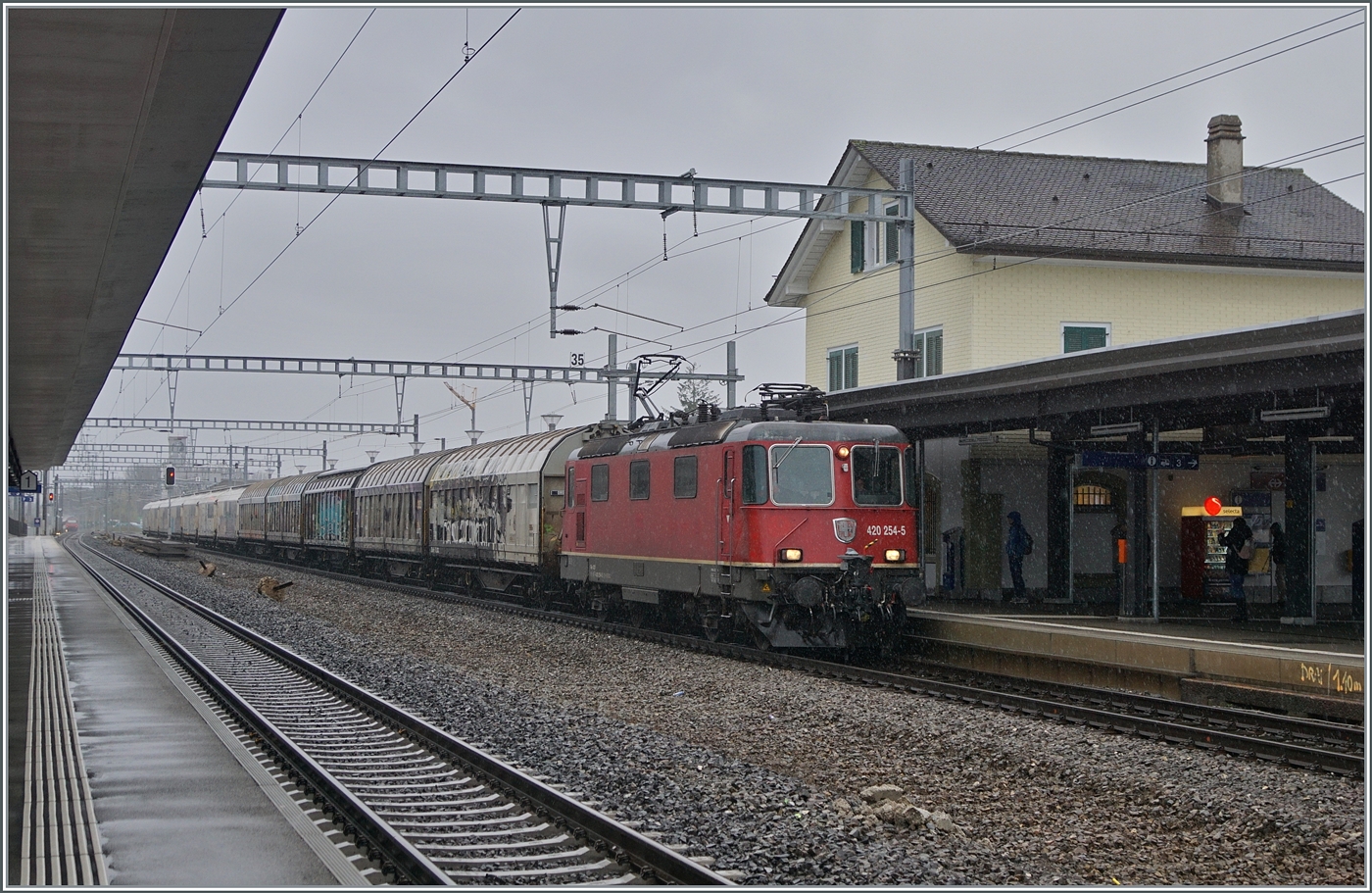 Die SBB R 4/4 II 11254-5 (Re 420 254-5) ist in Gland mit einem Güterzug in Richtung Lausanne unterwegs. 

22 Feb. 2024