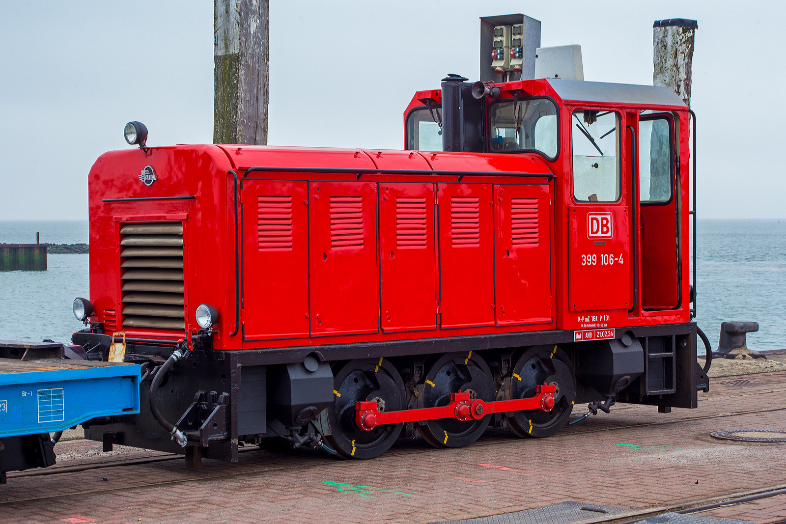 Die schmalspurige Diesellok 399 106-4 (98 80 3399 106-4 D-DB), eine der DB Fernverkehr AG bzw. der Wangerooger Inselbahn / SIW - Schifffahrt und Inselbahn Wangerooge steht am 13 März 2024, nun mit einem leeren Güterzug bestehend aus vierachsiger schmalspuriger Flachwagen DB 630xx, am Westanleger der friesischen Insel Wangerooge. Zuvor war der Güterzug beladen und wurde bereits mittels (20 t) Schwerlastgabelstapler entladen, bevor er wieder beladen wird, dies dauert aber gerade noch etwas, da gerade auch die Personenfähre MS Harlingerland angekommen ist.

Noch vor der Gründung der DB AG beschaffte die Deutsche Bundesbahn im Jahr 1992 zwei dreiachsige Kleinloks des rumänischen Typs Faur L18H vom ehemaligen Mansfeld-Kombinat für den Einsatz auf der Inselbahn Wangerooge. Sie sollten zunächst die Altbaulokomotiven der Baureihe 329 unterstützen, konnten aber die in sie gesetzten Erwartungen nicht erfüllen. Sie werden daher bis heute meist für kurze Güterzüge und als Reserve für die Personenzüge vorgehalten, wenn die Maschinen 399 107 und 399 108 nicht zur Verfügung stehen.

Die meterspurige Lok wurde 1990 vom rumänischen Hersteller FAUR S.A.(bis 1989 Faur Lokomotivwerke 23. August) in Bukarest unter der Fabriknummer 25666 gebaut und im April 1990 an das MKWP - VEB Mansfeld-Kombinat  Wilhelm Pieck  geliefert, wo sie kurz bei der zum Kombinat gehörenden meterspurige Schlackenbahn der August-Bebel-Hütte, ehemals bis 1951 Kochhütte, (eine Kupferhütte) in Helbra im Einsatz war. Am 10. September 1990 erfolgte der letzte Ofenabstich auf der Kochhütte. Die Gebäude und Betriebsanlagen wurden in den Folgejahren vollständig zurückgebaut, heute befindet sich hier ein Gewerbegebiet. So wurde bereits im November 1992 die Lok, wie eine weitere (399 105-6), an die DB - Deutsche Bundesbahn für die Wangerooger Inselbahn verkauft. Bevor sie dort zum Einsatz kam erfolgte im BW Wangerooge im Juli 1993 ein Umbau bzw. Anpassung an die EBO-Richtlinien und DB-Standards.

Insgesamt wurden zehn Diesellokomotiven der Baureihe L18H vom rumänischen Fahrzeug- und Maschinenherstellers FAUR zwischen 1983 und 1990 für verschiedene schmalspurige Wald- und Industriebahnen in Osteuropa gebaut. Es handelt sich um dreiachsige, stangengekuppelte Maschinen mit einem einseitigem Motorvorbau und Endführerstand sowie Antrieb in Z-Anordnung. Als Antrieb dient ein direkt angeflanschter Drehmomentwandler mit Lastschaltgetriebe und Achsgetriebe auf dem ersten Radsatz.

TECHNISCHE DATEN:
Spurweite: 	1.000 mm (Meterspur)
Achsformel: C
Länge über Puffer: 5250 mm
Höhe: 2.800 mm
Breite: 1.800 mm
Achsabstand: 2 x 900 = 1.800 mm
Treibraddurchmesser: 	750 mm
Kleinster befahrbarer Gleisbogen: R 20 m
Leergewicht: 16,0 t
Höchstgeschwindigkeit: 	28 km/h
Installierte Leistung: 132 kW
Motorentyp:  MAN (Lizenzbau) D2156 HM N8
Motorbauart: 6-Zylinder-Reihenmotor mit 10.350 cm³ Hubraum
Nenndrehzahl: 1.800/min
Leistungsübertragung: hydrodynamisch und mechanisch
Bremse: Druckluft
Lokbremse: Druckluft, indirekt
Kupplungstyp: Balancierhebel- bzw. Ausgleichkupplung (zp2)
