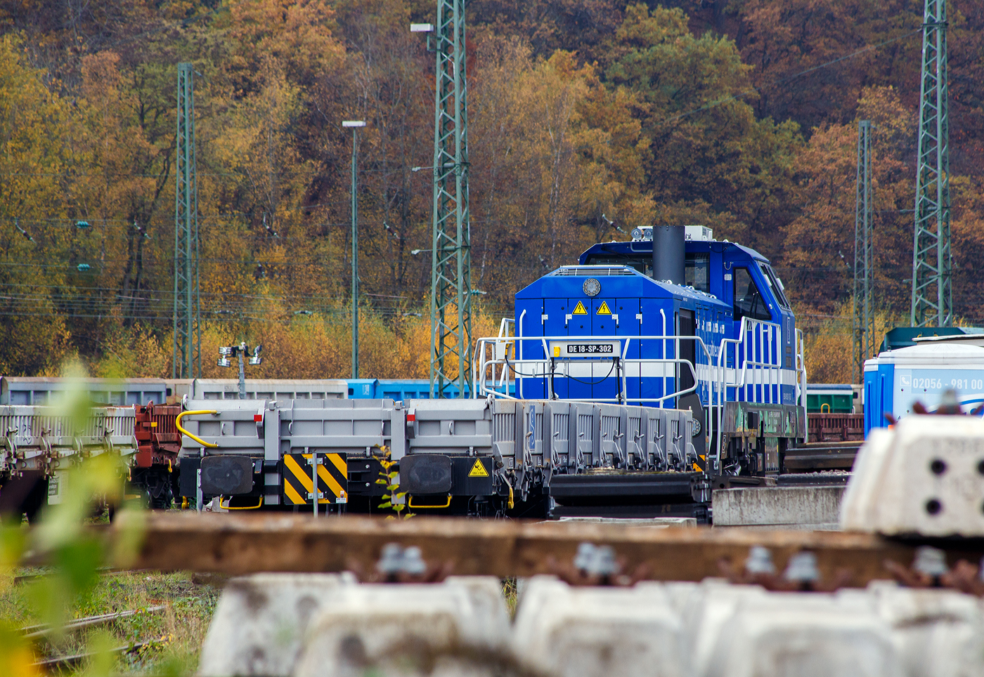 Die sehr neue SPITZKE DE18-SP-302 / 4185 302-1 (92 80 4185 302-1 D-SLG) eine dieselelektrische Vossloh DE 18 der SPITZKE SE steht am 08 November 2025 hinter einem Res-Wagen im Rbf Betzdorf/Sieg. 

Die DE18 wurde 2025 von der Vossloh Rolling Stock GmbH in Kiel unter der Fabriknummer 5502655 gebaut und am 14.08.2025 an die SPITZKE SE, Großbeeren ausgeliefert (Tag der Überführung).

Die Diesellokomotive der Baureihe DE 18 ist insbesondere für den schweren Rangier- und Streckenbetrieb mit hoher Zugkraft geeignet. Sie gilt als aktuell leistungsstärkste Mittelführerhauslokomotive auf dem europäischen Markt. Die DE 18 ist für den Rangierbetrieb mit einer Funkfernsteuerung ausgerüstet und ist für bis zu drei Loks mehrfachtraktionsfähig. Durch Energiesparmodus und Start-Stopp-System reduziert sie Schadstoffausstoß und spart Treibstoff ein, zudem besitzt sie einen Rußpartikelfilter. Zusätzlich lässt sich der Kraftstoffverbrauch durch ein effizientes Motormanagement und einer Begrenzung der Motorleistung, wenn nicht die Maximalleistung benötigt wird, reduzieren. Der 1.800 kW starke MTU Dieselmotor wird durch ein Batteriepaket ergänzt, das einen bis zu einstündigen emissionsfreien Rangierbetrieb gewährleistet und Fahrten durch Null-Emissions-Bereiche etwa in Tunneln, Werkhallen oder Bahnhöfen, ermöglicht.

Die Lok hat eine Anfahrzugkraft von 300 kN und eine Dauerzugkraft von 230 kN bei 24.2 km/h. Höchstgeschwindigkeit beträgt 120 km/h, die kleinste Dauerfahrgeschwindigkeit 3 km/h,
