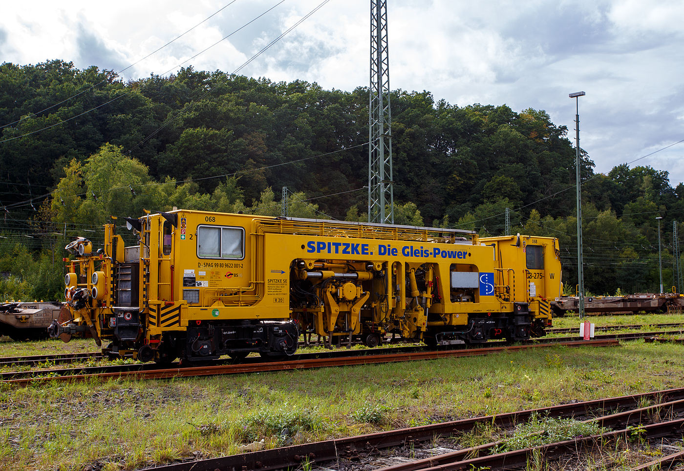 Die selbstverladbare halbautomatische Nivellier-, Hebe-, Richt- und Stopfmaschinen (Zweiwege-Stopfmaschine), D-SPAG 99 80 9622 001-2 „Zicke“ (SPITZKE Maschine 068), ex 97 43 43 510 10-9, vom Typ P&T 08 - 275/4 ZW-Y, der SPITZKE SE (Großbeeren) ist am 14. September 2025 in Betzdorf/Sieg abgestellt. 

Die selbstverladbare Zweiwege-Universalstopf- und Richtmaschine 08 - 275/4 ZW-Y wurde 1996 von Plasser & Theurer, Export von Bahnbaumaschinen, Gesellschaft m.b.H. in Linz/Donau (A) unter der Maschinen-Nr. 1069 gebaut und an die Spitzke GmbH geliefert. 

Die 08-275/4 ZW-Y haben 4 Achsen (in 2 Drehgestellen), ein längsverschiebbares Stopfaggregat und ist so auch für Y-Schwellen verwendbar. Die USM 08-275 4/ZWY sind halbautomatisch arbeitende Maschinen für Nivellier-, Hebe-, Richt- und Stopfarbeiten. Sie bearbeiten Weichen und Gleise, auch Gleise mit Y-Schwellen. Ihre Leistungsfähigkeit beweisen die Zweiwege-Universalstopfmaschinen auch beim Gleisbau für Straßenbahnen, U- und S-Bahnen. Mit einer separaten Messfahrt kann die Gleisanlage nach dem Stopfvorgang automatisch protokolliert werden. 

Durch die Ausstattung mit vier Verladehubzylindern kann sich die Maschine selbstständig aus- und eingleisen, so ist sie selbstverladbar für den Straßentransport auf einen Tieflader. Somit ist ein schienenunabhängiger Transport zur und von der Baustelle möglich. Ebenso kann sich dieser Maschinentyp ohne fremde Ladehilfe aus eigener Kraft auf das Gleis setzen. Zweiwegefahrbare Maschine heißt hier nicht, dass sie eigene Räder (wie die UST 79 S) für den Straßenverkehr besitzt, sondern sie kann sich mit eigener Kraft auf einen Tieflader verladen.

Um im Havariefalle das Fahrzeug abschleppen zu können besitzt die Maschine Scharfenberg- und Rockinger-Kupplungen. Die Stopfmaschine kann zusätzlich mit anderen Drehgestellen ausgerüstet werden, um auf Straßenbahnen und auf anderen Spurweiten eingesetzt zu werden.

Die Funktionsmerkmale sind:
-	Wechsel der Arbeitsrichtung auf asphaltierten Überwegen möglich
-	Flexibler Einsatz im Bauablauf
-	Zweiwege-Maschine
-	Transport auf dem Gleis oder auf dem Tieflader
-	Laden der Maschine auf den Tieflader bzw. vom Tieflader auf das Gleis erfolgt mit eigener Maschinenhydraulik
-	Richtungslaser
-	6-Kanal-Schreiber (08-275 4/ZWY) 
-	Automatischer Leitcomputer ALC mit EM-SAT Datenverarbeitung
-	Automatische Toleranz-Überwachung für die Arbeitsqualität
-	Sifa, Indusi und Zugfunkanlage
-	Einsetzbar auf DB-, Straßenbahn- und U-Bahnstrecken (08-275 4/ZWY)

TECHNISCHE DATEN:
Spurweite: 1.435 mm (Normalspur), Umbau auf andere möglich
Achsfolge: (A'A')(A'A')
Länge über Puffer: 14.800 mm
Höhe über SO: 3.170 mm
Drehzapfenabstand: 8.000 mm
Achsabstand in den Drehgestellen: 1.800 mm
Treib- und Laufraddurchmesser: 730 mm (neu)
Eigengewicht: 36.000 kg
Achslast: 9,0 t
Motorleistung (Dieselmotor): 170 kW
Höchstgeschwindigkeit: 40 km/h (eigen und geschleppt)
Min. befahrbarer Gleisbogen: R 20 m
Zur Mitfahrt zugelassene Personen: 3

Leistungsparameter der USM 08-275 4/ZWY:
Arbeitsleistung bei Durcharbeitung im Gleis: 400 m/h
Arbeitsleistung bei Durcharbeitung im Gleis (mit Y-Schwellen): 600 m/h
Arbeitsleistung bei Durcharbeitung von Weichen: 5 Weichen in 10 h
Arbeitsradius: min. 50 m
Fahrradius: min. 20 m
Arbeiten in Überhöhung: max. 180 mm

Bemerkung: Bekanntlich kommen nach einem Stopfvorgang immer Schotterverteil- und Planiermaschine wie z.B. SSP 110 SW zum Einsatz, aber hier bei dieser ZW-Stopfmaschinen verwendet man meist, da es kleinere Bauabschnitte sind, ZW-Bagger mit entspr. Anbaugeräte (Schotterpflug und hydraulischer Schotterbesen) zum Einsatz.

Quelle: Spitzke, Plasser & Theurer und Anschriften.
Stand: September 2025
