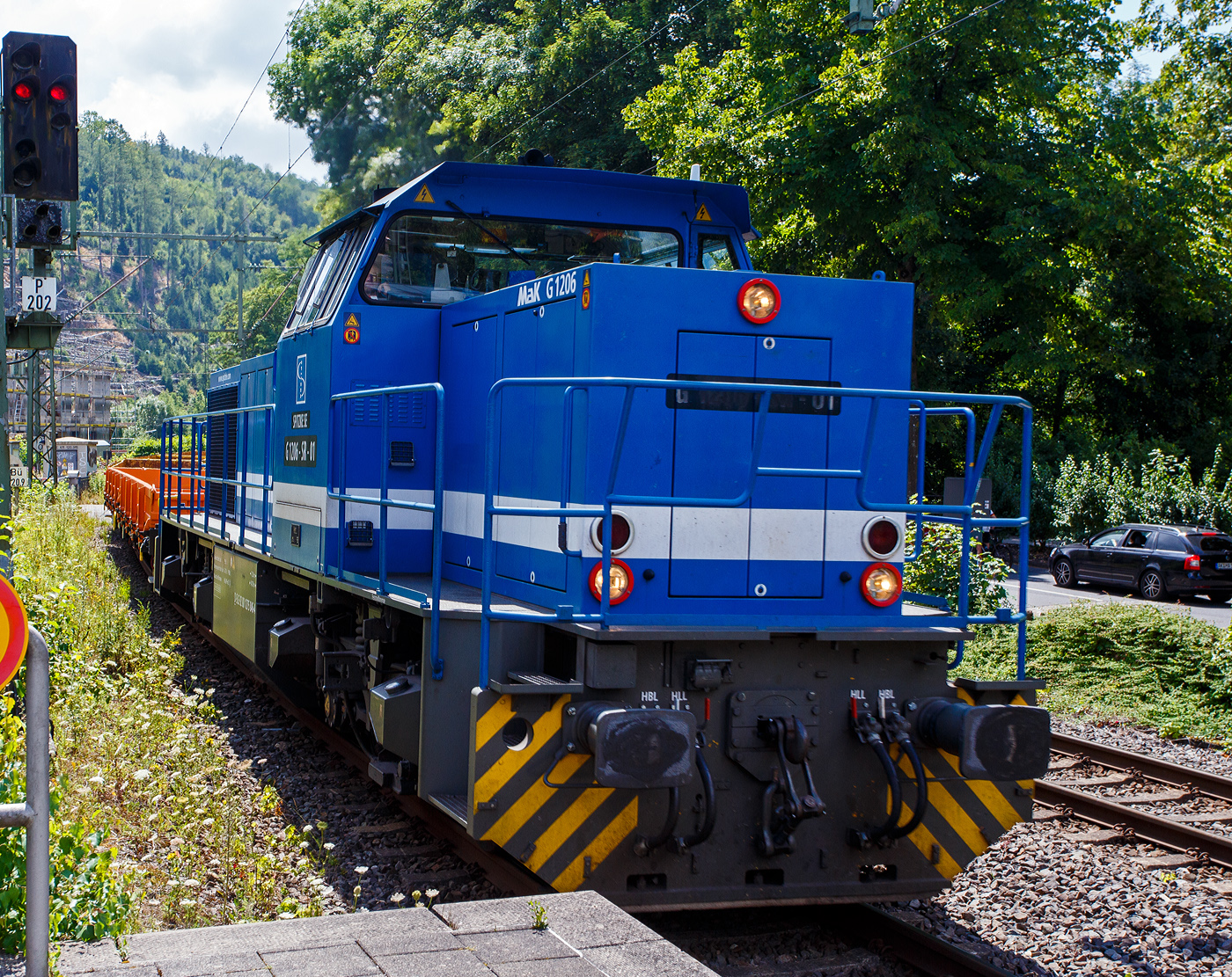 Die SPITZKE G 1206-SR-01 / 275 846-4 (92 80 1275 846-4 D-SLG) der SPITZKE SE (Großbeeren), ex XR 01 der SPITZKE RIEBEL GLEISLOGISTIK, ex V 200 001 der Xaver Riebel Gleisbau, fährt am 17 Juli 2025, mit einem Flachwagen-Güterzug (vierachsige Flachwagen mit Stahlfußboden, Seiten- und Stirnwänden der Gattung Res), durch Kirchen (Sieg) in Richtung Siegen.

Die MaK G 1206 wurde 2003 von Vossloh unter der Fabriknummer 1001382 gebaut und an die Xaver Riebel Gleisbau als V 200 001 geliefert.
Lebenslauf
18.03.2003 Auslieferung an Xaver Riebel Gleisbau GmbH & Co. KG, Buchloe  V 200 001  
09.12.2008 SRG - SPITZKE RIEBEL GLEISLOGISTIK GmbH, Buchloe  XR 01  (NVR-Nummer: 92 80 1275 846-4 D-XR)
Ab 01.07.2015 SPITZKE SE, Großbeeren  XR 01 (92 80 1275 846-4 D-SLG), später Umzeichnung in  G 1206-SR-01   

Die MaK G 1206 ist im schweren Rangier- und Streckendienst einsetzbar. Sie wurde 1997 zum ersten Mal gebaut und ist nach Deutschland, Österreich, der Schweiz, Luxemburg, Italien, Spanien, den Niederlanden und nach Frankreich verkauft worden. Allein 23 Lokomotiven fahren als BB 61000 bei der SNCF, davon sechs mit MTU-Motor (Die G 1206 gibt es wahlweise mit Caterpillar- oder MTU-Motor). Eine Weiterentwicklung der MaK 1206 ist die Vossloh G 1700 BB. 

Im Zuge der fortschreitenden Liberalisierung des Schienenverkehrs in Deutschland zeichnete sich Ende der 1990er Jahre ein zunehmender Bedarf an streckentauglichen Diesellokomotiven. Bei zahlreichen Bahnen bestanden damals Überlegungen, Verkehrsleistungen über das eigene Netz hinaus auf Gleisen der DB AG eigenständig zu erbringen, was in den folgenden Jahren auch vielfältig realisiert wurde.

Mit der G 1206 stand zwar im Prinzip schon eine für diese Einsätze geeignete Maschine zur Verfügung, jedoch gab es an der Maschine noch Verbesserungspotential, das nun genutzt wurde. Inzwischen standen in der benötigten Leistungsklasse neu entwickelten Motoren zur Verfügung, die mit 12 statt 16 Zylindern auskommen. Statt des in den Lokomotiven für die Dortmunder Eisenbahn verwendeten neuen MTU-Motors entschied man sich für die kommende Serienproduktion aber für einen technisch ähnlichen Motor von Caterpillar, den 3512B. Im Zuge der Anpassung der Lok an diesen Motor erhielt sie geringfügig breitere Motor- und höhere Getriebehauben, wodurch sich diese Loks schon äußerlich von ihren Vorgängern unterscheiden.

Ebenfalls überarbeitet wurde das Fahrwerk. Hier kamen weiterentwickelte Drehgestelle mit Lenkerführung für eine Höchstgeschwindigkeit von 100 km/h zum Einsatz. Die Radsätze werden bei diesen Drehgestellen nicht mehr von einer Gleitplattenführung sondern von verschleißfreien Lenkern geführt. Damit konnte nicht nur das Laufverhalten verbessert und damit die Höchstgeschwindigkeit gesteigert, sondern auch die Führung von Drehgestell und Radsatz weitgehend verschleißfrei ausgeführt werden. Für den Antrieb wurden nicht mehr die Radsatzgetriebe aus eigener Fertigung verwendet, sondern welche von ZF mit einer für die Höchstgeschwindigkeit besser geeigneten Übersetzung.

TECHNISCHE DATEN der G 1206:
Spurweite: 1.435 mm (Normalspur)
Antriebart: dieselhydraulisch
Achsfolge: B'B' 
Länge über Puffer: 14.700 mm
Drehzapfenabstand: 7.200 mm
Achsabstand im Drehgestell: 2.400 mm
größte Breite: 3.080 mm
Höhe über Schienenoberkante: 4.220 mm
Raddurchmesser neu: 1.000 mm
Motor: Caterpillar 12 Zylinder 4-Takt Dieselmotor mit Abgasturbolader und Ladeluftkühlung vom Typ 3512B DI TA-SC
Leistung: 1.500 kW bei1.800 U/min
Strömungsgetriebe: Voith L 5r4 zU2
Anfahrzugkraft: 267 kN
Höchstgeschwindigkeit: 100 km/h
max. Schleppgeschwindigkeit: 80 km/h
kleinste Dauerfahrgeschwindigkeit: 10 km/h
kleinster befahrbarer Gleisbogen:	60 m
Dienstgewicht: 87,3 t
mittlere Achslast: 21,8 t
Kraftstoffvorrat: 3.150 l
