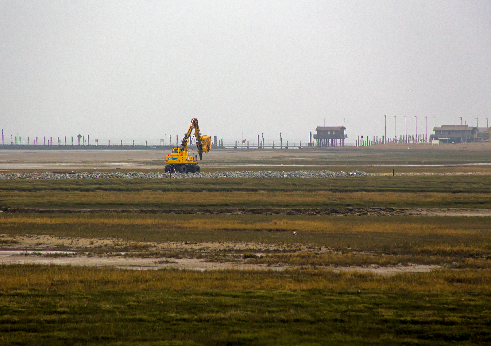 Ein ATLAS 1404 ZW-CR Zweiwege-Schmalspurbagger der SNG mit einem BSB - tinbin TC2 Saugbagger-Anbaugerät reinigt am Nachmittag des 12 März 2024 das Gleisbett der Wangerooger Inselbahn. Nun ist das Saugbagger-Anbaugerät gefüllt und der Bagger fährt zur Entleerung zum Westanleger (hinten rechts).

Der ATLAS Zweiwegebagger 1404 ZW-CR für 1.000 mm Spurbreite ausgerüstet, der niedriger Schwerpunkt und quer eingebauter Motor machen ihn standfest auf der schmalen Spur. 

Für den Zweiwege-Schmalspurbagger  ATLAS 1404 ZW-CR  Bagger im Einsatz auf schmaler Spur wurde ein den Anforderungen entsprechendes Fahrgestell gebaut und montiert. Der 1404 ZW ist mit 20 t Dienstgewicht der kleinste ATLAS Zweiwegebagger. Er ist mit einem Deutz Dieselmotor mit Turbolader vom Typ TCD 4.1 (mit 4.038 cm³ Hubraum)  der EU-Stufe V/US-EPA mit 95 KW/130 PS (bei 1.800 U/min) ausgerüstet. Eine Abgasnachbehandlungsanlage mit geschlossenem Diesel-Partikelfilter und kombiniertem SCR-Katalysator sorgen für Umweltfreundlichkeit. Die Linde Load- Sensing-Hydraulik in Verbindung mit dem ATLAS AWE 4 Hydraulikmanagement machen sensibles und millimetergenaues Arbeiten und Fahren möglich.

Das Kontergewicht ist integriert und beim ATLAS 1404 ZW in drei Heckradius- Varianten lieferbar 1.575 mm – 1.700 mm – 1.998 mm. Auf Wangerooge ist die 1.998 mm Variante im Einsatz. Ein niedriger Schwerpunkt und ein quer eingebauter Motor sorgen für optimale Stabilität und Standsicherheit beim Arbeiten auf dem Gleis. Auch beim Heben von wirklich schweren Gewichten bleibt der 1404 ZW trotz Schmalspur sicher und solide. Das Fahrwerk mit robusten, speziell konzipierten Baggerachsen mit Planetengetriebe in allen 4 Radnaben sowie Allradantrieb, Regelfahrmotor mit Lastschaltgetriebe und ein doppelt wirkendes Fahrbremsventil machen sichereres Fahren auf Straße und Schiene möglich. Ein Alleinstellungsmerkmal für ATLAS ist die Starrachse mit einem zuschaltbarem, 100%igem Sperrdifferential. Dieser 1404 ZW wird mit AWE 4 Technik über Reibräder angetrieben. Für diesen Einsatz auf Wangerooge wurden Achsen mit auf 1.000 mm reduzierter Breite montiert.