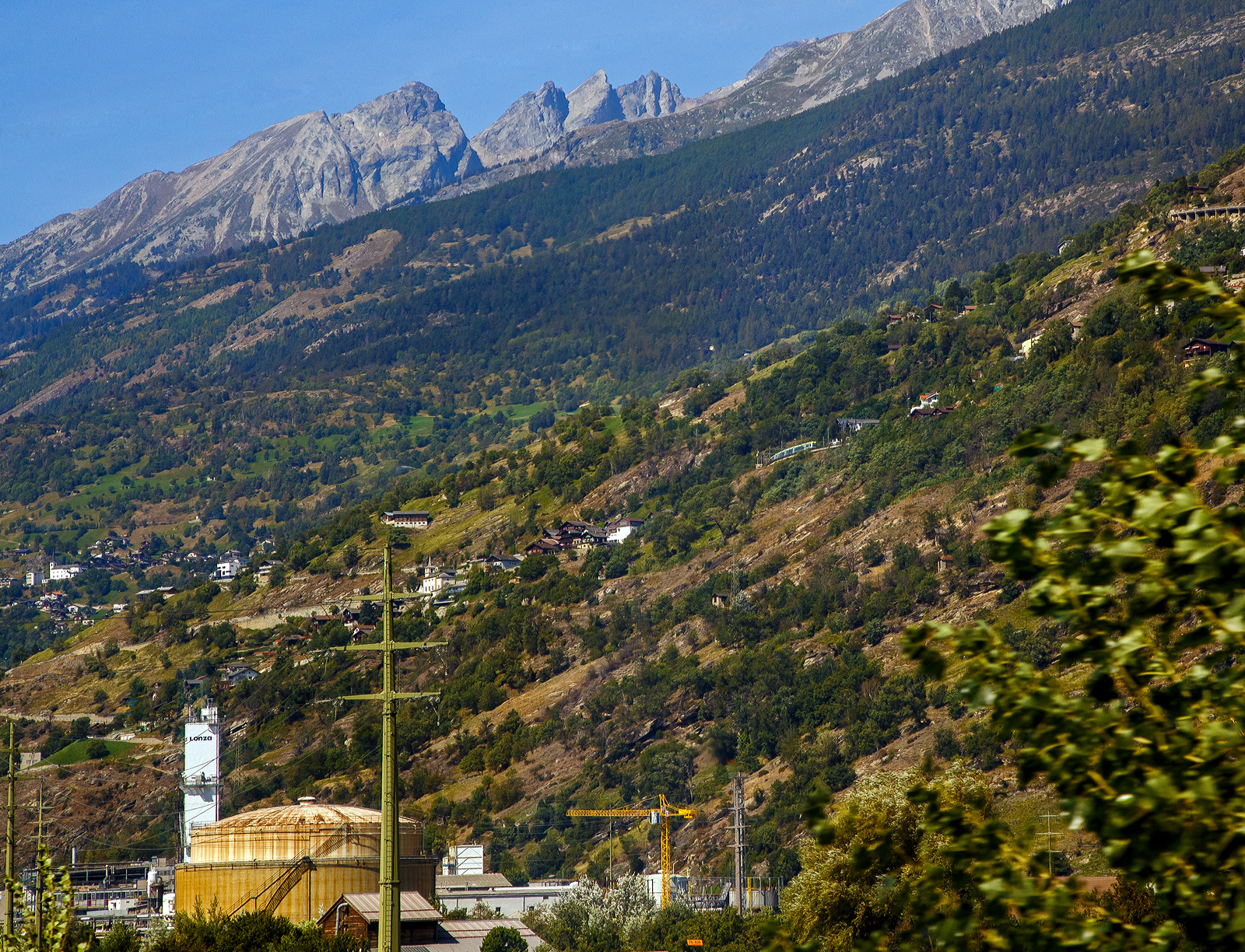 Ein Blick auf die BLS Lötschberg-Bergstrecke zwei gekuppelte BLS RABe 535  Lötschberger  fahren am 08.09.2021 beim Bahnhof Eggerberg (835 m ü. M.) gerade hinauf. 
Das Bild konnte ich durchs die Fensterscheibe aus dem SBB IC 8 (Brig – Romanshorn), hier kurz vor Visp machen.

Als Lötschberg-Bergstrecke wird die Schweizer Eisenbahnstrecke (Kursbuchfeld 330, vor Eröffnung des Basistunnels 300) bezeichnet, welche das Berner Oberland mit dem Wallis verbindet. Das Herzstück der Strecke ist der 14.612 m lange Lötschbergtunnel. Die Strecke ist aufgrund ihrer Doppelschleife (Kehrtunnel) an der Nordrampe, ihrer vielen Kunstbauten und der Südrampe im Rhonetal unter Eisenbahnenthusiasten weltbekannt. Mit der Eröffnung des Lötschberg-Basistunnels 2007 nimmt dieser nun einen Großteil des Verkehrs zwischen Frutigen und Brig auf. Die Bergstrecke wird seitdem nur noch durch RegioExpress- sowie von Güterzügen befahren, die nicht durch den Basistunnel befahren können.