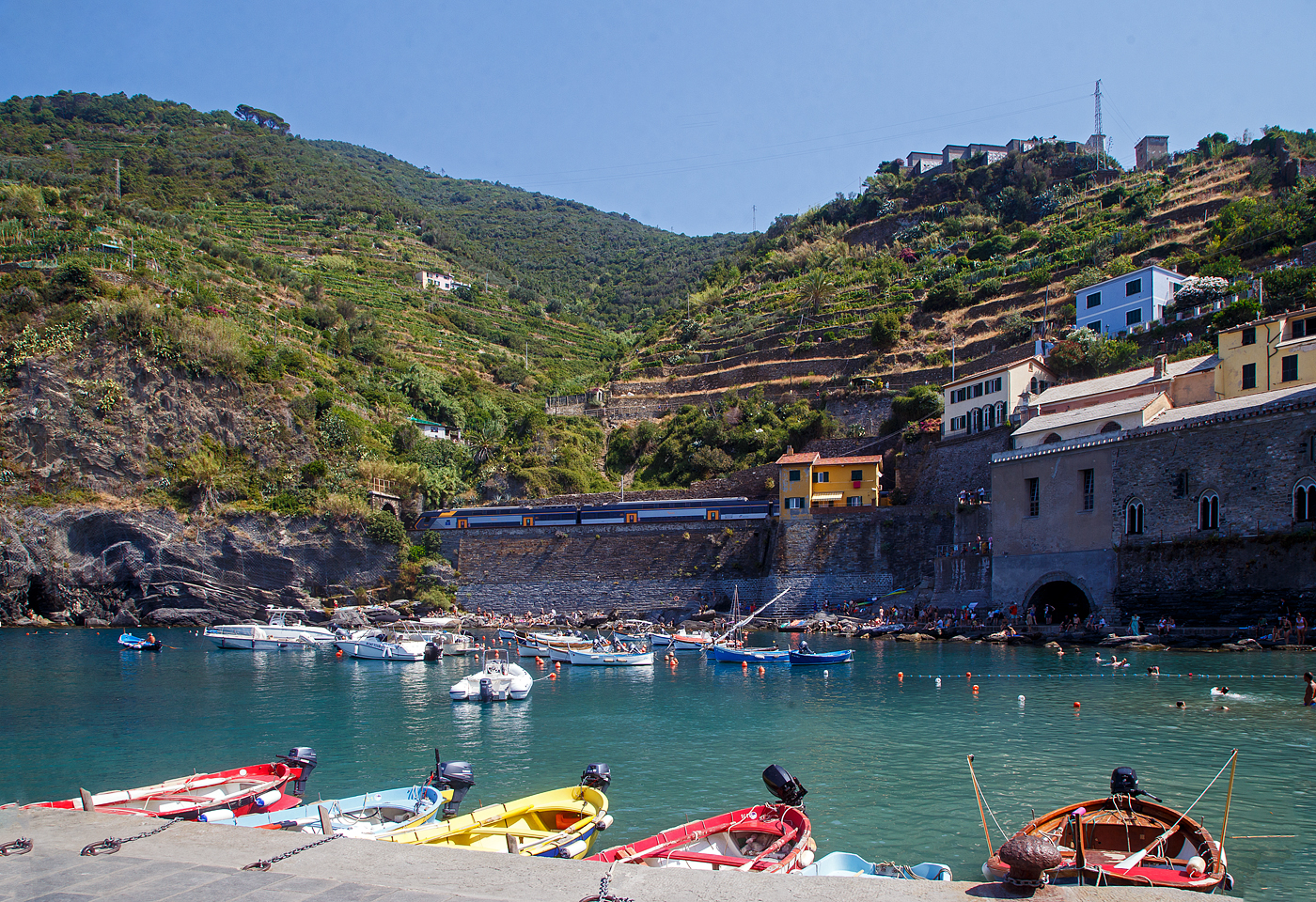 Ein Trenitalia “Rock” ETR 521, ein fünfteiliger Elektrotriebzug vom Typ Hitachi Caravaggio, verlässt am 22.07.2022 als Cinque Terre Express den Cinque Terre Bahnhof Vernazza und fährt weiter nach Levanto.

Vernazza ist eines der fünf Dörfer der Cinque Terre (Fünf Ortschaften) und verfügt, wie die anderen Dörfer, über einen Bahnhof an der Bahnstrecke Pisa–Genua (RFI Strecke-Nr. 77 / KBS 31 La Spezia–Genua). Der Bahnhof liegt zwischen zwei zweigeteilten Tunneln, jeder Bahnsteig hat seine eigenen Tunnelröhren. Wie auch in Riomaggiore passen die Bahnsteige nicht komplett unter freien Himmel, der Rest der Bahnsteige ist jeweils in einem der Tunneln.