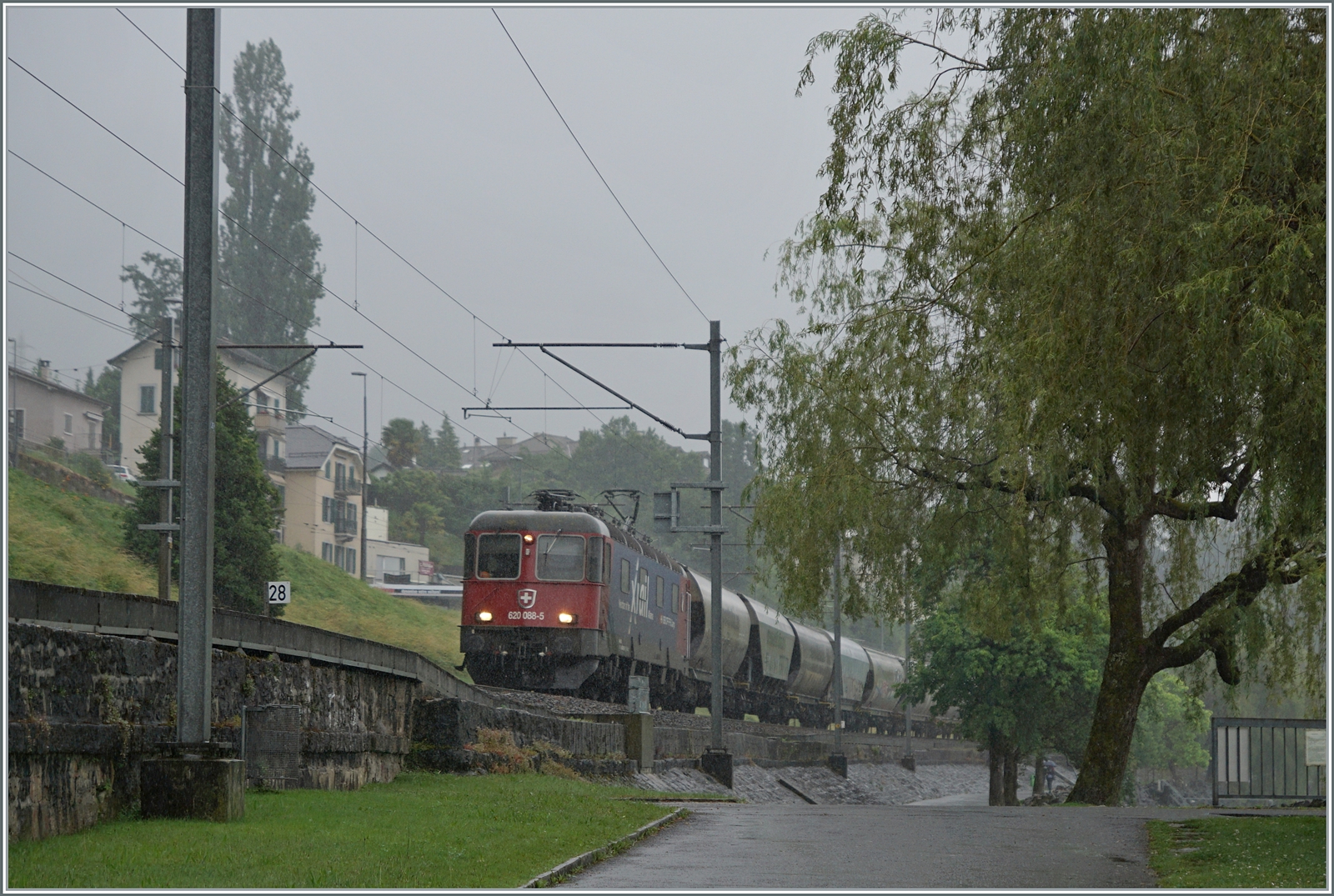 Es herrscht nicht gerade eitel Sonnenschein, als die SBB X-Rail Re 6/6 11688 (Re 620 088-5 / UIC Nummer Re 620  91 85 4620 088-5 CH-SBBC)  Linthal  mit dem  Spaghetti-Zug 47632 von Torino Orbassano (It) nach Perigny (F) kurz nach Villeneuve unterwegs ist. Die SBB Lok hat den Zug in Domo II übernommen und wird ihn in Vallorbe an die SNCF übergeben.

22. Juni 2024