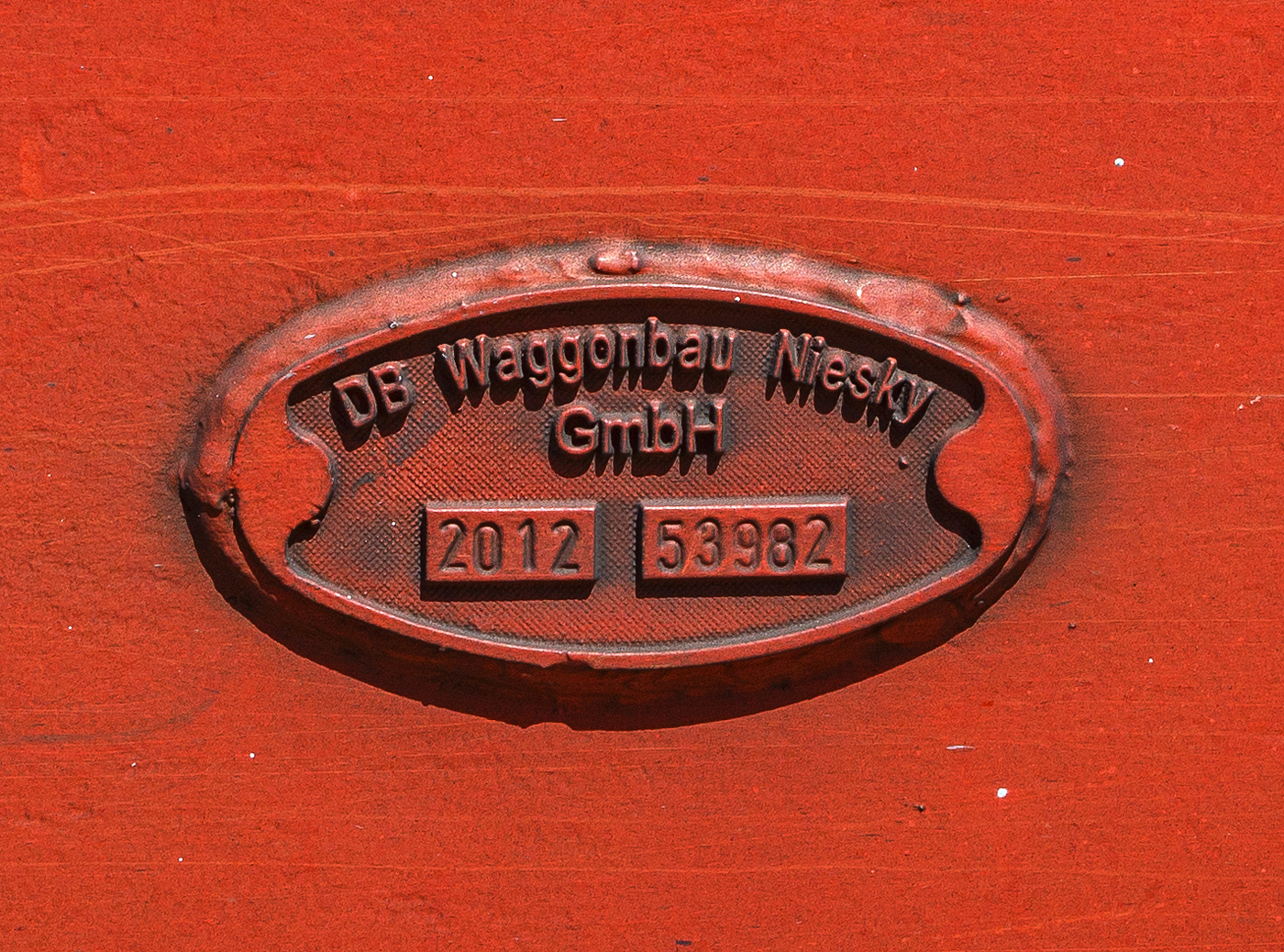 Fabrikschild „DB Waggonbau Niesky GmbH – 2012 – Fabriknummer 53982“ am vierachsigen (2 x zweiachsiger) Doppelstock-Autotransportwagen der Gattung Laaers 560.1 der DB Cargo Logistics GmbH (ex DB Schenker ATG) eingestellt als 25 80 4371 586-2 D-ATG am 28 Juni 2024 im Zugverband bei der Zugdurchfahrt in Rudersdorf (Kreis Siegen).

Geschichte vom Waggonbau Niesky
Im Jahr 1835 kaufte der in Niesky zugewanderte Kupferschmiedemeister Johann Ehrengott Christoph in der Horkaer Stra�e eine bestehende Kupferschmiede und begann am 5. Januar mit der Arbeit. Dies gilt als das Gr�ndungsjahr des Unternehmens. Der wirtschaftliche Erfolg des Unternehmens f�hrte im November 1898 zur Umwandlung in eine Aktiengesellschaft, die Firma wurde dabei verk�rzt zu Christoph & Unmack.

W�hrend des Ersten Weltkriegs wuchs der Bedarf an Holzbaracken stark an, was zu einer Erweiterung des Betriebs f�hrte. Hatte sich das Unternehmen bis dahin ausschlie�lich der Holzverarbeitung gewidmet, kam 1917–1918 zus�tzlich eine neu erbaute Waggonfabrik hinzu – zu einer Zeit, da im Waggonbau Bleche und Profile aus Metall zunehmend Holz als Baumaterial ersetzten. 1922 �bernahm die Christoph & Unmack AG auf dem Weg einer Fusion die ebenfalls in Niesky ans�ssige Maschinenfabrik J. E. Christoph. Fortan wurden auch Schienenfahrzeuge, Motore, Dampfmaschinen, Kessel und Stahlkonstruktionen hergestellt. Nun bestand die Christoph & Unmack AG aus vier Betriebsteilen; den Abteilungen Holzbau, Waggonbau, Stahlbau und Motorenbau. Besch�ftigt waren etwa 4.000 Personen. Das urspr�ngliche Aktienkapital von 1 Million Mark war durch den Kapitalbedarf f�r �bernahmen bzw. Fusionen, aber auch wegen der Hochinflation bis auf 100 Millionen Mark erh�ht worden, bevor es 1924 auf 8 Millionen Goldmark bzw. Reichsmark umgestellt wurde. 

Der Waggonbau
Neben der Herstellung von Holzbauten widmete sich die Christoph & Unmack AG ab 1917 auch der Herstellung von Schienenfahrzeugen. Unter anderem wurden in Niesky G�ter-, Post- und Reisezugwagen f�r die Deutsche Reichsbahn sowie Stra�enbahnwagen hergestellt. Zum Produktionsprofil geh�rten aber auch Br�cken, Motoren, Dampfmaschinen und andere Gro�ger�te aus Stahl. Ende der 1920er Jahre entwickelte die Waggonbaufabrik Christoph & Unmack in Kooperation mit der Sachsenwerk Licht- und Kraft AG Niedersedlitz einen neuen wegweisenden Stra�enbahn-Triebwagen, den sogenannten „Hechtwagen“, der in zwei Varianten als vierachsiger „Gro�er Hecht“ und zweiachsiger „Kleiner Hecht“ bei der Dresdner Stra�enbahn zum Einsatz kam. Auch die Stra�enbahn der Stadt K�strin erwarb sechs Trieb- und zwei Beiwagen von Christoph & Unmack.

1946 wurde der Betrieb enteignet und in Volkseigentum �berf�hrt. Unter der Firma VEB Waggonbau Niesky spezialisierte sich der Betrieb auf die Produktion von G�terwagen und G�terwagen-Drehgestellen. 1978 wurde er in das Kombinat Schienenfahrzeugbau der DDR eingegliedert.

1990 �bernahm die Deutsche Waggonbau AG (DWA) das Unternehmen. 1996 kam es in den Besitz der US-amerikanischen Advent International und geh�rte ab 1998 zum kanadischen Bombardier-Konzern, der hier 2001 sein europ�isches G�terwagenzentrum einrichtete. Zum 30. April 2005 wurde der Betrieb jedoch aus dem Bombardier-Konzern wieder herausgel�st und ging nach Insolvenz im Juli 2008 als selbstst�ndiges Unternehmen in den Besitz der Deutsche Bahn AG (DB Waggonbau Niesky GmbH) �ber. Diese gab am 16. Juli 2014 den Verkauf der Firma an die M�nchner Unternehmensholding Quantum Capitals bekannt, verbunden mit einer f�nfj�hrigen Standortgarantie. Das Unternehmen firmierte danach unter dem Namen Waggonbau Niesky GmbH.

Ende Dezember 2017 meldete der Waggonbau erneut Insolvenz an. Der Gesellschafter aus M�nchen war nicht in der Lage, den Verlust aus dem Gesch�ftsjahr 2017 auszugleichen. In den vorangegangenen Jahren habe Quantum jedoch die erzielten Gewinne aus dem Unternehmen herausgezogen und Investitionen seien nie geflossen. Trotz der Insolvenz lief der Betrieb unter Beibehaltung der Stammbelegschaft mit 300 Mitarbeitern weiter. Im September 2018 wurde das Unternehmen an den slowakischen G�terwagenhersteller Tatravag�nka Poprad verkauft. Seitdem hei�t das Unternehmen ELH Waggonbau Niesky GmbH. Im Mai 2023 ging das Werk mit noch 190 Mitarbeitern wieder in Insolvenz. Die Fortf�hrung des Betriebs ist nun leider gescheitert.
