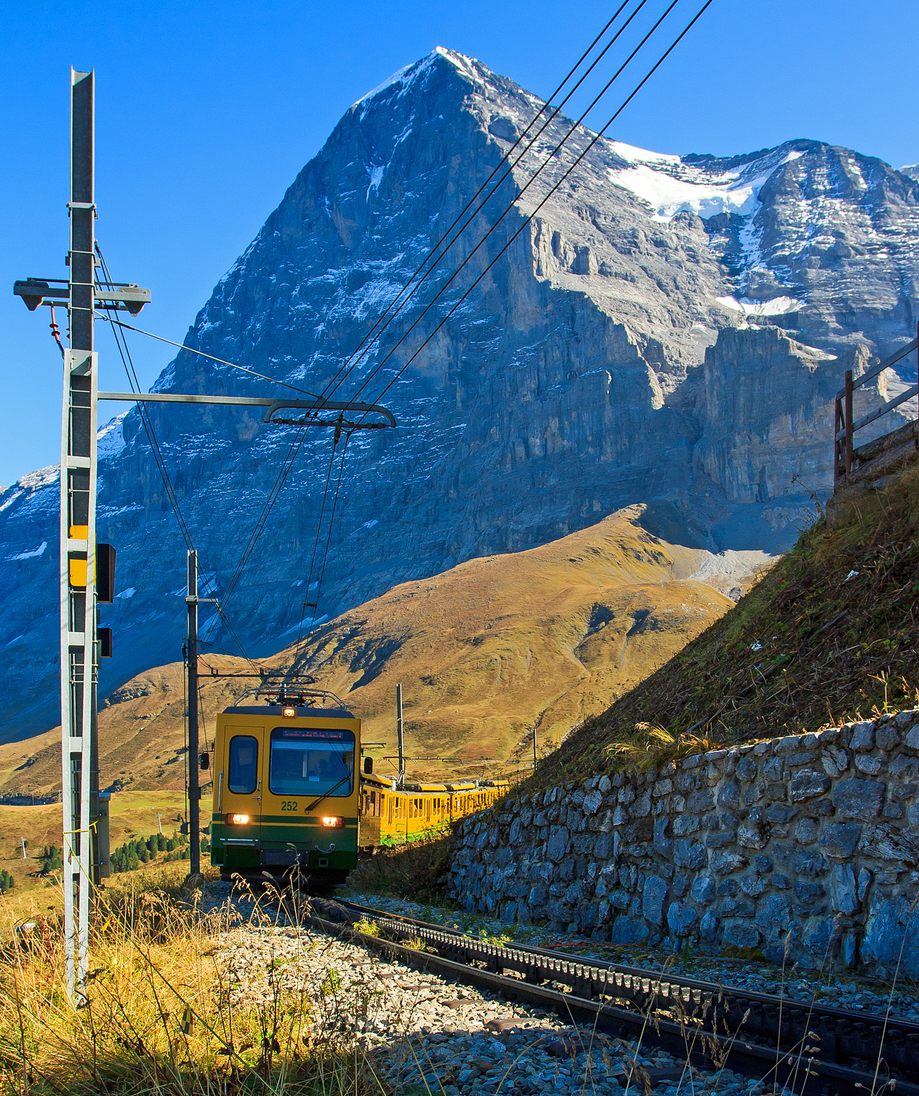 Geführt vom sechsachsigen Gelenksteuerwagen Bt 252 erreicht der WAB – Wengernalpbahn Zug von Grindelwald kommend am 02.10.2011 die Kleine Scheidegg.

Im Hintergrund die berühmte Eiger Nordwand.
