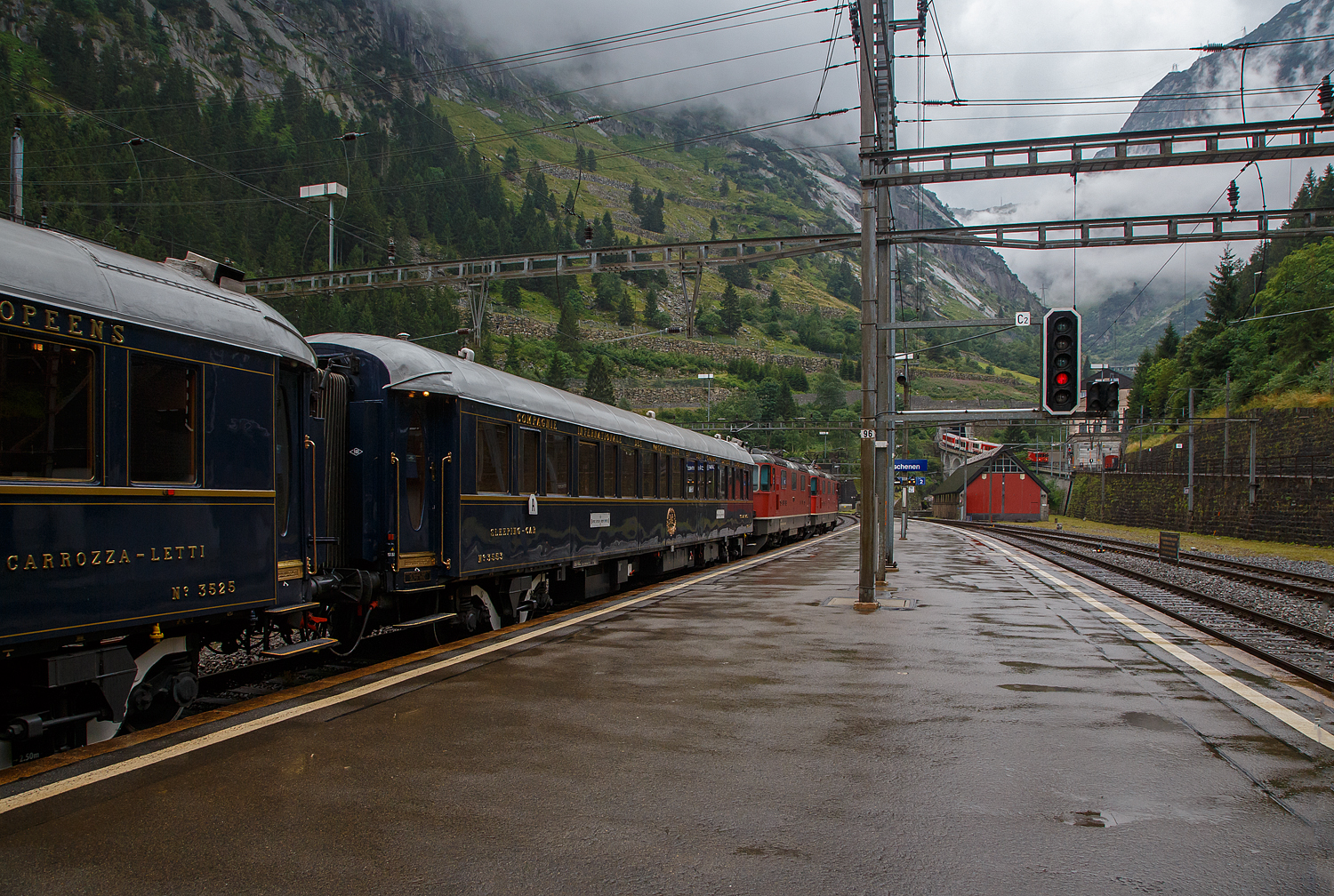 Gezogen von einer SBB Re 8/8 (Doppeltraktion der Re 4/4 11194 und der Re 4/4 11156) verlässt der VSOE - Venice Simplon-Orient-Express von Amsterdam über Brüssel und Paris nach Venedig am 02 August 2019, leider bei Regen, den Bahnhof Göschenen. Hier fährt er nicht, wie es im Namen steht, durch den Simplon, sondern über den Gotthard. Der „König der Züge“ der Orient-Express, bestand aus einem Zug mit 18 Wagen, es waren modernisierte historische ehemalige CIWL-Wagen. Ob es auch einen „Mord im Orient-Express“ gab? Das kann ich nicht sagen, hatte aber gehört das man wohl einen im Zug nachspielte.

Übrigens, rechtshinten kommt gerade der meterspurige Elektrische Zahnradgepäcktriebwagen MGB Deh 4 /4 II - 93 „Oberwald“, ex FO Deh 4/4 II – 93, mit seinem Schöllenenbahn Regionalzug von Andermatt nach Göschen hinab. Allein dieser wäre für mich schon Bilder wert, aber hier habe ich doch lieber das Augenmerk auf den „König“ gehalten😉

Hier gleich hinter den Loks der Schlafwagen Nr. 3553 – VSOE Voiture-Lits / Carrozza-Letti N° 3553 (F- VSOE 61 87 06-70 553-9 [P]), seit 2024 läuft dieser Wagen nach Umbau nun als N° 3553 - L'Observatoire (Privatwagen) im VSOE, nun der UIC-Nummer F- VSOE 61 87 76-70 000-6 [P].

Der Schlafwagen, wurde 1929 von EIC - Entreprises industrielles des Charentes (EIC, heute zu Alstom gehörend) in Aytré (F), als CIWL Typ Lx 18 (Schlafwagen mit Schlafwagenschaffnerabteil), gebaut und als Schlafwagen Nr. 3553 an die CIWL - Compagnie Internationale des Wagons-Lits geliefert. 1943 wurde er zum in den Typ LX 20 (zehn Zweibettabteile) umgebaut. Im Jahr 1980 wurde er an die VSOE (Venice Simplon-Orient-Express Ltd.) verkauft. Hier wurde der Wagen überholt und technisch modernisiert, unter anderem mit Klimaanlagen. Bei den VSOE-Wagen wurde ein Schlafwagenabteil zum Abteil für den Schlafwagenschaffner hergerichtet, die Wagen werden seitdem (wieder) als Typ Lx 18 bezeichnet. 

Zwischen 2003 und 2006 wurde die Wagen der VSOE wieder modernisiert und erhielten unter anderem moderne Drehgestelle von Bombardier sowie neue Klimaanlagen. Durch die neuen Drehgestelle sind die Wagen seitdem für 160 km/h zugelassen. 

TECHNIK
Mit der Einführung von Ganzstahlwagen ging die CIWL dazu über, von Ausnahmen abgesehen alle Fahrzeuge auf einem einheitlichen Rahmen mit 23.452 mm Länge über Puffer und einem Drehzapfenabstand von 16.000 mm aufzubauen. Die Fahrzeugbreite beträgt 2.850 mm, die Höhe über Schienenoberkante 4.000 mm. Auf dieser Basis entstanden neben dem Typ Lx auch die Schlafwagen der Typen S, Y und Z. Die gleichen Rahmen wurden auch für Speisewagen und Pullmanwagen verwendet, sie bestehen aus drei Längsträgern mit Querverbindungen und zwei Gussstahlblöcken an den Enden zur Aufnahme der Zug- und Stoßvorrichtungen. Auf dem Rahmen sind die Seitenwände und Fußböden sowie die beiden Zustiegsplattformen aufgebaut. Das Gewicht des Typs Lx beläuft sich auf 53 Tonnen (heute 57 t). Als Drehgestelle erhielten die Wagen ursprünglich Schwanenhals-Drehgestelle mit Rollenlagern, auch als Pennsylvania-Drehgestelle bezeichnet. Im Laufe der Jahre wurden diese teilweise durch neuere Drehgestelle oder andere Bauarten ersetzt. Ursprünglich waren die Wagen lediglich für 130 km/h zugelassen, nach dem Krieg wurde die Geschwindigkeit auf 140 km/h angehoben. Die mit neuen Drehgestellen modernisierten Wagen des VSOE sind für 160 km/h zugelassen.

Die CIWL rüstete alle Wagen neben einer über die Heizdampfleitung des Zuges versorgten Dampfheizung mit einer unabhängig zu betreibenden Kohleheizung aus, die durch den Schlafwagenschaffner bedient wurde und bei längerem Stillstand eines Zuges zum Einsatz kam. In den Nachkriegsjahren erhielten viele Fahrzeuge außerdem elektrische Heizleitungen. In jedem Abteil befand sich zur Belüftung ein Ventilator, die Wagen der VSOE wurden mit Klimaanlagen ausgerüstet.

Es gab kein gesondertes Abteil für den Schlafwagenschaffner, dieser nächtigte auf einer an einem Ende des Wagens aufgeklappten Liege im Gang. Vorräte für die Versorgung der Fahrgäste befanden sich in Schränken an den Wagenenden. An einem Ende war ein WC untergebracht. Jeweils zwei der Abteile (mit Ausnahme der beiden äußersten Abteile) ließen sich mittels einer verschließbaren Tür zu einer größeren Suite verbinden. Die in den historischen Luxuszügen eingesetzten, noch erhaltenen Wagen des Typs sind teils umfassend modernisiert und umgebaut worden. Bei den im VSOE eingesetzten Wagen wird eines der Abteile für den Schaffner genutzt. Die Wagen besitzen zudem moderne Klimaanlagen.

TECHNISCE DATEN:
Spurweite: 1.435 mm (Normalspur)
Anzahl der Achsen: 4 in zwei Drehgestellen
Länge über Puffer: 23.452 mm
Drehzapfenabstand: 16.000 mm
Achsabstand im Drehgestell: 2.500 mm
Eigengewicht: 57 t
Höchstgeschwindigkeit: 160 km/h (ursprünglich 140 km/h)
Betten- und Sitzplätze: 18 (in 9 Zweibettabteilen) plus Schaffnerabteil 

DER HEUTIGE WAGEN 3553 - L'Observatoire
Im Jahr 2023 entwarf französische Künstler JR das Innere des neuen Privatwagens 3553 - L'Observatoire (Privatwagen) des Venedig Simplon-Orient-Express, der so 2023/24 umgebaut wurde und nun die UIC-Nummer F- VSOE 61 87 76-70 000-6 [P] trägt. Jetzt ist es ein Privatwagen mit einem Schlafzimmer für zwei Personen, einem Wohnzimmer, einer Bibliothek, einer Teekammer und einem Badezimmer mit freistehender Badewanne. Das Fahrzeug wurde im April 2024 auf der Biennale in Venedig ausgestellt, um erste Eindrücke zu liefern, und es läuft seit 2025 im Zug des Venice Simplon-Orient-Express. Ich würde ich gerne mal selbst von innen sehen. 

L’Observatoire, dass sich über einen ganzen Wagen an Bord des Venedig Simplon-Orient-Express entfaltet, ist ein einzigartiger Raum, um Neugier, Abenteuer und Kreativität zu genießen. Inspiriert von astronomischen Observatorien hat der Künstler JR eine wagengroße Suite entworfen, er soll ermutigen, zu blicken, hinaus und darüber hinaus - und zwar mit Handwerkskunst sowohl von alten Meistern als auch von aufstrebenden Wegbereitern harmonieren. Wenn man das nötige Kleingeld hat😉.

In einem 23 Meter langen Raum entfalten sich die Innenräume des Wagens in mehreren Umgebungen, von einem Schlafzimmer mit einer freistehenden Badewanne bis zu einer Bibliothek voller Gallimard-Bücher. Wenn man den Korridor entlang schlendert, kann man die ausgestellte JR-Fotografie bewundern. Ein Plattenspieler mit einer kuratierten Vinyl-Sammlung ist als Soundtrack zum außergewöhnlichen Abenteuer auch dabei.

Zudem heißt es: Enthüllen Sie handgefertigte Intarsien, Glasmalereien und sogar einen Miniatur-Zugwagen, der von einem Modellbaumeister aus der Schweiz geschaffen wurde. Schauen Sie näher, um eine Welt von Feiernden zu entdecken, die auf winzigen Bildschirmen im Inneren des Modells laufen. Entdecken Sie die versteckte Teestube, ein kreisförmiges Refugium, in dem Sie Momente stiller Kontemplation genießen können. Dieser exklusive Raum ist nur für Ihre Augen reserviert. Schließlich schauen Sie auf, um einen Oculus zu enthüllen und den Himmel zu bestaunen.