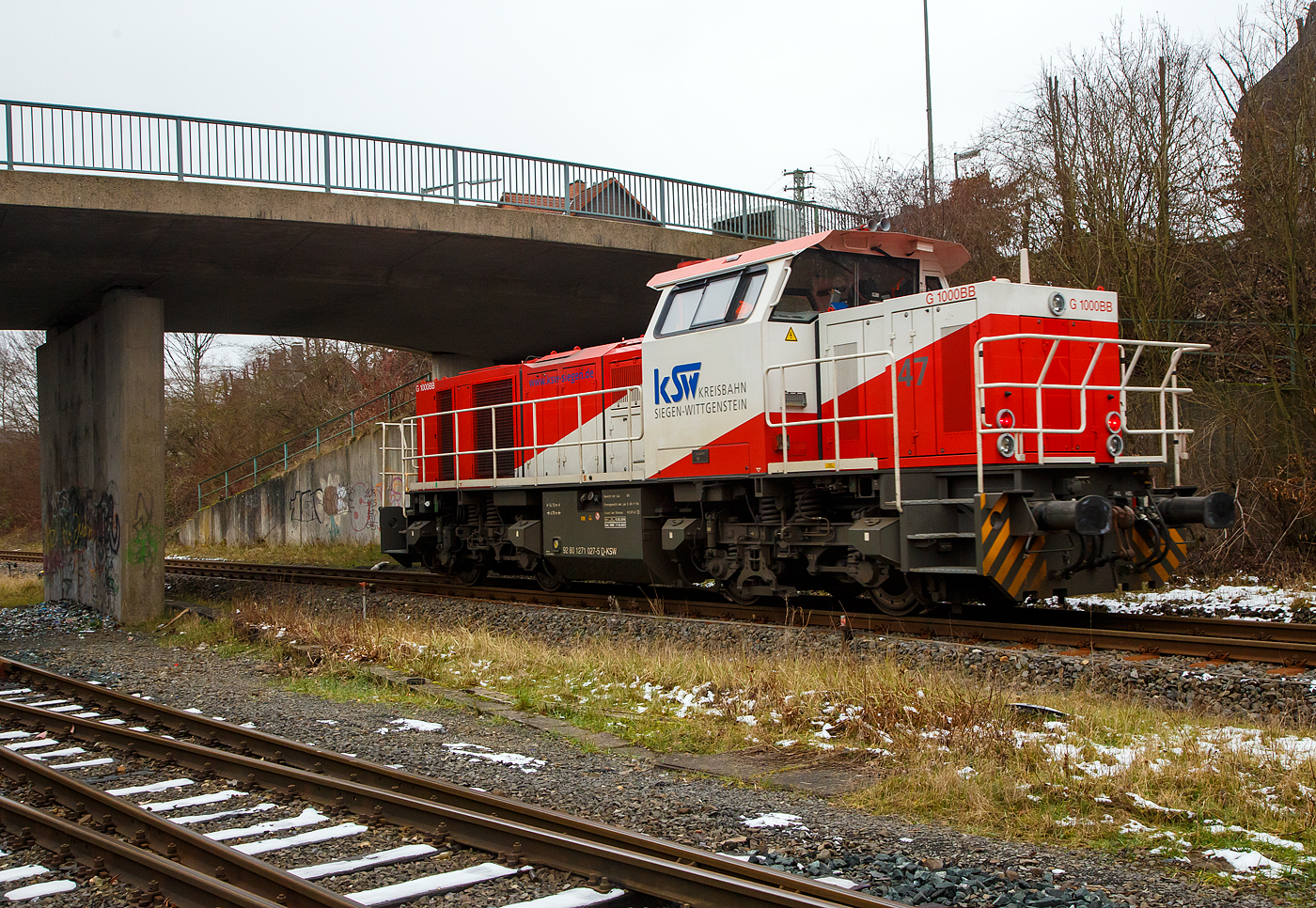 Güterverkehr gibt es noch in Herdorf....
Die KSW 47 (92 80 1271 027-5 D-KSW), ex D 2 der HFM, eine Vossloh G 1000 BB der KSW (Kreisbahn Siegen-Wittgenstein), fährt am 24.01.2023 von Herdorf auf der Hellertalbahn (KBS 462 / Strecke-Nr. 2651) in Richtung Haiger los.

Normalerweise würde sie in Richtung Betzdorf fahren, aber der Streckenanschnitt Herdorf – Betzdorf ist bis min. Ende April gesperrt, so muss die KSW den Umweg über Haiger fahren. Wobei hier als Lokzug ist es nur der Umweg und der entsprechende Mehrverbrauch an Kraftstoff, aber für den Güterverkehr ist noch die Streckenklasse sehr entscheidend und die beträgt bei dem Streckenanschnitt Herdorf – Haiger nur CE (anstatt D4 zwischen Betzdorf und Herdorf). Bei CE beträgt die Radsatzlast max. 20 t bei D4 aber 22,5 t. Dadurch kann ein Coil weniger geladen werden, da man nicht gerademal Coils vierteln kann, ergibt sich daraus ein bis zu 35% geringeres Ladegewicht und ein Mehraufwendung von Waggons.
