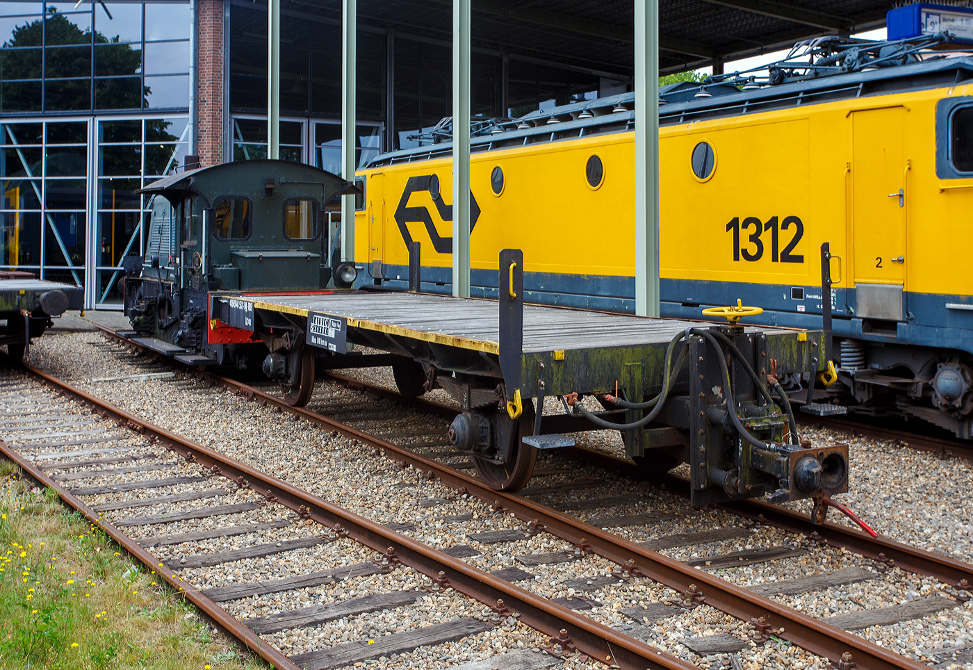 Hinter der ex NS Sik 311 der zweiachsige Kupplungswagen (Koppelwagen) ex 40 84 9441 532-1 NL-RFF (Rotterdam Rail Feeding), ex 30 84 9820 501-9 NL-NS, ex NS 61844, der Gattung U741, am 24 Juni 2025 im Het Spoorwegmuseum (bis 2005 NSM - Nederlands Spoorwegmuseum / Niederl�ndischen Eisenbahnmuseum) in Utrecht im ehemaligen Bahnhof Maliebaan. 

Diese Adapter- oder Kupplungswagen sind n�tig, wenn man mit einer Lok mit Puffern und Schraubkupplung Triebwagen und -z�ge mit Scharfenberger-Kupplung rangieren oder abschleppen muss. 

Nach dem Umbau (ca. 1970) aus Flachwagen erhielt der Wagen an einem Wagenende eine h�henverstellbaren Scharfenberger-Kupplung und wurde in Hoek van Holland stationiert. Die Kupplungsh�he ist von 610 mm �ber Schienenoberkante bis 1.070 mm verstellbar, sodass er an alle Stromlinienfahrzeuge gekoppelt werden kann. Am anderen Wagenende behielt er die Puffer und Schraubkupplung, so kann er an diese Seite an eine Lok gekuppelt werden. An der Unterseite des Fahrgestells sind au�erdem l�ngs 15 Stahlschienen f�r zus�tzlichen Ballast angebracht. An drei Ecken wurden Rangiertritte und Eckpfosten mit Griffen angebracht.

Auff�llig ist (nach meiner Sichtung), dass der Wagen keine eigenen Bremsen hat. Er hat aber durchg�ngige Bremsluftleitungen, so dass die abzuschleppende Triebz�ge von der Lok mit der erforderlichen Druckluft f�r die Bremsen versorgt werden konnten. Wobei hier der Sik 311 (Rangierlok) wohl nicht eine ausreichende Luftmenge liefern kann, da der rein mechanisch gebremst wird und keinen Kompressor besitzt.

TECHNISCHE DATEN:
Spurweite: 1.435 mm (Normalspur)
Anzahl der Achsen: 2
L�nge �ber Puffer: 9.550 mm
Achsabstand: 5.000 mm
Ladefl�che: 
Leergewicht: 9.000 kg
Max. Zuladung: 0 kg (Nur als Kupplungswagen verwendbar)
H�chstgeschwindigkeit: 80 km/h