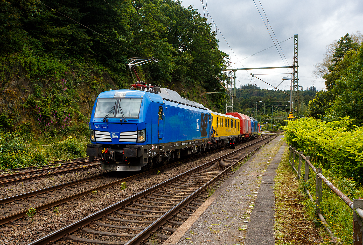 Im Sandwich zweier SIEMENS Vectron Dual Mode fährt ein Schienenprüfzug (SPZ 3), auf Prüffahrt (der Messwagen ist auf die Schiene absenkt) am 14 Juni 2024 durch Scheuerfeld/Sieg in Richtung Siegen.

Die vierteilige Komposition bestand aus:
• Der SIEMENS Vectron Dual Mode der 248 027-5 (90 80 2248 027-5 D-PRESS) alias 248 106-8 der PRESS (Eisenbahnbau- und Betriebsgesellschaft Pressnitztalbahn mbH, Jöhstadt).
• Dem Messwagen SPZ-STW (STW steht für Steuerwagen) 720 301(99 80 9360 006-7 D-DBMP) der DB InfraGO AG, ehemals DB Netz AG (NetzInstandhaltung/Fahrwegmessung).
• Einem Hilfszug-Wagen (Nummer unbekannt) der DB Netz AG (Notfalltechnik) bzw. DB InfraGO AG.
• Und der SIEMENS Vectron Dual Mode der 248 026-7 (90 80 2248 026-7 D-PRESS) alias 248 105-9 der PRESS (Eisenbahnbau- und Betriebsgesellschaft Pressnitztalbahn mbH, Jöhstadt).

Die Energieversorgung vom Messwagen und dem Hilfszug-Wagen erfolgte von den Loks (spartanisch) über außenverlegte Kabel.

Normalerweise ist der Schienenprüfzug ein zweiteiliger Messtriebwagen, bestehend aus Trieb- (ATW - 719 301) und einem Steuerwagen (STW - 720 301), siehe u.a. http://hellertal.startbilder.de/bild/Deutschland~Unternehmen~DB+Netz+AG/773623/der-plasser--theurer-schienenpruefzug-der.html Warum es nun diese Komposition ist, das ist mir nicht bekannt, vielleicht setzt man nun noch mehr auf E-antrieb.

Der Schienenprüfzug wurde 2015 von Plasser & Theurer in Linz (A) unter der Fabriknummer 6003 (SPZ-STW) gebaut. Um Schäden am Oberbau frühzeitig zu erkennen, setzt die Deutsche Bahn AG verschiedene Prüfzüge der Baureihen 719 und 720 ein. Mittels zweier zerstörungsfreier Prüfverfahren werden die Schienen auf Schädigungen untersucht. Bei der Ultraschallprüfung können Materialfehler durch Materialermüdung innerhalb der Schiene bis zum Schienenfuß erkannt werden. Mit der Wirbelstromprüfung wird der Schienenkopf geprüft.

Die beiden SIEMENS Vectron Dual Mode wurden 2022 von SIEMENS in München-Allach, unter den Fabriknummern 23168 und 23169, gebaut und an die PRESS - Eisenbahnbau- und Betriebsgesellschaft Pressnitztalbahn mbH in Jöhstadt geliefert. Die beiden Vectron DM haben die Zulassung in Deutschland für eine Höchstgeschwindigkeit 160 km/h.

Der Vectron Dual Mode vereint die Vorteile einer vollwertigen Diesellokomotive mit denen von elektrischen Lokomotiven. Dank des leistungsstarken Dieselantriebs sowie der Ausstattung für die Nutzung der Fahrleitung kann man jederzeit flexibel auf die Traktionsanforderungen reagieren. So bleibt man immer in Bewegung, egal ob mit oder ohne Fahrdraht. Wo ein Fahrdraht ist, sollte man ihn nutzen. Denn der Betrieb unter Oberleitung ist im Vergleich zum Dieselbetrieb deutlich kosteneffizienter und umweltfreundlicher. Doch weil es in Deutschland noch lange Zeit Strecken geben wird, die nicht vollständig elektrifiziert sind, fahren viele Diesellokomotiven unter Fahrdraht weiter. Das ist aber ökonomisch und ökologisch wenig sinnvoll. Dies ist hier ein Beispiel einer echten Alternative.