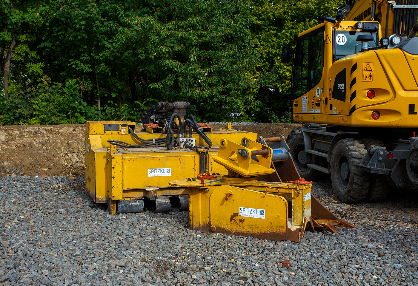 In Betzdorf/Sieg am 14 September 2025 abgelegte Gleisbau-Anbaugeräte für ZW-Bagger der SPITZKE SE (Großbeeren). 

Vorne ein Schotterpflug S1, mit diesem wird immer eine Gleishälfte planiert. Das Umsetzen des Schotters von links nach rechts und umgekehrt ist durch das Verstellen der Seitenklappen kein Problem. Das aufwendige Umsetzen des Schotters mittels Greifer oder Schaufel entfällt.

Einstellungsmöglichkeiten der Seitenbleche:
•	Seitenbleche werden V-Förmig angeordnet, wenn der vorhandene Schotter nur verteilt und die Schwellen gereinigt werden sollen.
•	Außen liegender Schotter wird in die Mitte befördert, durch einfaches Umschwenken der Seitenbleche. Um Schotter von innen nach außen zu befördern, werden die Bleche nur entgegengesetzt angeordnet.
•	Soll der Schotter nach außen befördert werden, dann werden die Seitenblech entsprechend entgegengesetzt eingestellt.
Das Gewicht von dem Schotterpflug S1 beträgt 800 kg.

Hinten ein hydraulischer Schotterbesen HSB 2, mit diesem wird der Schotter im ganzen Gleis gekehrt. 

Einsatzmöglichkeiten:
Der Schotterbesen ist durch seine Kompaktheit und seine höhenverstellbaren Führungsrollen in jedem Gleis einsetzbar. Ob Betonschwellen oder Holzschwellen, er ist überall verwendbar. Selbst die Förderrichtung des Schotters nach links oder rechts kann vom Bagger aus umgestellt werden.

Der Schotterbesen wird in den Baggerstiel eingeführt oder wie hier der Bagger nimmt ihn mit Schnellwechselsystem auf. Dann müssen noch die Hydraulikleitungen verbunden, was sich hier mit Liebherr-Schnellwechselsystem LIKUFIX erübrigt, da auch die Hydraulikanschüsse gleichzeitig ankuppelt. Nun kann der Bagger den Schotterbesen über das Gleis schieben. Durch die Verstellbarkeit der Seitenklappen, kann festgelegt werden, wie weit der Schotter nach außen geworfen wird.

Funktionsbeschreibung:
Die grundlegende Funktion des Schotterbesens ist das Entfernen von überschüssigem Schotter im Gleis, hierzu rotiert die Schotterbürste. Ideal ist der Einsatz des Schotterbesens in Kombination mit einem Schotterpflug. Der Schotter kann dabei nach rechts oder links ausgeworfen werden. Durch den Vortrieb des Trägergerätes wird der Schotterbesen, ohne Druck auf ihn auszuüben, nach vorne geschoben. Durch Betätigen der Greifer-drehen-Funktion, kann die zu reinigende Höhe eingestellt werden. Durch die Greifer-öffnen/schließen-Funktion wird der Besen in Rotation versetzt, und das Förderband arbeitet. Je nachdem, ob Greifer öffnen oder schließen betätigt wird, wirft das Förderband den Schotter nach rechts oder links aus.

TECHNISCH DATEN:
Gewicht: 2.850 kg
Transportmaße (Breite x Länge x Höhe): 2.780 x 2.120 x 1.300 mm
Betriebsdruck: 210 bar
Fördervolumen: min. 120 L/min
Voraussetzungen am Bagger: 2 Leitungen Greifer öffnen – schließen, 2 Leitungen Greifer drehen, sowie 1 Leitung für Tankrücklauf.

Quelle: Richter&Müller HandelsGmbH, Dormagen
Stand: September 2025
