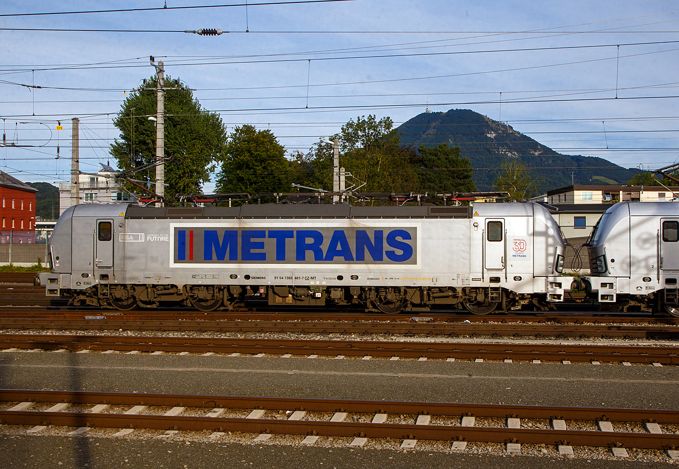 In Doppeltraktion fahren die 383 401-7 (91 54 7383 401-7 CZ-MT) und die 383 407-4 (91 54 7383 407-4 CZ-MT), zwei Siemens Vectron MS der METRANS Rail s.r.o. (Prag / Praha), mit einem Containerzug am 12.09.2022 durch den Hbf Salzburg in Richtung Osten. Die METRANS gibt es schon über 30 Jahren, sie ist ein 100 %-iges Tochterunternehmen der Hamburger Hafen und Logistik AG (HHLA).

Die beiden Siemens Vectron MS (Vectron X4 A01) wurden 2019 von Siemens Mobilitiy in München-Allach gebaut und an die METRANS geliefert. Die 401 unter der Fabriknummer 22688 und die 407 unter der Fabriknummer 22695. Sie sind in der Vectron MS Version A01und haben so die Zulassungen und Zugbeeinflussungssysteme für Tschechien, Deutschland, Österreich, Slowakei, Ungarn und Polen (CZ, D, A, SK, H, PL). Die neuen Lokomotiven für Metrans erreichen eine Höchstleistung von 6,4 MW und eine Spitzengeschwindigkeit von 160 km/h. 

Zukünftige Aufrüstungen für den Einsatz in Bulgarien, Kroatien, den Niederlanden, Rumänien, Serbien und Slowenien sind möglich. 

Für alle Varianten des Vectron hat Siemens ein neues Drehgestell vom Typ SF4 entwickelt. Die einheitlichen Drehgestellrahmen sind so konstruiert, dass entweder ein teilabgefederter Antrieb für Geschwindigkeiten bis 200 km/h oder ein vollabgefederter Antrieb für Geschwindigkeiten bis 230 km/h eingebaut werden kann. Die Fahrmotoren sind dabei elastisch im Drehgestell gelagert und die Kraftübertragung erfolgt über einen Ritzelhohlwellenantrieb. Es besteht die Möglichkeit, zwei verschiedene Bremsausrüstungen zu montieren. Die Drehgestelle dienen zusätzlich als Antennenträger für einige Zugsicherungssysteme. Je nach Kundenwunsch können die Lokomotiven auch mit dem „aktiven Drehfederdämpfer“ (ADD) ausgerüstet werden. Diese Einrichtung steuert aktiv den Ausdrehwinkel des Drehgestells mit. So wird auch ein optimaler Kraftschluss zwischen Rad und Schiene gewährleistet.

TECHNISCHE DATEN:
Hersteller: Siemens Mobilitiy in München-Allach
Herstellerbezeichnung: Vectron X4 A01
Spurweite: 1.435 mm
Achsanordnung: Bo’Bo’
Fahrzeugbegrenzungslinie: UIC 505-1
Länge über Puffer: 18 980 mm
Breite: 3 010 mm
Fahrzeughöhe: 3 860 mm
Drehzapfenabstand: 9 500 mm
Achsabstand im Drehgestell: 3 000 mm
Treibraddurchmesser: 1 250 mm (neu) / 1170 mm (abgenutzt)
Dienstgewicht: 89 t
Dauerleistung: 6 400 kW, bei 3 kV DC  6 000 kW
Höchstgeschwindigkeit: 160 km/h
Maximale Anzugsfahrkraft: 300 kN
Elektrische Bremskraft: 150 kN
Stromsystem:  25 kV 50 Hz/ 15 kV 16,7 Hz und 3 kV DC
Kleinster befahrbarer  Gleisbogenradius: R 80 m  
Bremse: KE-GPR-E mz