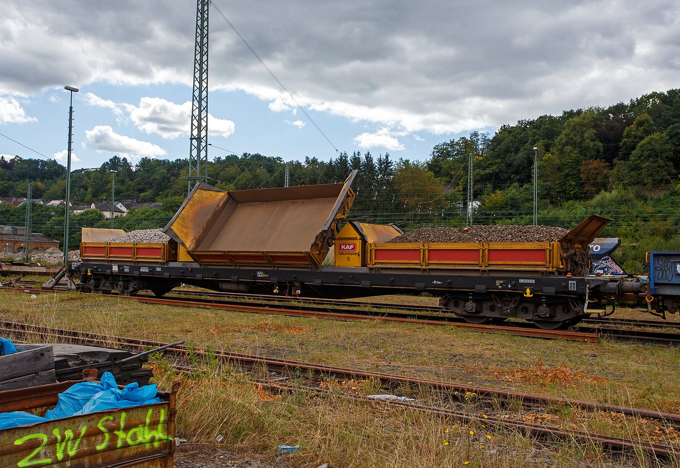 Kippwagen MK 45 DH „LW-Kipper“, 37 80 3832 020-6 D-KAF, der Gattung Rlps, der KAF Falkenhahn Bau AG, Kreuztal (ehemaliger Wagen der Leonhard Weiss) abgestellt am 24 August 2025 in Betzdorf/Sieg.

Der von LEONHARD WEISS entwickelte Kippwagen MK 45 DH „LW-Kipper“, ist für den offenen Transport von losen, nicht zu verwehenden Schüttgütern vorgesehen. Dank der niedrigen Bauweise ist die Beladung unter abgeschalteten Oberleitungen gefahrlos möglich. Die Ladekante ist 2.049 mm über Schienenoberkante. Der speziell ausgebildete Bediener ist für das Entladen rechts und links vom Gleis verantwortlich. Jeder Wagen ist mit einer eigenständigen Hydraulikanlage ausgestattet, welche von einem Kubota 3-Zyl. Dieselmotor angetrieben wird. So braucht man keine Fremdenergie, wie Strom oder Druckluft von der Lok.

Es wird jeweils eine Mulde pro Wagen gekippt. Es können bis zu 10 Kippwagen miteinander gekoppelt und über ein ansteckbares Bedienpult gemeinsam gesteuert werden. Die Standsicherheit ist in üblichen Überhöhungen und Radien durch eine intelligente Steuerung jederzeit gewährleistet. Die Entladezeit beträgt ca. 10 Minuten für alle 3 Mulden.

TECHNISCHE DATEN:
Gattung: Rlps
Spurweite: 1.435 mm (Normalspur)
Achsanzahl: 4 (in zwei Drehgestellen)
Länge über Puffer: 20.740 mm
Drehzapfenabstand: 15.700 mm
Achsabstand im Drehgestell: 1.800 mm
Eigengewicht: 34.450 kg
Max Zuladung: 45,5 t ab Streckenklasse C (8,5 m³)
Muldenmaß (L x B x H): 5.000 x 2.480 x 520 mm
Höchstgeschwindigkeit: 100 km/h (leer und beladen)
Bremse: KE-GP-A (max. 68 t)
Kleister befahrbarer Gleisbogen: R = 60 m, (Arbeit R =150 m)
Internationales Profil: G1
Intern. Verwendungsfähigkeit:  RIV

Kippaggregat: Wassergekühlter 3-Zyl. Dieselmotor Kubota D 1105 mit zwei Hydraulikpumpen und Überdruckventil
Motor-Leistung: 18,5 kW (24,8 PS)
Motor-Hubraum 1.123 l (Bohrung Ø 78 mm x 78,4 mm Hub)
Tankkapazität: 120 l Diesel
Hydr. Tankkapazität: 140 l Panolin HLP 46
Höhe über Schienenoberkante in Transportstellung: 2.690 mm
Höhe über Schienenoberkante in Kippstellung: 4.009 m
Höhe über Schienenoberkante in Bordwandhöhe: 2.049 mm
Max. Kippwinkel der Mulden: 55°
