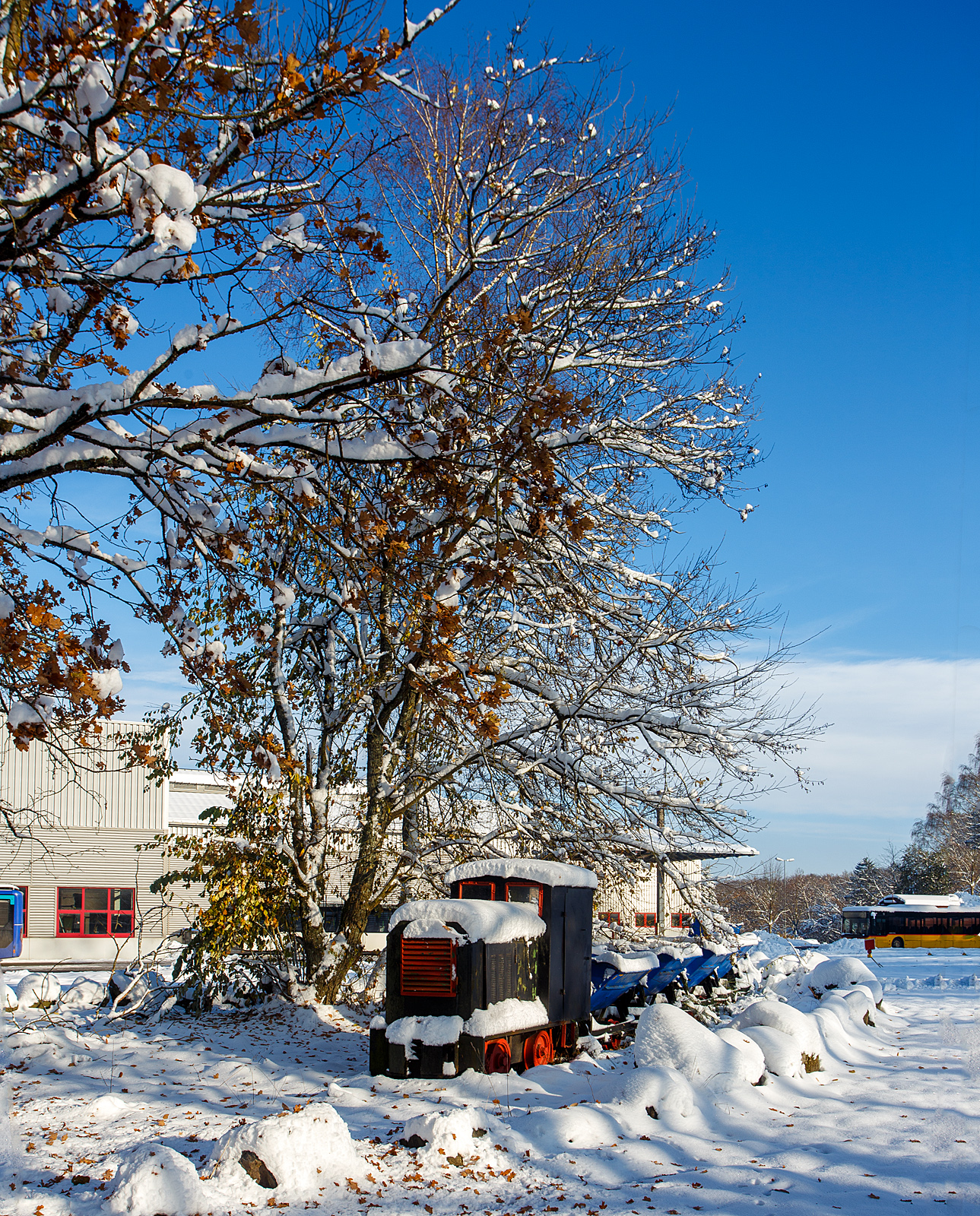 Kleiner 600mm Feldbahn-Kipplore-Zug „ganz groß“ als Denkmal beim Betriebshof der Westerwaldbahn (WEBA), hier am ersten Advent dem 03 Dezember 2023 auf der Bindweide bei Steinebach/Sieg.

Vorne eine 600mm DIEMA Feldbahnlok (Typ und Baujahr sind mir unbekannt), dahinter 5 Kipploren. 

Für den Laien ist alles, was auf der Feldbahn gezogen wird eine Lore. Tatsächlich bezieht sich dieser Ausdruck auf die wohl am weitesten verbreitete Wagenform - eine einfaches Rahmengestell mit zwei Achsen, Pilzkopfkupplungen und kippbarer Mulde. Die Mulden gab es in schmaler Bauform für den beengten Tiefbaubetrieb (Untertage-Bergbau), in breiter Bauform für die Tagebaue, Steinbrüche, Fabrikanlagen, usw.. In dieser Form war dieser Wagentyp in 100.000 und mehr Exemplaren weltweit im Einsatz. Von der Westerwälder Tongrube bis zum Bau der Autobahnen. In den Ausführungen zeigte sich eine kaum zu überblickende Vielfalt.

Diese Kipplore ist in der Bauart Eluco Record, in geschweißter Ausführung: Mulde aus Stahlblech, Abrollwiegen, Schlagleisten und Untergestell aus Profilstahl.
