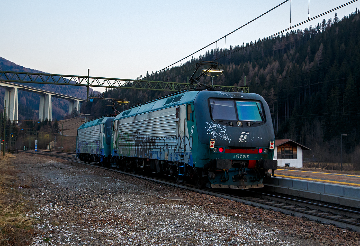 Leider sehr beschmiert....
In Doppeltraktion fahren zwei Brennerloks (ex Trenitalia E.412) am 26.03.2022 als Lokzug vom Brenner hinab kommend durch den Bahnhof Gossensaß/Colle Isarco in Richtung Bozen. Nochmal einen lieben Gruß an den netten Lokführer zurück. Vorne die E412 005 (91 83 2412 005-7 I-MIR) und dahinter die E412 018 (91 83 0412 018-4 I-MIR), beide gehören heute zur Mercitalia Rail Srl., die aber auch eine 100%tige Tochter der Ferrovie dello Stato Italiane (FS, deutsch Italienische Staatseisenbahnen) ist. Sie betreibt heute die Güterverkehrssparte. 

Beide wurden 1997 vom damaligen Hersteller ABB Tecnomasio in Vado Ligure (Italien), später Bombardier, heute Alstom, gebaut und an die Trenitalia S.p.A. geliefert. Die E.412 005 unter der Fabriknummer 7420 und die E.412 018 unter der Fabriknummer 7433. 

Die Brennerloks vom Typ Adtranz 112E sind ähnlich denen später von Bombardier (2001/2) gebauten 8 Loks für die polnische PKP - Polskie Koleje Państwowe vorgesehen EU43 vom Typ Bombardier 112E. Der Verkauf scheitere aus finanziellen Gründen seitens der PKP. Die 8 polnischen Loks sind danach an die italienische Privatbahngesellschaft RTC (Rail Traction Company) verkauft worden, die polnische Bezeichnung EU43 wurde später an Lokomotiven der TRAXX-Variante MS2 vergeben.

Ursprünglich war für beide Baureihen die Zulassung für Österreich und Deutschland vorgesehen. Die ÖBB hatte zunächst die Zulassung verweigert und erst 2006 erteilt.

Geschichte:
Im Jahr 1993 gaben die FS im Zuge der wachsenden internationalen Aktivitäten der europäischen Bahngesellschaften Mehrsystemlokomotiven in Auftrag, die sowohl im italienischen 3-kV-Gleichstromnetz als auch im Süden von Frankreich (1,5 kV =) und insbesondere für den Brennerverkehr auch im österreichischen und deutschen Netz (15 kV, 16,7 Hz) einsetzbar sein sollte. Die Lokomotiven sollten sowohl für schnelle EuroCity-Züge als auch für den Güterverkehr einsetzbar sein. Die vier Prototyp-Lokomotiven wurden ab 1996 vom damaligen Hersteller ABB Tecnomasio (heute Alstom) in Vado Ligure, Italien, gebaut. Dieses Werk produziert nahezu ausschließlich für den italienischen Markt. 

Technik:
Die Lokomotiven laufen auf Drehgestellen mit Integriertem Gesamtantrieb (IGA), der auch bei den Lokomotiven der DB-Baureihe 101 und den italienischen E405 vorhanden ist, die Stromrichter ähneln denen der SBB Re 460. Für den Antrieb werden Doppelsternmotoren verwendet, was Drehstrom-Asynchronmotoren mit zwei Wicklungssystemen in Sternschaltung im selben Gehäuse sind – eine eher unübliche Schaltung.

Der geschweißte Wagenkasten in Stahlleichtbaukonstruktion stützt sich über Flexicoil-Schraubenfedern auf die Drehgestelle ab. Die Seitenwände aus Aluminium sind zur Erhöhung der Steifigkeit gesickt. Der estergekühlte Transformator ist wie bei Neubaulokomotiven üblich unterflur angeordnet. Die Lokomotive ist mit Gruppenantrieb ausgeführt, wobei eine Antriebsgruppe aus einer Achse aus dem Drehgestell 1 und einer aus dem Drehgestell 2 besteht, eine ebenfalls unübliche Anordnung.

Die Lokomotiven verfügt über eine elektrische Nutzbremse. Es sind zwei Einholmstromabnehmer der Bauart WBL 85 vorhanden, je einer für Gleichspannung (Führerstand A, italienische Palette) und Wechselspannung (Führerstand B, deutsch-österreichische Palette).

In der Lokomotive sind zwei Stromrichter angeordnet. Unter Wechselstromsystemen wird die sekundärseitige Spannung des Haupttransformators in einem Vierquadrantensteller (4QS) in eine Gleichspannung umgewandelt, welche in einen Gleichstromzwischenkreis eingespeist wird. Unter den Gleichstromsystemen erfolgt die Speisung des Zwischenkreises direkt aus der Fahrleitung.

Die Pulswechselrichter wandeln den Gleichstrom des Zwischenkreises in Dreiphasenwechselstrom zur Speisung der Fahrmotoren um. Im Gleichstromnetz sind zwei Pulswechselrichter in Serie geschaltet, die je ein Wicklungssystem der Fahrmotoren mit Strom versorgen, im Wechselstromsystem wird nur ein Pulswechselrichter benötigt, der die beiden parallel geschalteten Wicklungssysteme der Fahrmotoren mit Spannung versorgt.

Die Steuerung der Antriebe erfolgt durch ein rechnerunterstütztes Betriebssystem. Die Lokomotiven sind mit 18-poligen IS-Steckdosen für die UIC-Leitung, einer Vielfachsteuerung und einer Speiseeinrichtung der Zugsammelschiene für Reisezüge ausgerüstet. Lauftechnisch sind die Lokomotiven für eine Geschwindigkeit von 220 km/h ausgelegt, jedoch in Italien nur für 200 km/h zugelassen. Ausgerüstet wurden sie mit Fahrzeugeinrichtungen der Zugbeeinflussungen RS4 Codici (Italien) sowie punkt- und linienförmiger Zugbeeinflussung (Österreich und Deutschland). Von einem Einsatz in Frankreich wurde abgesehen.

Die E 412 wurden mit dem damals üblichen XMPR-Anstrich der FS ausgeliefert, werden seit 2021 aber im Rahmen von Hauptuntersuchungen auf den neuen rot-grauen Anstrich der FS-Tochter Mercitalia Rail umlackiert.

TECHNISCHE DATEN:
Spurweite:  1.435 mm (Normalspur)
Achsformel: Bo'Bo'
Länge: 19.400 mm
Drehzapfenabstand: 11.400mm
Achsabstand im Drehgestell: 2.650 mm
Dienstgewicht: 88 t
Höchstgeschwindigkeit: 150 km/h Italien / 140 km/h Deutschland / 120 km/h Österreich
Dauerleistung: 5.600 kW (15 kV AC) / 5.400 kW (3 kV DC) / 2.700 kW (1,5 kV DC)
Anfahrzugkraft: 280 kN
Stromsysteme: 15 kV, 16,7 Hz AC, 3.000 V DC und 1.500 V DC 
Anzahl der Fahrmotoren:  4× IGA-Drehstrom-Asynchronmotoren
Bremse: Druckluftbremse, el. Nutzbremse
Zugbeeinflussung: RS 4 Codici, PZB, LZB