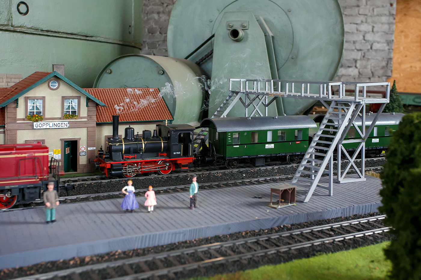 Lokschuppenfest der WEF - Westerwälder Eisenbahnfreunde 44 508 e. V. am 07 Juli 2024 in Westerburg. Im Lokschuppen gibt es eine Spur 1-Modelbahnanlage um einen Kohlekran herum. Hier erreicht gerade die DR 98 7505, ex Bayern 853, ex. K.Bay.Sts.B. 853  EURYDICE , mit ihrem Lokalbahnzug den Bahnhof Göpplingen (Fantasienamen von PIKO). 

Dies Spur 1 Lok, das Original, eine Bayerische D VI Lokalbahnlokomotive, gibt es heute leider nicht mehr (wurde 1936 ausgemustert), aber ich will gerne doch beschreiben:
Die Dampflokomotive wurde 1880 von der  Lokomotiv- und Maschinenfabrik J. A. Maffei in München unter der Fabriknummer 1233 gebaut und als K.Bay.Sts.B. 853  EURYDICE  an die Königlich Bayerischen Staatseisenbahnen geliefert. Ab April 1920 wurde sie als DR Bayern 853 der Reichseisenbahnen des Deutschen Reiches, Gruppenverwaltung Bayern bezeichnet, ab August 1924 als DRG 853 der Deutsche Reichsbahn-Gesellschaft bezeichnet und zum 30.05.1925 wurde sie zur DR 98 7505. Im Jahr 1936 wurde sie dann ausgemustert, der Verbleib ist unbekannt. 

Die Bayerische D VI:
Die Lokomotiven der Gattung D VI waren leichte, zweigekuppelte Nassdampf-Tenderlokomotiven der Königlich Bayerischen Staatseisenbahnen Maffei lieferte 1880 bis 1883 die ersten 30 Lokomotiven, 23 weitere lieferte Krauss bis 1894. Die Lokomotiven wurden für flachere Lokalbahnstrecken mit einer höchstzulässigen Radsatzfahrmasse von 12 t beschafft. Die ersten 44 Lokomotiven hatten noch keine seitlichen Vorratsbehälter. Das Wasser war in einem Rahmenwasserkasten untergebracht, die Kohle im Führerhaus. Die letzten neun Lokomotiven hingegen wurden mit kurzen Vorratsbehältern beidseitig vor dem Führerhaus gefertigt. Damit vergrößerten sich dann der Wasservorrat von 1,8 auf 2,3 m² und der Kohlenvorrat von 0,5 auf 0,8 t.

Die Deutsche Reichsbahn übernahm 1925 als Baureihe 9875 noch 26 Fahrzeuge, davon fünf mit seitlichen Vorratsbehältern. 

Die Lokomotive Nr. 83 „Berg“ (98 7508), 1883 durch Krauss geliefert, war zuletzt in einem Torfwerk in Raubling eingesetzt und ist erst 1964 aus dem Dienst geschieden. Diese Maschine ist als einziges Exemplar ihrer Baureihe erhalten geblieben und befindet sich in der Obhut der DGEG im Eisenbahnmuseum Neustadt/Weinstraße.

Konstruktive Merkmale:
Die Lokomotiven D VI wurde mit einem genieteten und zugleich als Wasserkasten ausgestalteten Blechrahmen ausgeführt. Den Langkessel nietete man aus zwei Schüssen, die Feuerbüchse mit quadratischem Querschnitt ordnete man zwischen den Rahmenwangen an. Zur Kesselspeisung wurden zwei Dampfstrahlpumpen vorgesehen.

Das außenliegende Zweizylinder-Nassdampftriebwerk wurde mit einer Stephenson-Steuerung ausgerüstet, als Treibachse wählte man den zweiten Radsatz.

Erstmals bei bayerischen Lokomotiven wurden bei der D VI Umlaufbleche und Saugluftbremsen des Typs Hardy, teilweise aber auch Westinghouse-Druckluftbremsen eingesetzt. Einige Exemplare verfügten überdies über Übergangsbrücken, ungewöhnlich war seinerzeit die Anordnung der Sandkästen unterhalb des Laufblechs zwischen den Kuppelachsen.

TECHNISCHE DATEN:
Gebaute Anzahl: 53
Hersteller: Krauss (30 Stück), Maffei (26 Stück)
Baujahre: 1880 bis1894
DR-Nummerierungen: DR 98 7501–7526
Spurweite:  1435 mm (Normalspur)
Bauart:  B n2t
Länge über Puffer:  6.860/6.910 mm
Leergewicht: 14,2 t
Dienstgewicht: 18,5 t
Höchstgeschwindigkeit: 45 km/h
Treibraddurchmesser:  1.006 mm (neu)
Zylinderanzahl: 2
Zylinderdurchmesser:  266 mm
Kolbenhub: 508 mm
Kesselüberdruck: 12 bar
Anzahl der Heizrohre:  72
Heizrohrlänge: 2.500 mm
Rostfläche:  0,75 m²
Strahlungsheizfläche: 3,03 m²
Rohrheizfläche: 22,68 m²
Verdampfungsheizfläche: 25,71 m²
Wasservorrat: 1,8 m³ (spätere 2,3 m³)
Kohlvorrat: 0,5 t (spätere 0,8 t)
Lokbremse: Hardy-Saugluftbremse (z. T. Druckluftbremse)
Steuerung:  Außenliegende Stephenson-Steuerung mit Flachschiebern

Quellen: wikipedia.org, dampflokomotivarchiv.de, albert-gieseler.de