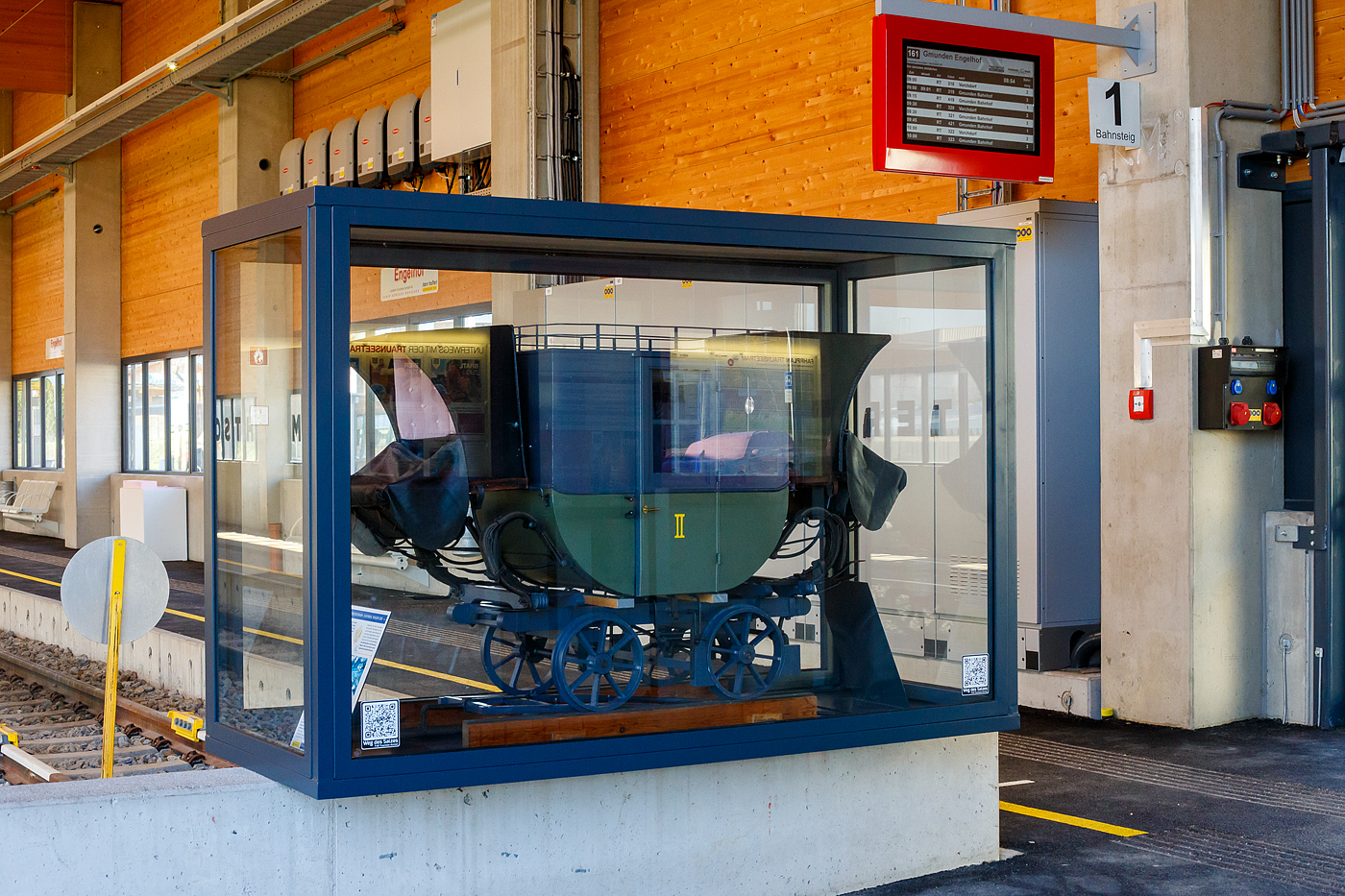 Nein keine Postkusche, sondern ein Modell von einem Personenwagen der 2. Klasse  Hannibal  der der Budweis-Linz-Gmundener Pferdeeisenbahn, hier auf einem Schleppwechsel (Weiche) dieser Bahn stehend. Ausgestellt im Bahnhof Engelhof der Traunseetram (Lokalbahn Gmunden–Vorchdorf), hier am 04 April 2025. 

Das heute noch erhaltene Bahnhofsgebäude Engelhof hat von 1836 bis 1855 als Stationsplatz Englhof mit Pferdeställen der Pferdeeisenbahn gedient. Nach 1855 wurde der Bahnhof von der inzwischen längst eingestellten Linie Gmunden–Laakirchen–Lambach genutzt. Heute nutzt ihn noch die Traunseebahn (Lokalbahn Gmunden–Vorchdorf) als Bahnhof. Der denkmalgeschützte Bahnhof Engelhof ist der älteste noch in Funktion stehende Bahnhof Kontinentaleuropas!

Ein erhaltenes Original von einem dieser 1941 in Linz-Urfahr gebauten Hannibal-Waggon steht heute im Technischen Museum Wien. Mit der Einstellung der Linz Budweiser Pferdeeisenbahn am 15. Dezember 1872 wurde der Wagen außer Verwendung gesetzt. Ursprünglich war es ein 1. Klasse Wagen, mit der Umstellung der Südstrecke von Linz nach Gmunden auf Dampfbetrieb in Jahr 1855, und der Anschaffung neuer und komfortablerer Personenwagen, wurden die alten Pferdebahnwagen zur 2. Klasse umgezeichnet. Nach Einstellung der Pferdeeisenbahn 1872, war  Hannibal  ein Glanzstück der Ausstellung über die Verkehrsgeschichte auf der Wiener Weltausstellung 1873. Danach geriet er in einem Schuppen im Prater in Vergessenheit. Nach der Wiener Gewerbeausstellung 1888, wurde er zerlegt am Dachboden der Werkstätten am Westbahnhof gelagert. Dort gingen einige Teile verloren. 1893 fand er einen neuen Platz im k.k. historischen Museums der Österreichischen Staatsbahnen.

Bereits seit Achttausend Jahren wird im Salzkammergut Salz abgebaut und das abgebaute Salz wurde, über 1000 Jahre lang über die Traun (Fluß) befördert. Der Salztransport entlang der Traun, war nicht nur gefährlich, sondern auch teuer. Demnach war der Bau der Pferdeeisenbahn plausibel. Im Jahre 1834 begannen die ersten Bauarbeiten der südlichen Strecke von Linz nach Gmunden, welche bereits nach zwei Jahren abgeschlossen wurden. So war nun die komplette Strecke der Pferdeeisenbahn Budweis–Linz–Gmunden fertig. Sie war nach der 1827 eröffneten Bahnstrecke Saint-Étienne–Andrézieux, die zweite öffentliche Eisenbahnlinie auf dem europäischen Festland und diente hauptsächlich dem Transport von Salz aus dem oberösterreichischen Salzkammergut nach Böhmen (was ja bis 1918 zur Habsburgermonarchie gehörte). 

Die Strecke war in der ungewöhnlichen Spurweite von 1.106 mm (3 österr. Fuß 6 Zoll) ausgeführt. Es waren aber keine Eisenschienen auf denen die Spurkranzräder liefen, sondern Holzschienen (Balken) auf denen Flacheisen mit handgefertigten Nägeln befestigt waren. Die Streckenlänge betrug von Budweis nach Linz 128,8 km und von Linz nach Gmunden 67,9 km, somit fast 200 km. Die Trasse war eingleisig mit zahlreichen Ausweichen ausgeführt.

Die Bahngesellschaft besaß ca. 1000 Güterwagen. Das Ladegewicht betrug 2,5-3,3 t. Zur Beförderung der Fracht verwendete man offene und gedeckte Wagen. Die Hauptfracht Salz wurde mit zweiachsigen, offenen Niederbordwagen, auf denen man rund 40 Fässer mit je 56 kg laden konnte, befördert. Einige Wagen waren für den Kohle-, Steine- und Langholztransport vierachsig. Die Personenwagen wiesen verschiedene Bauarten auf, es gab offene und gedeckte Wagen und hatten bis zu 24 Sitzplätze. Die Wagen waren in drei Klassen unterteilt und trugen Namen.

Gezogen wurden die Wagen meist von einem Pferd, bei steigungsreichen Abschnitten wurde ein zweites Pferd vorgespannt. Zugpferde waren so gut wie ausschließlich Noriker. Der Noriker (auch Pinzgauer) ist ein mittelschweres, kräftiges und ausdauerndes Gebirgskaltblutpferd, die sich als stark und genügsam erwiesen. Die Gesellschaft verfügt im Vollbetrieb über 600 Pferde. Die Geschwindigkeit der Güterzüge betrug im Schnitt 4 km/h, pro Tag wurden maximal 40 Kilometer zurückgelegt. So brauchte ein Güterwagen von Gmunden nach Budweis 5 Tage.

Die Strecke zwischen Linz und Gmunden wurde in den Jahren 1855 und 1856 auf Dampfbetrieb umgestellt. Auf der gebirgigen Strecke zwischen Linz und Budweis (České Budějovice) war diese Umstellung aufgrund zu enger Krümmungsradien und zu großer Steigungen nicht möglich. Bis 1873 wurden daher als Ersatz die Bahnstrecken Linz–Gaisbach-Wartberg und St. Valentin–České Budějovice mit zumeist anderer Trassenführung zwischen Linz und Budweis errichtet, die den Dampfbetrieb zuließ. Der Pferdebahnbetrieb wurde im Dezember 1872 eingestellt.