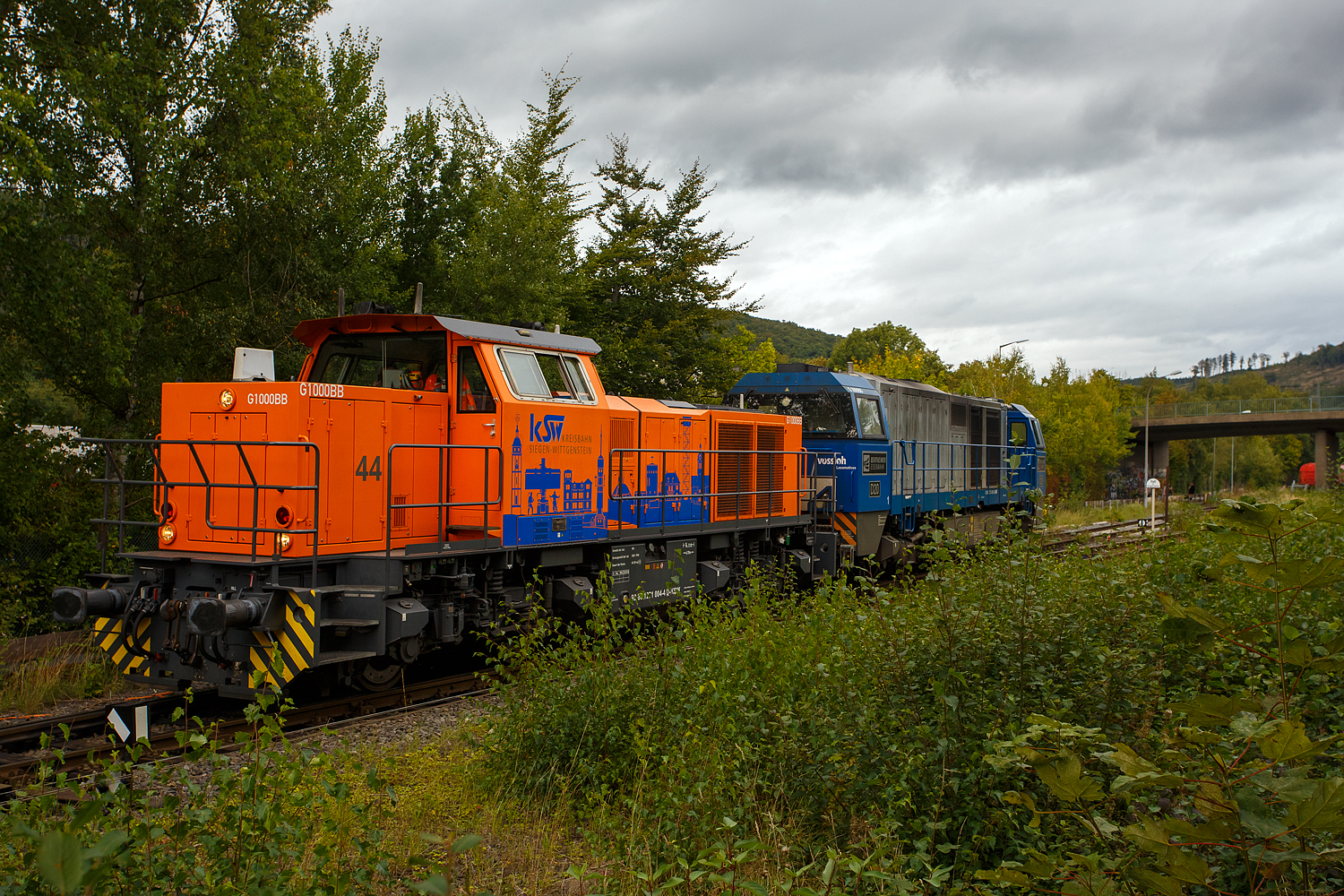 Nun am 18 September 2025 verlassen die KSW 44 (92 80 1271 004-4 D-KSW) eine MaK G 1000 BB und die an die KSW vermietete 272 408-6 / D20 der Bentheimer Eisenbahn AG (92 80 1272 408-6 D-BE), ex Rurtalbahn V 203 (92 80 1272 408-6 D-RTBC), eine Vossloh G 2000BB (mit symmetrischem Führerhaus), beide gemeinsam wieder den KSW-Rangierbahnhof (Betriebsstätte FGE - Freien Grunder Eisenbahn) in Herdorf und fahren über die Hellertalbahn in Richtung Betzdorf/Sieg zurück um neue Aufgaben zu erfüllen. Zuvor hatten sie im Sandwich einen sehr langen und schweren Coilzug nach Herdorf gebracht. Für die weitere Fahrt war dann die KSW 47 zuständig, die den Zug in 2 bis 3 Partien von Herdorf nach Neunkirchen-Salchendorf abfuhr. 