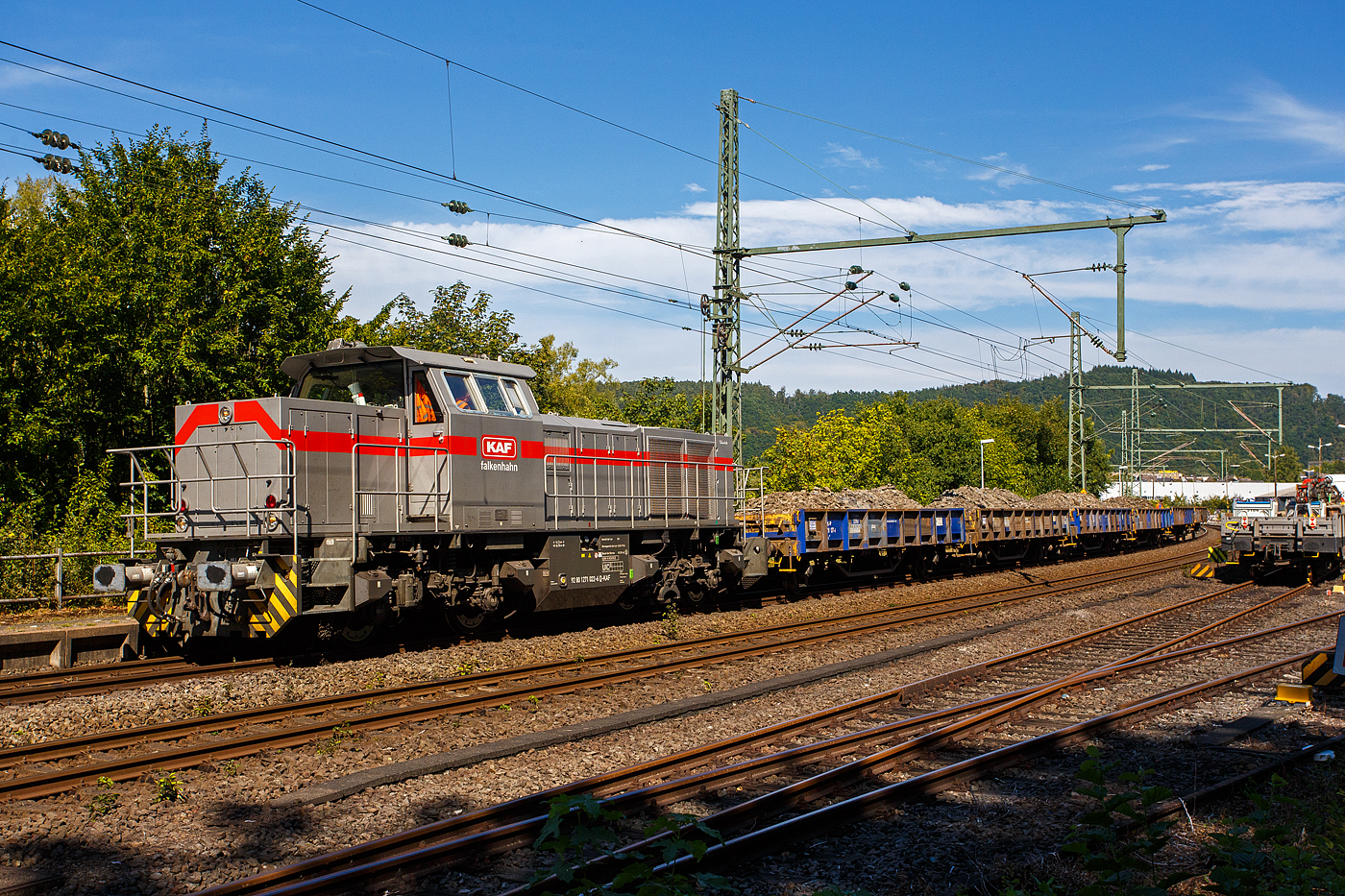 Nun drückt die 271 022-6 „Charlotte“ (92 80 1271 022-6 D-KAF) eine Vossloh/MaK G 1000 BB der KAF Falkenhahn Bau AG. ex MRCE bzw. ex HGK DH 49, am 26 August 2025 den mit Aushub beladenen Niederbordwagen-Zug (zweiachsiger Flachwagen NS Gattung Klmos 702 der Vermietungsfirma Railpro), von der Baustelle im Bf Scheuerfeld/Sieg ca. 3 km nach Betzdorf/Sieg. Beim Rbf Betzdorf befindet sich die Umladestation, hier wird der Aushub von Baggern abgeladen und zwischengelagert. 