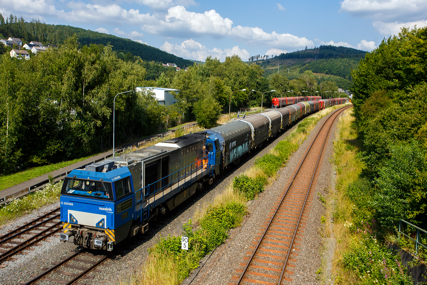 Nun hat der ganze lange Coilzug den KSW-Rangierbahnhof (Betriebsstätte FGE - Freien Grunder Eisenbahn) in Herdorf am 25 Juli 2025 erreicht. Hier am Zugschluss die nachschiebende an die KSW vermietete 272 408-6 / D20 der Bentheimer Eisenbahn AG (92 80 1272 408-6 D-BE), ex Rurtalbahn V 203 (92 80 1272 408-6 D-RTBC), eine Vossloh G 2000BB (mit symmetrischem Führerhaus). Vorne (ganz hinten rechts im Bild) die KSW 44 (92 80 1271 004-4 D-KSW) eine MaK G 1000 BB. Rechts die DB-Strecke KBS 462 „Hellertalbahn“.

Für die Talbahn (Freien Grunder Eisenbahn) zum Pfannenberg ist der Zug einfach zu lang, so wird er hier geteilt und die KSW 44 zieht später 9 oder 10 Wagen weiter zum Pfannenberg. Wobei für die Spitzkehre Pfannenberg ist dann dieser Zug auch nach zu lang und er wird in Neunkirchen-Salchendorf nochmals geteilt. 