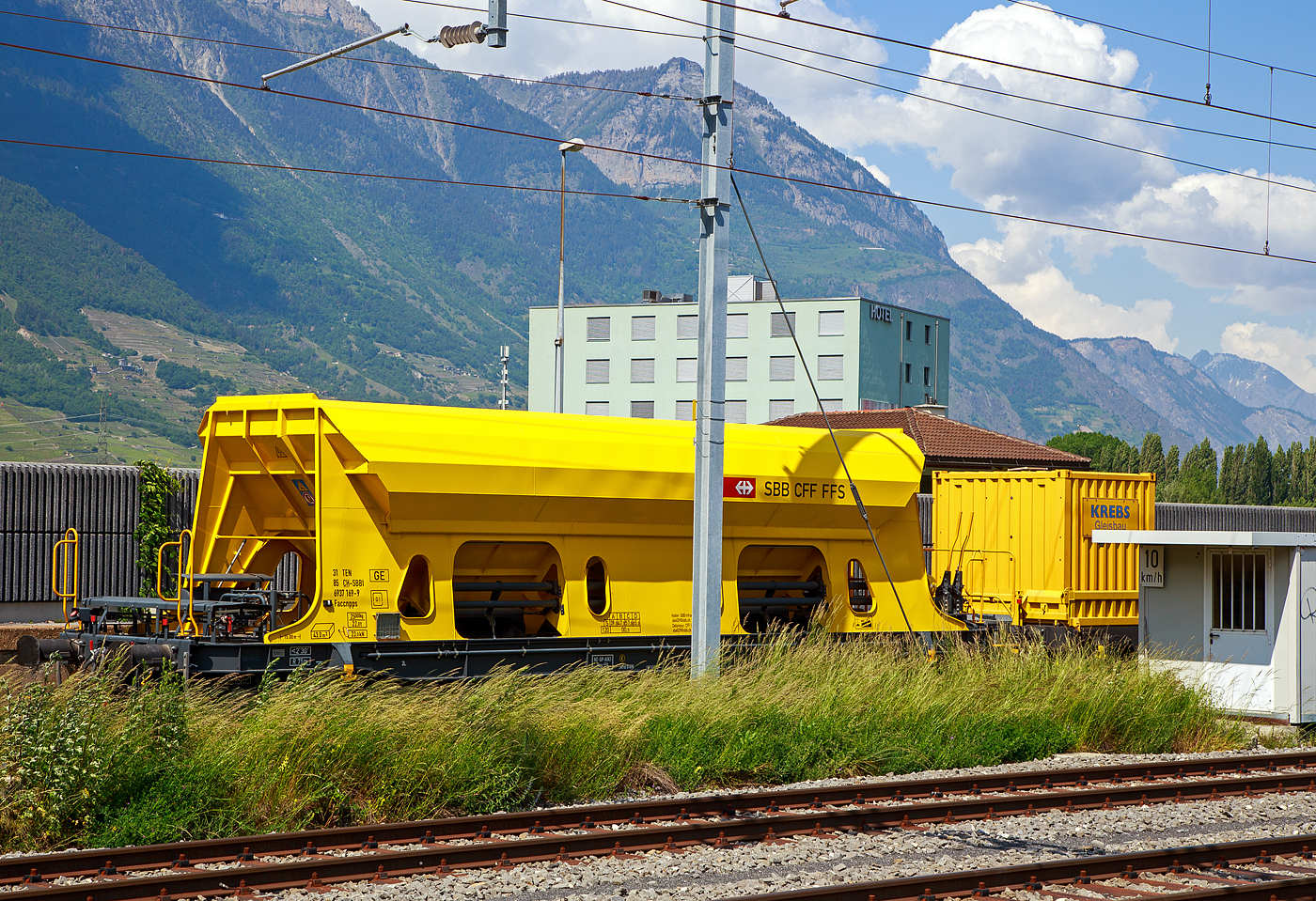 Offener 4-achsiger Drehgestell-Schüttgutwagen mit dosierbarer Schwerkraftentladung 31 85 6937 169-9 der Gattung Faccnpps (Xans) der SBB Infrastruktur abgestellt am 26.05.2023 beim Bahnhof Martigny.

Der Wagen wurde von ´OS Trnava, a. s. in Trnava (Slowakische Republik) gebaut.

Der 4-achsige Selbstentladewagen der Reihe Faccnpps wurde neu entwickelt und so konstruiert, damit er alle neuesten Anforderungen der TSI-Güterwagen, TSI-Lärm und die Anforderungen für den internationalen Transport erfüllt. Er ist für den Transport von lockeren Substraten (gebrochene Steine, Schotter, Makadam ...) bestimmt. Das Entladen erfolgt über Klappen unter Nutzung der Gravitationskraft, inklusive Dosiermöglichkeiten. Die Klappen werden mechanisch von der Wagenbühne aus betätigt, mit der Möglichkeit des Öffnens von vier Klappen (auf jeder Seite des Wagens befinden sich zwei Klappen). Der Wagen besteht aus einem Skelett, einem geschweißten Untergestell, in dem die Zug- und Stoßeinrichtungen sowie die Wagenbremse eingebaut sind. Den Wagenkasten bilden Blechverkleidungen mit den dazugehörigen Querverbindungen und Stützen, Stirnwände, vier Klappen, ein Öffnungsmechanismus zum Öffnen und Schließen der Seitenklappen und ein sattelförmiger Wagenboden. Der Wagen ist mit einem Schutz gegen unbefugtes Betreten der Leiter ausgestattet, sowie mit einer LED-Beleuchtung des Bedienungs- und Entleerungsplatzes, wodurch es möglich ist, den Wagen auch für Arbeiten in der Nacht zu nutzen. Die Hauptzuleitung aus dem Stromnetz für die Einspeisung ist 400 V/16 A gleichgerichtet auf 230 V/12 V.

TECHNISCHE DATEN:
Spurweite: 1.435 mm
Achsanzahl: 4
Länge über Puffer: 15.000 mm
Drehzapfenabstand: 10.200 mm
Achsabstand im Drehgestell: 1.800 mm
Laderaum: 43 m³
Höchstgeschwindigkeit: 100 km/h (beladen) / 120 km/h (leer)
Maximales Ladegewicht: 65,0 t (ab Streckenklasse D)
Eigengewicht: 25.000 kg
Kleinster bef. Gleisbogenradius: 75 m
Bremse: KE-GP-A (K)
Bremssohle: Jurid 816M
Intern. Verwendungsfähigkeit: TEN-GE