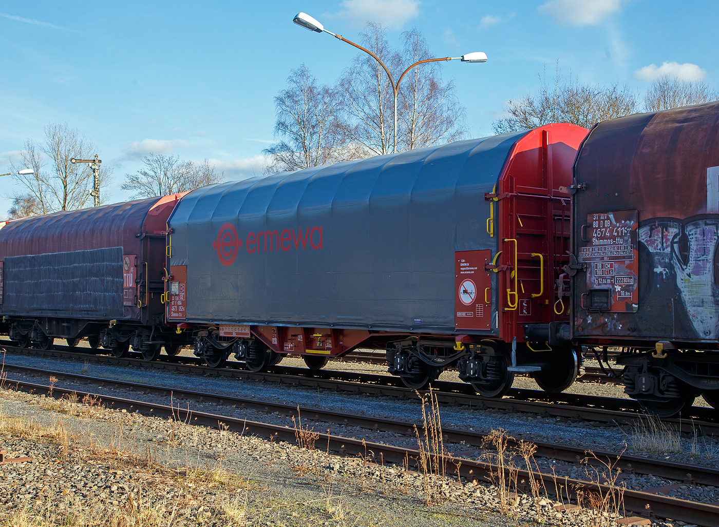 Recht neuer und noch nicht beschmierter, vierachsiger Drehgestell-Flachwagen mit verschiebbarem Planenverdeck und Lademulden für Coil-/Spaltbandtransporte, 33 87 4673 052-6 F-ERSA der Gattung Shimmns-ttu, der französischen Vermietungsfirma ERMEWA S.A., abgestellt am 21.02.2013 im Zugverband, auf dem KSW Rbf in Herdorf (Betriebsstätte Freien Grunder Eisenbahn - NE 447).

Der Wagen wurde vom kroatischen Hersteller Đuro Đaković in Slavonski Brod gebaut. Die Plane mit Spriegel und Laufwagen ist vom Schleswiger Tauwerkfabrik Oellerking GmbH & Co. KG.

Die Ausstattung mit fünf Lademulden sowie das Planverdeck optimieren die Beförderung nässeempfindlicher Coils. Diese Planen können jeweils soweit zusammen geschoben werden, dass zum Be- und Entladen die Ladefläche zu 2/3 freigelegt ist. Der Wagen ist für die Beförderung von schweren witterungsempfindlichen Blechrollen (Coils) mit 5 fest im Untergestell eingebauten Lademulden ausgerüstet.

Das Untergestell und die Stirnwände, die als Abkantrahmenkonstruktion mit Blechbekleidung und U-förmigen Verstärkungsprofilen ausgeführt sind, bilden den Wagenkasten. Die sattelförmig angeordneten, jeweils mit den Außenlangträgern verschweißten Querträger bilden zusammen mit den Muldenblechen die Lademulden. Die Wagenabdeckung erfolgt mit einer PVC-beschichteten Gewebeplane, die auf 11 Rohrrahmen aufliegt. Über Laufwagen ist das Planendach in Wagenlängsrichtung verschiebbar. Die Verriegelung des Planendaches an den Stirnwänden erfolgt über eine 4-PunktZentralverriegelung, die sowohl vom Erdboden als auch von der Rampe aus bedient werden kann. Das Planendach lässt sich an einem Wagenende so weit zusammenschieben, dass ca. 2/3 der Ladefläche zur Beladung freigegeben wird. Zwischen den Spriegeln sind Hilfsspriegel so angeordnet, dass ein Einfallen der Plane beim Zusammenschieben um die Hälfte vermindert wird, um den notwendigen Freiraum für größere Coildurchmesser zu gewährleisten. Der Wagen darf nur mit geschlossenem und verriegeltem Planendach verkehren.

Die Wagen sind mit 20 verstellbaren Festlegearmen (4 je Mulde) ausgerüstet, die auf den Muldenhöckern gelagert sind und sich über Rollen in den Mulden abstützen. Ihre Form und Festigkeit ist so ausgelegt, dass sie einen sicheren Schutz gegen unzulässiges seitliches Verschieben als auch gegen Kippen gebundener Schmalbandcoils (Spaltband) gewährleisten. Gegenüber Festlegeeinrichtungen früherer Bauarten (z. B. Shimmns-tu 718) sind die einzelnen Arme sowohl grob verschiebbar als auch über Spindeln fein einstellbar. Dadurch können die Arme bis auf Kontakt an die Coils herangeführt werden. Die Spindeln werden dazu über seitlich an den Muldensätteln angeordnete Handräder oder auch über geeignete Maschinen angetrieben. Die Auskleidung der Mulden mit einer Gummiauflage soll einen optimalen Schutz des Coilbleches, der auch durch eine spezielle Muldenkonstruktion erreicht wird, unterstützen. Im Wageninneren sind auf Piktogrammen Beladehinweise und -schemen angebracht.

TECHNISCHE DATEN:
Spurweite: 1.435 mm
Achsanzahl: 4 (in 2 Drehgestelle)
Länge über Puffer: 12.040 mm
Länge der Ladefläche: 10.795 mm
Ladebreite (Mulden): 2.410 mm
Drehzapfenabstand: 7.000 mm
Achsabstand im Drehgestell: 1.800 mm
Drehgestell-Bauart: Y 25Ls1(K)
Laufraddurchmesser: 920 mm (neu)
Eigengewicht:  21.880 kg
Höchstgeschwindigkeit: 100  km/h (beladen) / 120 km/h (leer)
Maximales Ladegewicht: 68,1 t (ab Streckenklasse D4)
Kleinster bef. Gleisbogenradius: 35 m
Bauart der Bremse: KE-GP-A (K)
Bremssohle: Cosid 810
Intern. Verwendungsfähigkeit: TEN-GE

Die Bedeutung der Gattungs- und Kennbuchstaben (hier Shimmns-ttu):
S - Drehgestellflachwagen in Sonderbauart
h - für den Transport von Blechrollen, liegend verladen, eingerichtet
i - mit beweglicher Abdeckung und festen Stirnwänden
mm - mit vier Radsätzen Ladelänge unter 15 m, bei sechs unter 18 m
n - höchste Lastgrenze über 60 t
s - Höchstgeschwindigkeit 100 km/h (beladen)
-ttu - 	Mit besonderer, stufenlos verstellbarer Festlegeeinrichtung zum Sichern gebündelter Schmalbandcoils und Auskleidung der Mulden mit gewebeverstärkten Gummimatten.
