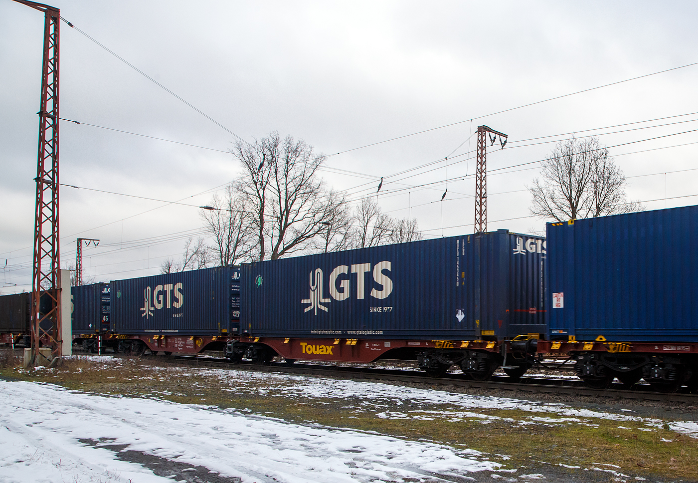 Sechsachsige Drehgestell-Gelenk-Containertragwagen-Einheit (6-achsiger Containertragwagen), 33 85 4962 219-4 CH-TOUAX, der Gattung Sggmrss 90', der irischen Vermietungsfirma Touax Rail Limited, am 27.01.2023 im Zugverband bei der Durchfahrt in Rudersdorf (Kr. Siegen), hier beladen mit zwei Containern.

TECHNISCHE DATEN:
Spurweite: 1.435 mm
Anzahl der Achsen: 6 in drei Drehgestellen
L�nge �ber Puffer: 29.590 mm
Drehzapfenabstand: 2 x 11.995 mm
Achsabstand im Drehgestell: 1.800mm
Laufraddurchmesser: 920 mm (neu)
Ladel�nge : 2 x 13.820mm  (2 x 45 ft)
H�he der Ladeebene �ber SOK: 1.155 mm
Eigengewicht: ca. 28.000 kg
Max. Zuladung bei Lastgrenze S: 107,0 t (ab Streckenklasse D)
Max. Zuladung bei Lastgrenze SS: 92,0 t (ab Streckenklasse C)
Max. Geschwindigkeit: 100 km/h (Lastgrenze SS oder leer 120 km/h)
Kleinster bef. Gleisbogenradius: R 75 m
Verwendungsf�higkeit: TEN-GE