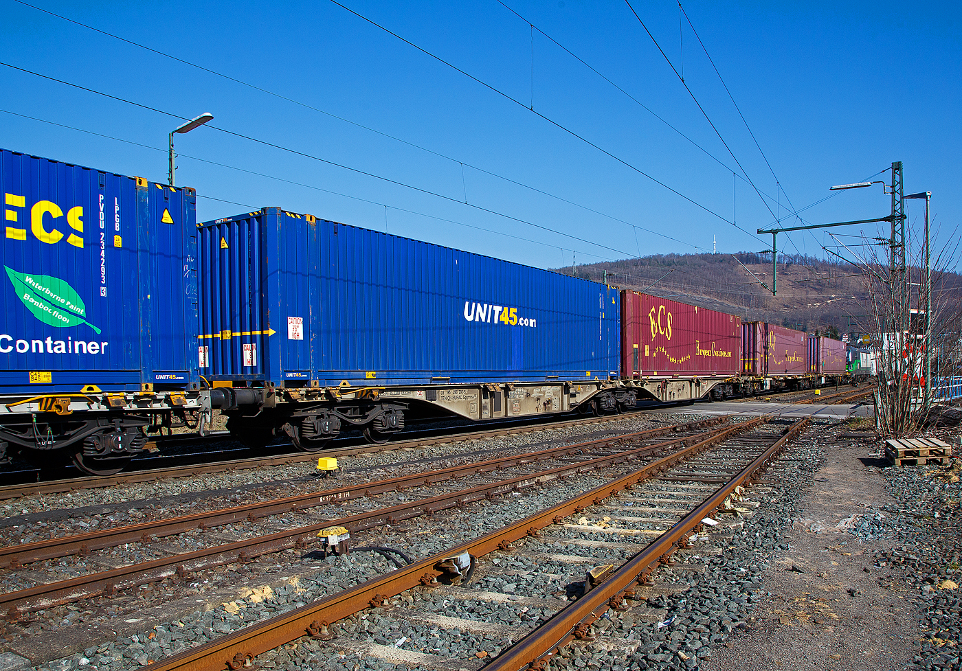 Sechsachsiger Drehgestell-Gelenk-Containertragwageneinheit 90´, 33 85 4961 290-5 CH-HUPAC der Gattung Sggmrss 90`der HUPAC AG am 24.03.2021 im Zugverband bei der Durchfahrt in Niederschelden an der Siegstrecke (KBS 460) in Richtung Siegen.

Diese Gelenkwagen mit sechs Radsätzen sind für den Transport von Großcontainern und Wechselbehältern vorgesehen. Auf den Außenlangträger des Wagens befinden sich für jede vorgesehene Ladeposition feste und klappbare Aufsetzzapfen zum Festlegen der Ladungseinheiten (gemäß UIC- Merkblatt 592-1 und 2) in verschiedenen Kombinationen.

Das aus zwei Wagenhälften bestehende Untergestell ist eine verwindungsweiche, geschweißte Rahmenkonstruktion aus Walz- und Blechprofilen, gebildet aus den Kopfstücken, den Hauptquerträgern und den äußeren Langträgern. In der Wagenmitte befindet sich eine Übersteigmöglichkeit.

TECHNISCHE DATEN:
Spurweite: 1.435 mm
Länge über Puffer: 29.590 mm
Drehzapfenabstand: 2 x 11.995 mm
Achsabstand in den Drehgestellen: 1.800 mm
Drehgestelle: 3 x Y25Lss1-K
Laufraddurchmesser: 920 mm (neu)
Ladelänge: 2 x 13.820 mm
Höhe der Ladeebene über S.O.: 1.155 mm
Eigengewicht: 27.400 kg
Max. Zuladung bei Lastgrenze S: 107,6 t (ab Streckenklasse D)
Max. Zuladung bei Lastgrenze SS: 92,6 t (ab Streckenklasse C)
Max. Geschwindigkeit: 100 km/h (Lastgrenze SS und leer 120 km/h)
Kleinster befahrbarer Gleisbogen: R 75 m 
Bremse: 2 x KE-GP-A 
Bremssohle: Jurid 816M
Feststellbremse: Ja
Verwendungsfähigkeit: TEN GE