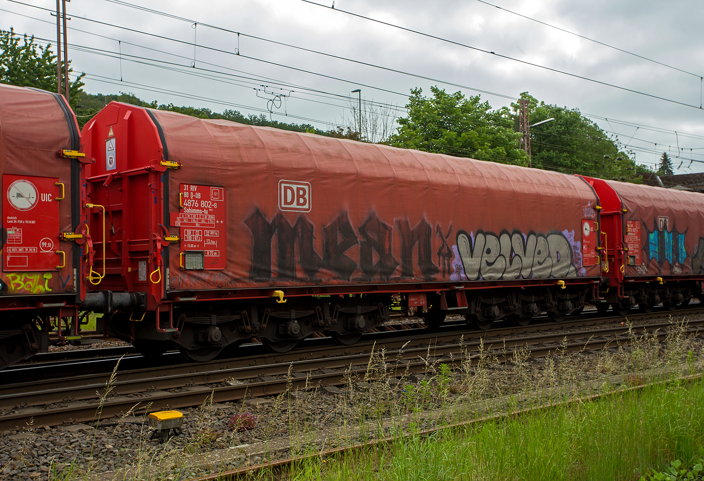 Sechsachsiger Drehgestellflachwagen mit verschiebbarem Planenverdeck und Lademulden für Coiltransporte, 31 80 4876 802-8  D-DB der Gattung Sahimms-tu 900.2, der DB Cargo AG, am 03 Juni 2024 in Kreuztal, eigereiht im Zugverband. Leider beschmiert, wie viele solcher Wagen. 

Der Wagen ist für die Beförderung von schweren witterungsempfindlichen Blechrollen bestimmt. Dieser Spezialwagen besitzt Stirnwände und fünf fest im Untergestell eingebaute Mulden. Die Wagenabdeckung erfolgt mit einer PVC-beschichteten Gewebeplane, die auf 14 Rohrrahmen aufliegt. Zwei auf dem Außenlangträger aufgeständerte Laufschienen dienen als Rollenbahn für mehrere abhebesichere Laufwagen, welche über die Querspriegel mit dem Planendach verbunden sind und dieses somit in Wagenlängsrichtung verschiebbar machen. Die Verriegelung des Planendaches an den Stirnwänden erfolgt über eine Zentralverriegelung, die vom Erdboden aus bedient werden kann. Das Planenverdeck lässt sich an einem Wagenende so weit aufschieben, dass ca. 2/3 der Ladefläche zur zum Be- und Entladen freigegeben werden. Zur Fixierung der Laufwagen des Planenverdecks in der geöffneten Stellung sind an den Endspriegelwagen Festlegeeinrichtungen montiert.

Der Wagen besitzt insgesamt fünf feste Mulden, wobei die beiden äußeren Mulden Coils mit einem Gewicht von maximal 25 t und einem maximalen Durchmesser von 2.250 mm, die mittleren drei Mulden Coils mit maximal 45 t Gewicht bei einem maximalen Durchmesser von 2.700 mm aufnehmen können.

Erstes Baujahr der z VEB Niesky. Z. ältesten Wagen war 1984. Hersteller dieser Wagen waren u.a, LHB - Linke-Hofmann-Busch GmbH in Salzgitter, die Waggonfabrik Talbot in Aachen, O&K - Orenstein & Koppel AG in Dortmund-Dorstfeld und die VEB Waggonbau Niesky (DDR). 

TECHNISCHE DATEN:
Gattung: Sahimms-tu 900.2
Spurweite: 1.435 mm
Achsenanzahl: 6 (in 2 Drehgestelle)
Länge über Puffer: 15.000 mm
Drehzapfenabstand: 8.000 mm
Achsabstand im Drehgestell: 3.400 mm (2 x 1.700 mm)
Laufraddurchmesser: 920 mm (neu)
Eigengewicht: 32.300 kg
Höchstgeschwindigkeit: 100 km/h (beladen) / 120 km/h (leer)
Maximales Ladegewichte: 87,5 t (Streckenklasse CE)
Maximale Tragfähigkeit: 99,5 t
Kleinster bef. Gleisbogenradius: 75 m
Bauart der Bremse: KE-GP (IP 116)
Intern. Verwendungsfähigkeit: RIV
Hersteller der Plane: Schleswiger Tauwerkfabrik Oellerking GmbH & Co. KG
