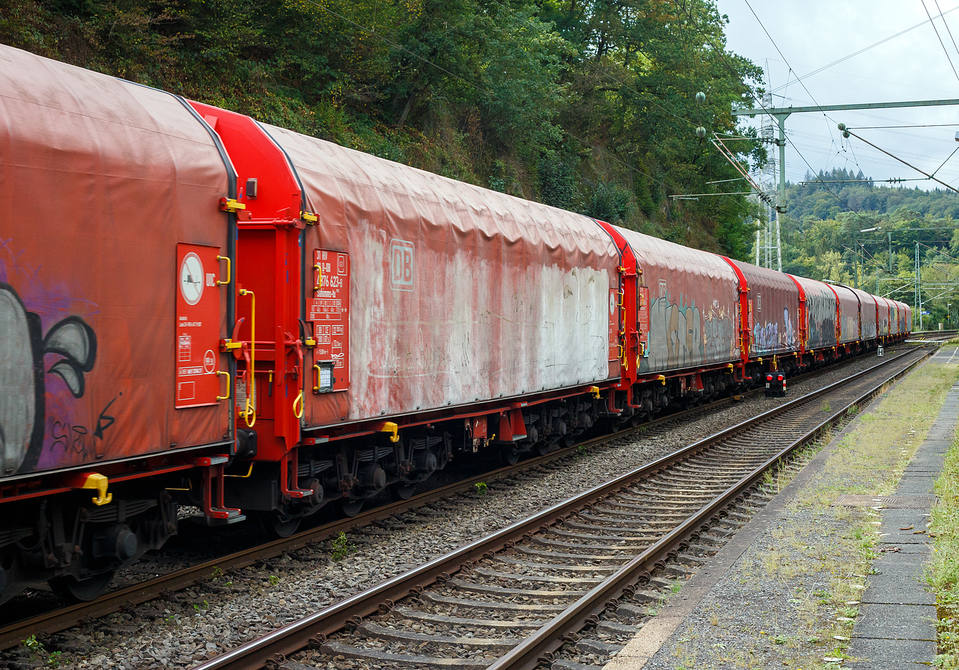 Sechsachsiger Drehgestellflachwagen mit verschiebbarem Planenverdeck und Lademulden für Coiltransporte, 31 80 4876 623-8 D-DB der Gattung Sahimms-tu 900.2, der DB Cargo AG, am 11 September 2024 im Zugverband bei einer Zugdurchfahrt in Scheuerfeld (Sieg). Leider beschmiert, wie viele solcher Wagen.

Der Wagen ist für die Beförderung von schweren witterungsempfindlichen Blechrollen bestimmt. Dieser Spezialwagen besitzt Stirnwände und fünf fest im Untergestell eingebaute Mulden. Die Wagenabdeckung erfolgt mit einer PVC-beschichteten Gewebeplane, die auf 14 Rohrrahmen aufliegt. Zwei auf dem Außenlangträger aufgeständerte Laufschienen dienen als Rollenbahn für mehrere abhebesichere Laufwagen, welche über die Querspriegel mit dem Planendach verbunden sind und dieses somit in Wagenlängsrichtung verschiebbar machen. Die Verriegelung des Planendaches an den Stirnwänden erfolgt über eine Zentralverriegelung, die vom Erdboden aus bedient werden kann. Das Planenverdeck lässt sich an einem Wagenende so weit aufschieben, dass ca. 2/3 der Ladefläche zur zum Be- und Entladen freigegeben werden. Zur Fixierung der Laufwagen des Planenverdecks in der geöffneten Stellung sind an den Endspriegelwagen Festlegeeinrichtungen montiert.

Der Wagen besitzt insgesamt fünf feste Mulden, wobei die beiden äußeren Mulden Coils mit einem Gewicht von maximal 25 t und einem maximalen Durchmesser von 2.250 mm, die mittleren drei Mulden Coils mit maximal 45 t Gewicht bei einem maximalen Durchmesser von 2.700 mm aufnehmen können.

Erstes Baujahr der z.Z. ältesten Wagen war 1984. Hersteller dieser Wagen waren u.a, LHB - Linke-Hofmann-Busch GmbH in Salzgitter, die Waggonfabrik Talbot in Aachen, O&K - Orenstein & Koppel AG in Dortmund-Dorstfeld und die VEB Waggonbau Niesky (DDR).  

TECHNISCHE DATEN:
Gattung: Sahimms-tu 900.2
Spurweite: 1.435 mm (Normalspur)
Achsenanzahl: 6 (in 2 Drehgestelle)
Länge über Puffer: 15.000 mm
Drehzapfenabstand: 8.000 mm
Achsabstand im Drehgestell: 3.400 mm (2 x 1.700 mm)
Laufraddurchmesser: 920 mm (neu)
Eigengewicht: 32.300 kg
Höchstgeschwindigkeit: 100 km/h (beladen) / 120 km/h (leer)
Maximales Ladegewichte: 87,5 t (Streckenklasse CE)
Maximale Tragfähigkeit: 99,5 t
Kleinster bef. Gleisbogenradius: 75 m
Bauart der Bremse: KE-GP (LL)
Bremssohle: IP 116
Handbremse: nein
Intern. Verwendungsfähigkeit: RIV
Hersteller der Plane: Schleswiger Tauwerkfabrik Oellerking GmbH & Co. KG

Die Bedeutung der Gattungs- und Kennbuchstaben (hier Sahimms-tu):
S - Drehgestellflachwagen in Sonderbauart
a - mit sechs Radsätzen (2 Drehgestelle mit je 3 Radsätzen)
h - für den Transport von Blechrollen, liegend verladen, eingerichtet
i - mit beweglicher Abdeckung und festen Stirnwänden
mm – mit sechs o. mehr Radsätzen Ladelänge 18 m bis unter 22 m
s - Höchstgeschwindigkeit 100 km/h (beladen)
-tu - Mit besonderer Festlegeeinrichtung zum Sichern gebündelter
Schmalbandcoils und Auskleidung der Mulden mit gewebeverstärkten Gummimatten
