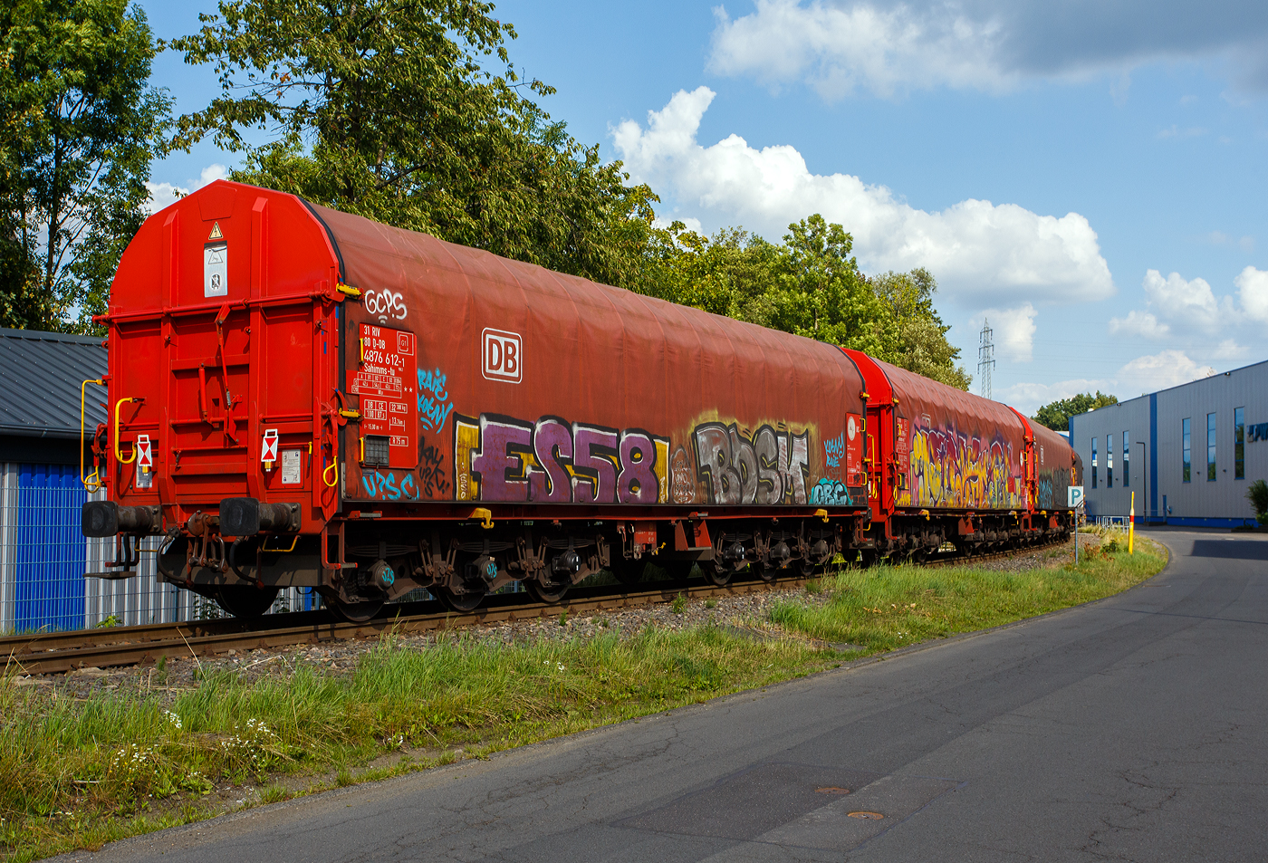 Sechsachsiger Drehgestellflachwagen mit verschiebbarem Planenverdeck und Lademulden für Coiltransporte, 31 80 4876 612-1 D-DB der Gattung Sahimms-tu 900.2, der DB Cargo AG, am 25 Juli 2025 im Zugverband bei der Zugdurchfahrt in Neunkirchen-Struthütten auf der Talbahn (KSW-Strecke, Betriebsstätte FGE - Freien Grunder Eisenbahn) in Richtung Pfannenberg. Leider ist der Wagen wie viele solcher Wagen beschmiert. 

Der Wagen ist für die Beförderung von schweren witterungsempfindlichen Blechrollen bestimmt. Dieser Spezialwagen besitzt Stirnwände und fünf fest im Untergestell eingebaute Mulden. Die Wagenabdeckung erfolgt mit einer PVC-beschichteten Gewebeplane, die auf 14 Rohrrahmen aufliegt. Zwei auf dem Außenlangträger aufgeständerte Laufschienen dienen als Rollenbahn für mehrere abhebesichere Laufwagen, welche über die Querspriegel mit dem Planendach verbunden sind und dieses somit in Wagenlängsrichtung verschiebbar machen. Die Verriegelung des Planendaches an den Stirnwänden erfolgt über eine Zentralverriegelung, die vom Erdboden aus bedient werden kann. Das Planenverdeck lässt sich an einem Wagenende so weit aufschieben, dass ca. 2/3 der Ladefläche zur zum Be- und Entladen freigegeben werden. Zur Fixierung der Laufwagen des Planenverdecks in der geöffneten Stellung sind an den Endspriegelwagen Festlegeeinrichtungen montiert.

Der Wagen besitzt insgesamt fünf feste Mulden, wobei die beiden äußeren Mulden Coils mit einem Gewicht von maximal 25 t und einem maximalen Durchmesser von 2.250 mm, die mittleren drei Mulden Coils mit maximal 45 t Gewicht bei einem maximalen Durchmesser von 2.700 mm aufnehmen können.

Erstes Baujahr der z.Z. ältesten Wagen war 1984. Hersteller dieser Wagen waren u.a, LHB - Linke-Hofmann-Busch GmbH in Salzgitter, die Waggonfabrik Talbot in Aachen, O&K - Orenstein & Koppel AG in Dortmund-Dorstfeld und die VEB Waggonbau Niesky (DDR). Ursprünglich waren die Wagen mit verschiebbaren Teleskophauben ausgeführt, ab 2018 wurden sie in Wagen mit verschiebbarem Planenverdeck umgebaut.

TECHNISCHE DATEN:
Gattung: Sahimms-tu 900.2
Spurweite: 1.435 mm (Normalspur)
Achsenanzahl: 6 (in 2 Drehgestelle)
Länge über Puffer: 15.000 mm
Drehzapfenabstand: 8.000 mm
Achsabstand im Drehgestell: 3.400 mm (2 x 1.700 mm)
Laufraddurchmesser: 920 mm (neu)
Eigengewicht: 32.300 kg
Höchstgeschwindigkeit: 100 km/h (beladen) / 120 km/h (leer)
Maximales Ladegewicht: 72,5 (ab Streckenklasse D3) / DB 87,5 t (ab CE)
Maximale Tragfähigkeit: 99,5 t
Kleinster bef. Gleisbogenradius: 75 m
Bauart der Bremse: KE-GP (LL)
Bremssohle: IP 116
Handbremse: nein
Intern. Verwendungsfähigkeit: RIV / G1
Hersteller der Plane: Schleswiger Tauwerkfabrik Oellerking GmbH & Co. KG
