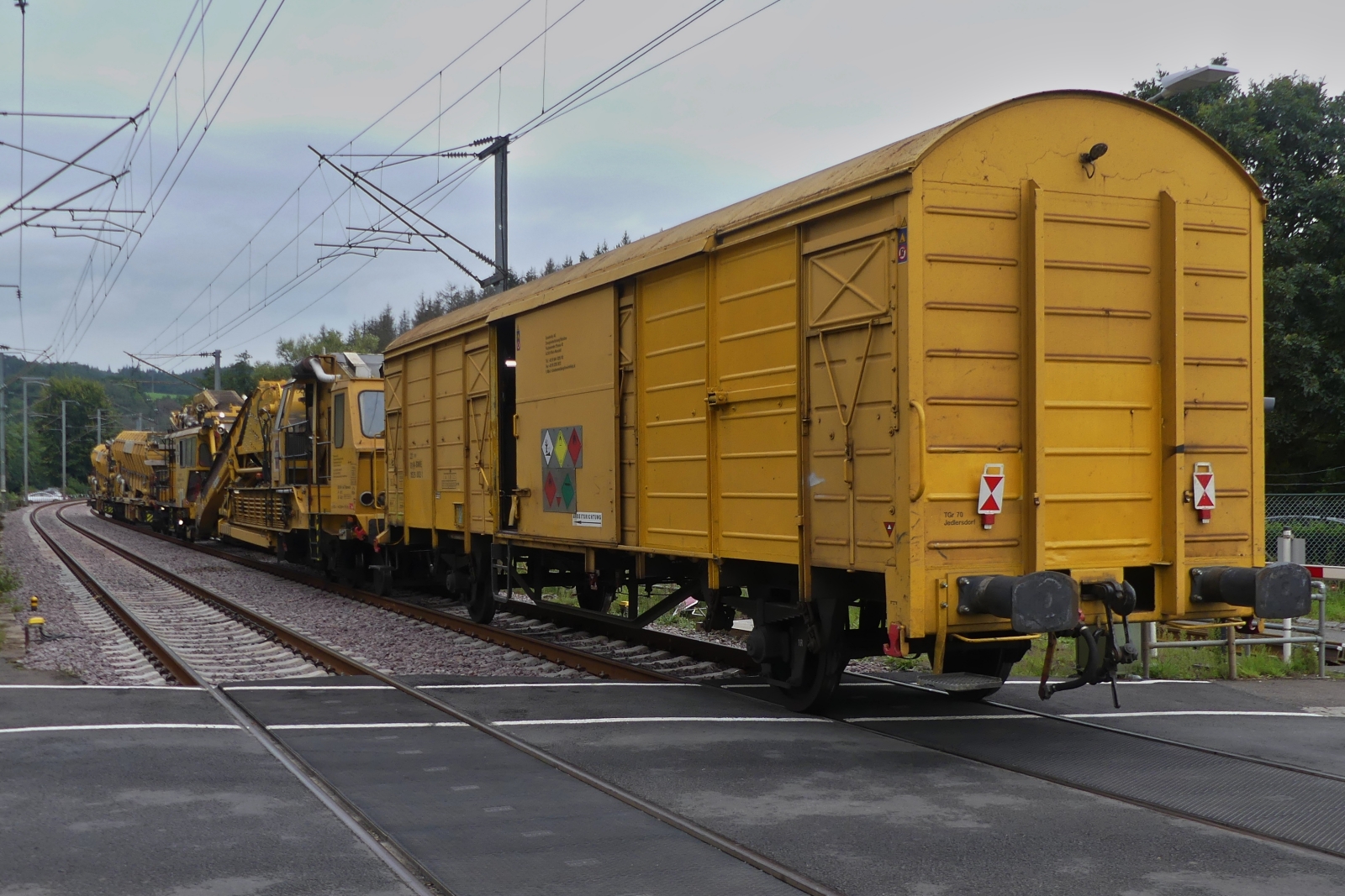 Swietelsky Schotterbettreinigungsmaschine RM 80-92 (9981 9414 001-3) schiebt die Schottersammelwagen im Schneckentempo über den Bahnübergang in Enscherange.  25.08.2023