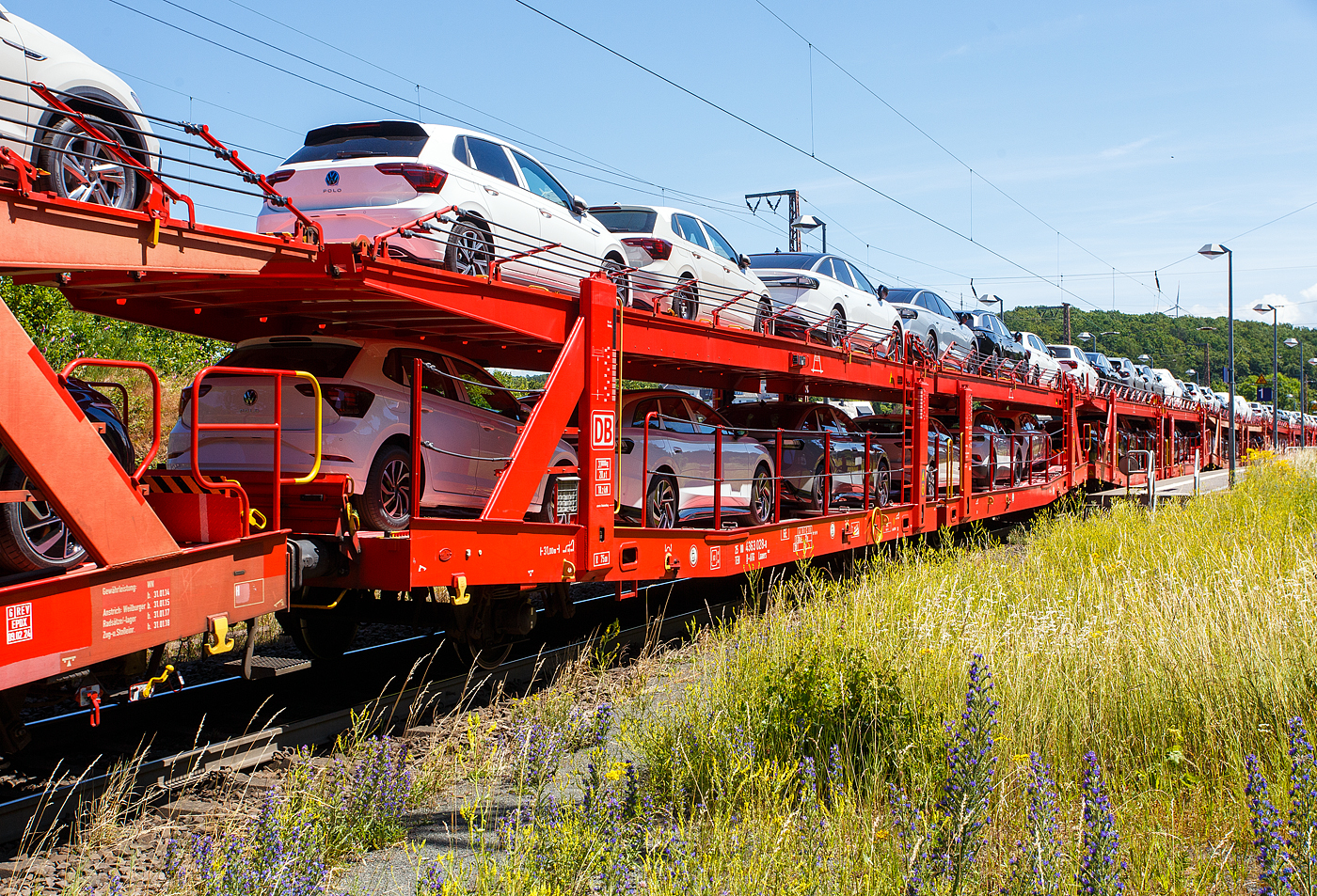 Vierachsiger (2 x zweiachsiger) Doppelstock-Autotransportwagen, 25 80 4363 028-8 D-ATG, der Gattung Laaers 560.2, der DB Cargo Logistics GmbH (ex DB Schenker ATG) am 28 Juni 2024 im Zugverband bei der Zugdurchfahrt in Rudersdorf (Kreis Siegen), hier beladen mit VW PKW´s aus der „Stadt des KdF-Wagens bei Fallersleben“ (ab 1945 Wolfsburg).

Der Wagen wurde 201_ von der damaligen DB Waggonbau Niesky GmbH gebaut.

Diese Waggons haben zwei Ladeebenen und sind für den europaweiten Transport geeignet. Sie werden für den internationalen Transport von PKWs, SUVs und Vans eingesetzt und bieten maximale Flexibilität durch eine stufenlos verstellbare obere Ladeebene. Aufgrund der hohen Lastgrenze (bis 34 t) ist der Transport von besonders schweren Fahrzeugen der genannten Typen möglich.

Damit sowohl ein typenreiner Transport als auch eine Mischverladung in den unterschiedlichen Lademaßen möglich ist, kann die obere Ladeebene hinsichtlich der Transportstellungen stufenlos eingestellt werden.

Durch die Entwicklung eines veränderten Ladungssicherungssystems wurde den Kundenanforderungen nach optimierten Transportmöglichkeiten für Fahrzeuge mit niedrigerer Bodenfreiheit Rechnung getragen.

TECHNISCHE DATEN:
Gattung: Laaers (Bauart 560.2)
Erstes Baujahr der Wagengattung: 2007
Spurweite: 1.435 mm
Anzahl der Achsen: 4 (2 x 2)
Länge über Puffer : 31.000 mm
Achsabstände: 10.000 mm / 5.160 mm / 10.000 mm
Laufraddurchmesser (neu): äußere 840 mm und mittlere 730 mm
Ladelänge : 30.070 mm (unten) / 30.550 mm (oben)
Ladelänge waagerechter Teil untere Ebene: 19.400 mm
Ladebreite : 2.950 (unten) / 2.750 mm (oben)
Höchstgeschwindigkeit: 100 km/h (120 km/h leer)
Eigengewicht: 30.500 kg
Max. Zuladung bei Lastgrenze S: 33,5 t (ab Streckenklasse B, bei A 32,0 t)
Max. Zuladung der Ladeebenen: unten und oben jeweils max. 18 t
Max. Gewicht je Pkw: 2.800 kg (Radlast max. 1 t)
Anzahl der Radvorleger: 64
Höhe Geländer oben: 600 mm
Kleinster befahrb. Gleisbogenhalbmesser: 75 m
Bremse: KE-GP-A (K)
Bremssohle: Jurid 816 M
Handbremse: Ja
Intern. Verwendungsfähigkeit: TEN-GE

Der große Unterschied zwischen den Laaers-Wagen der Bauart 560.2 (wie hier) und der Bauart 560.1 sind das Lastgrenzenraster (Max. Zuladung), zudem ist die Bauart 560.2 meist 500 kg leichter. 