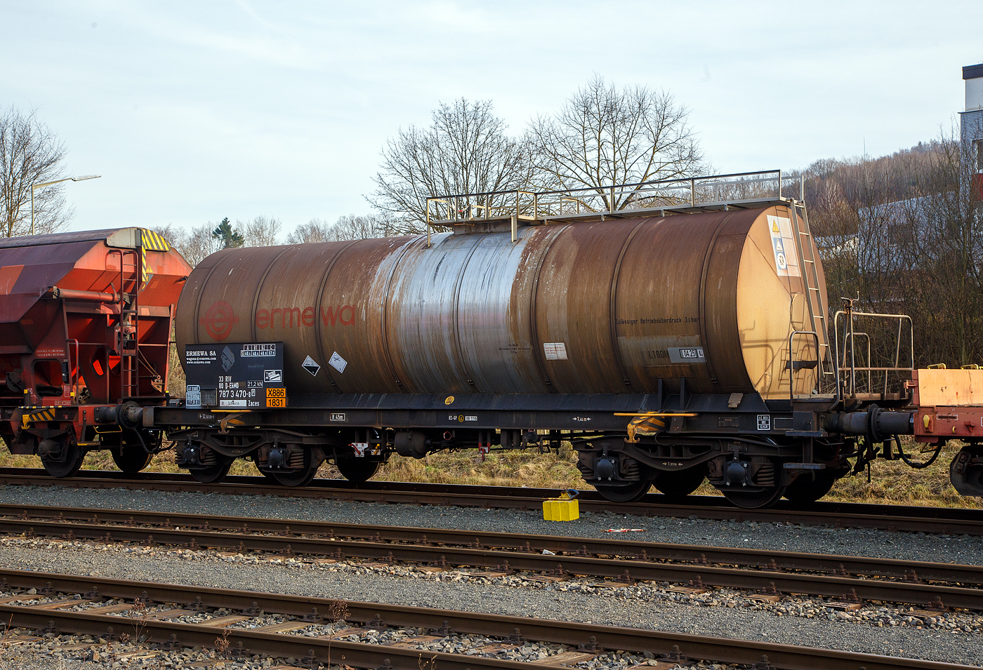 Vierachsiger 41 m� Drehgestell Kesselwagen mit Bremserb�hne, 33 80 7873 470-8 [P] D-ERMD, der Gattung Zaces,  der franz�sischen Vermietungsfirma ERMEWA S.A., abgestellt am 09.02.2023 in Herdorf, im Zugverband eines �bergabezuges der KSW, auf dem Rbf. der KSW. 

Die Gefahrguttafel (X886/1831) zeigt an, was drin war oder ist:
Schwefels�ure (rauchend), auch bekannt als Oleum oder Vitriol (rauchend). Sie wird unteranderem zur Herstellung von Sprengstoffen verwendet, was hier der Fall ist.

TECHNISCHE DATEN:
Gattung: Zaces 
Spurweite: 1.435 mm
L�nge �ber Puffer : 12.500 mm
Drehzapfenabstand: 7.460 mm
Achsabstand im Drehgestell: 1.800 mm
Laufraddurchmesser:  920 mm (neu)
H�chstgeschwindigkeit: 100 km/h
Eigengewicht: 22.050 kg
Max. Ladegewicht: 57,9 t (ab Streckenklasse C)
Kleinster befahrbarer Gleisbogen: R 45 m
Gesamtvolumen: 41.330 Liter (41 m�)
Bauart der Bremse: KE-GP (LL)
Bremssohle: IP 116
Handbremse: Ja
Pr�fdruck: 4 bar
Zul�ssiger Betriebs�berdruck: 3 bar
Tankcode: L10DH
Beh�lterwerkstoff : Edelstahl
Intern. Verwendungsf�higkeit: RIV
