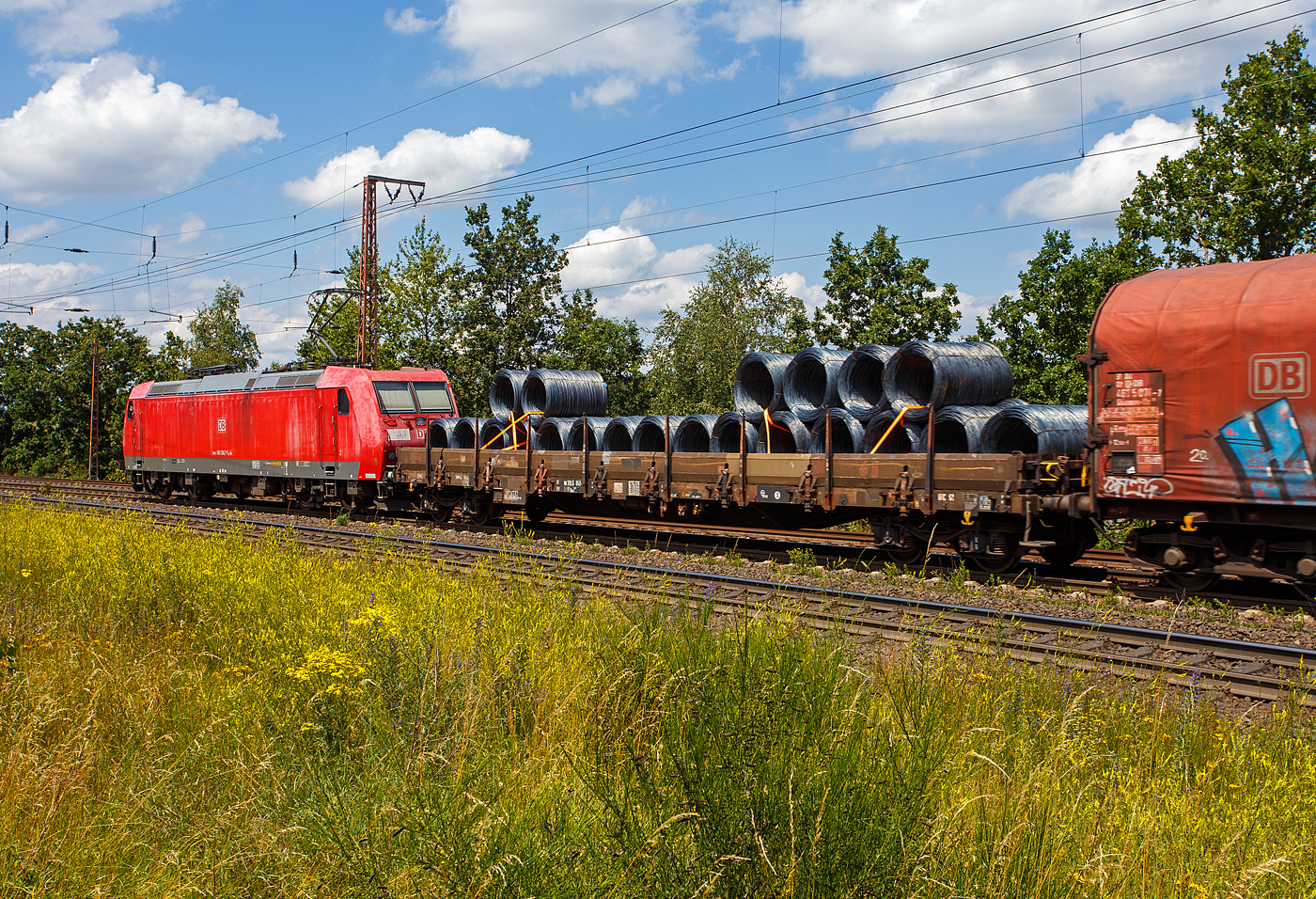 Vierachsiger Drehgestell-Flachwagen, mit Seiten-, Stirnwandklappen und Rungen, 31 80 3945 043-x D-DB, der Gattung Res 687, der DB Cargo, am 11 Juni 2024 im Zugverband bei einer Zugdurchfahrt durch Rudersdorf (Kreis Siegen) in Richtung Siegen bzw. Kreuztal. Hier beladen mit Drahtringen.

Davor die 185 062-7 (91 80 6185 062-7 D-DB) eine Bombardier TRAXX F140 AC1 der DB Cargo.