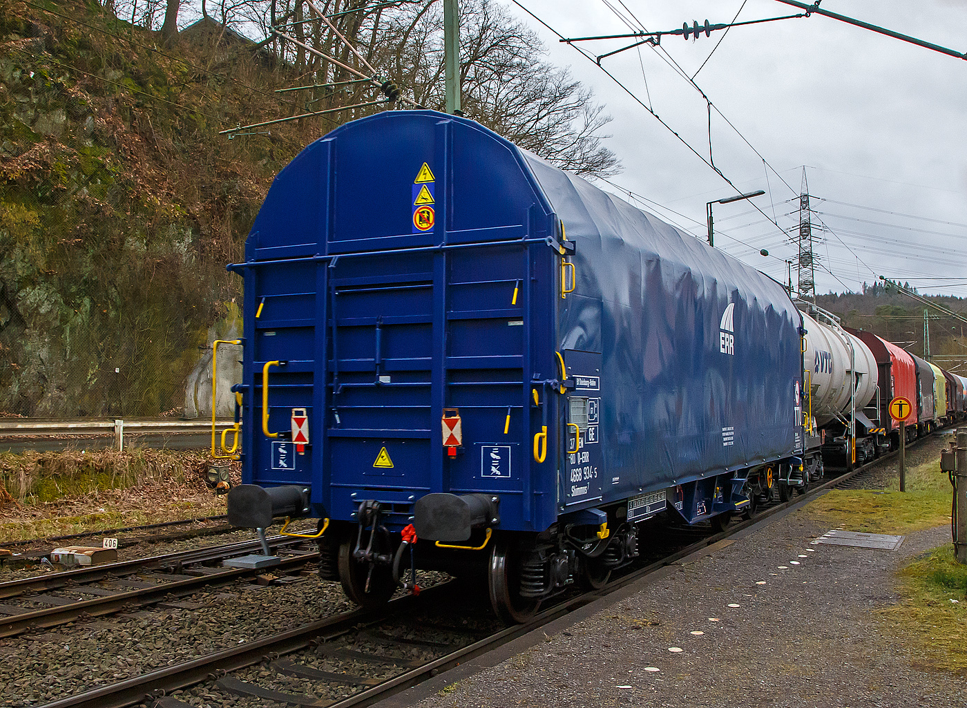 Vierachsiger Drehgestell-Flachwagen mit verschiebbarem Planenverdeck und Lademulden für Coiltransporte, 37 80 4668 934-5 D-ERR, der Gattung Shimmns7 (-ttu), der ERR European Rail Rent GmbH, am 18.02.2023 im Zugverband bei einer Zugdurchfahrt in Scheuerfeld (Sieg).

Diese Wagen sind speziell für den Transport witterungsempfindlicher Blechrollen (Coils) bestimmt. Er besitzt feste Stirnwände, 5 fest im Untergestell eingebaute Lademulden. Die Wagenabdeckung erfolgt mit einer PVC-beschichteten Gewebeplane, die auf 11 Rohrrahmen aufliegt. Über Laufwagen ist das Planendach in Wagenlängsrichtung verschiebbar. Die Verriegelung des Planendaches an den Stirnwänden erfolgt über eine 4-Punkt-Zentralverriegelung, die sowohl vom Erdboden als auch von der Rampe aus bedient werden kann. Das Planenverdeck lässt sich an einem Wagenende so weit zusammenschieben, dass ca. 2/3 der Ladefläche zur Beladung freigegeben wird. Hierdurch ist eine einfache Beladung des Wagens sowohl von oben als auch von der Seite aus möglich. 

TECHNISCHE DATEN:
Spurweite: 1.435 mm
Achsanzahl: 4 (in 2 Drehgestelle)
Länge über Puffer: 12.040 mm
Länge der Ladefläche: 10.800 mm
Drehzapfenabstand: 7.000 mm
Achsabstand im Drehgestell: 1.800 mm
Eigengewicht:  ca. 22 t
Höchstgeschwindigkeit: 100 km/h (beladen) / 120 km/h (leer)
Maximales Ladegewicht: 68 t (ab Streckenklasse D4)
Kleinster bef. Gleisbogenradius: 35 m
Bauart der Bremse: KE-GP-A (K)
Bremssohle: C 810
Intern. Verwendungsfähigkeit: TEN – GE