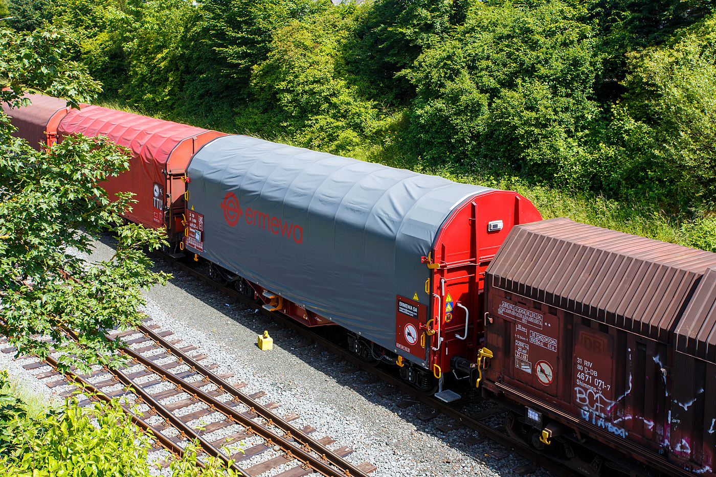 Vierachsiger Drehgestell-Flachwagen mit verschiebbarem Planenverdeck und Lademulden f�r Coil-/Spaltbandtransporte, 33 87 4669 621-4 F-ERSA der Gattung Shimmns, der franz�sischen Vermietungsfirma ERMEWA S.A., abgestellt am 13 Juni 2024 im Zugverband, auf dem KSW Rbf in Herdorf (Betriebsst�tte Freien Grunder Eisenbahn - NE 447).

Die Ausstattung mit f�nf Lademulden sowie das Planverdeck optimieren die Bef�rderung n�sseempfindlicher Coils (Blechrollen/aufgewickeltes kalt gewalztes Blech). Diese Planen k�nnen jeweils soweit zusammen geschoben werden, dass zum Be- und Entladen die Ladefl�che zu 2/3 freigelegt ist. Der Wagen ist f�r die Bef�rderung von schweren witterungsempfindlichen Blechrollen (Coils) mit 5 fest im Untergestell eingebauten Lademulden ausger�stet.

Die Lademulden k�nnen wie folgt belegt werden:
Lademulden 1 und 5 f�r �1.000 mm bis 2.250 mm mit je max. 34 t
Lademulden 2 und 4 f�r � 800 mm bis 1.700 mm mit je max. 17 t
Lademulden 3 f�r � 1.000 mm bis 2.700 mm mit max. 45 t

TECHNISCHE DATEN:
Spurweite: 1.435 mm
Achsanzahl: 4 (in 2 Drehgestelle)
L�nge �ber Puffer: 12.040 mm
L�nge der Ladefl�che: 10.800 mm
Drehzapfenabstand: 7.000 mm
Achsabstand im Drehgestell: 1.800 mm
Laufraddurchmesser: 920 mm (neu)
Eigengewicht:  21.600 kg
H�chstgeschwindigkeit: 100  km/h (beladen) / 120 km/h (leer)
Maximales Ladegewicht: 68,4 t (ab Streckenklasse D4)
Kleinster bef. Gleisbogenradius: 35 m
Bauart der Bremse: KE-GP-A (K)
Bremssohle: Cosid 810
Intern. Verwendungsf�higkeit: TEN-GE
