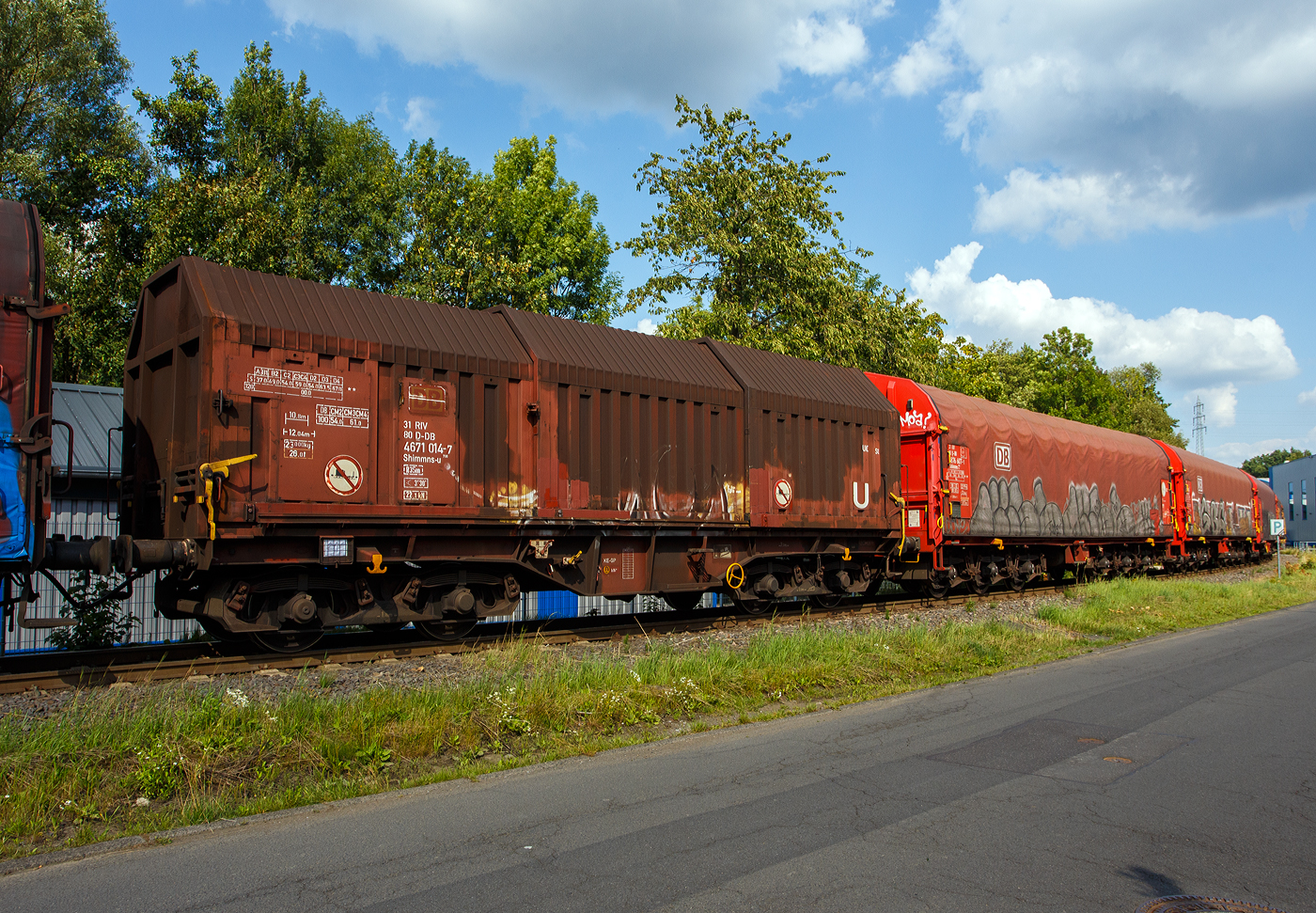 Vierachsiger Drehgestell-Flachwagen mit verschiebbaren Teleskophauben für Coiltransporte, 31 80 4671 014-7 D-DB, der Gattung Shimmns-u 708, der DB Cargo AG, am 25 Juli 2025 im Zugverband bei der Zugdurchfahrt in Neunkirchen-Struthütten auf der Talbahn (KSW-Strecke, Betriebsstätte FGE - Freien Grunder Eisenbahn) in Richtung Pfannenberg.

Der Wagen eignet sich speziell für den Transport witterungsempfindlicher Blechrollen. Er besitzt feste Stirnwände, 5 fest im Untergestell eingebaute Lademulden und drei teleskopartig angeordnete Hauben, die sich zu beiden Wagenenden hin soweit durch Ineinanderschieben öffnen lassen, dass jeweils 2/3 des Wagens freigelegt werden kann. Hierdurch ist eine einfache Beladung des Wagens sowohl von oben als auch von der Seite aus möglich. Der Wagen darf nur mit geschlossenen und verriegelten Hauben verkehren.

Das Untergestell und die festen Stirnwände, die als Abkantrahmenkonstruktion mit Blechbekleidung und hutförmigen Verstärkungsprofilen ausgeführt sind, sowie die fest auf den Außenlangträgern angeordneten drei Laufschienen je Wagenseite bilden den als Schweißkonstruktion ausgeführten Wagenkasten. Das Untergestell mit seinen beiden kräftigen Außenlangträgern besteht aus Walz- und Abkantprofilen. Die Untergestellenden bestehen aus den Hauptquerträgern, den AK-Trägern und den Kopfstücken. Die sattelförmig angeordneten, jeweils mit den Außenlangträgern verschweißten Querträger bilden zusammen mit 6 mm dicken Muldenblechen die Lademulden.

Die teleskopartig ineinander verschiebbaren Stahlhauben bestehen aus einer Hohlprofil-Rahmenkonstruktion und einer mit Sicken versehenen Beblechung. Die Abdichtung der Hauben untereinander und zu den Stirnwänden hin erfolgt über labyrinthartig ausgeführten Umrandungsprofilen. Die Endhauben verriegeln in geschlossener Stellung automatisch. Das Entriegeln der Hauben ist sowohl vom Erdboden wie auch von der Rampe möglich. Die beidseitig an jeder Stirnwand angeordneten Verriegelungseinrichtungen sind durch Wellen miteinander verbunden. Hierdurch ist das Entriegeln von nur einer Wagenseite aus möglich. Jede Haube läuft auf 4 jeweils und mit Abhebesicherungen versehenen Laufwagen mit nadelgelagerten Doppelrollen.

Die Wagen der Bauart Shimmns 708 sind mit 12 verstellbaren Festlegearmen ausgerüstet, die in fest auf den Muldenkappen angeordneten kammartig ausgeführten Halterungen gelagert sind. Die Festlegearme und ihre Anordnung ergeben einen wirksamen Schutz gegen unzulässiges seitliches Verschieben der Coils.

Um unzulässige Radlastabweichungen auszuschließen, ist eine möglichst mittige Verladung der Coils erforderlich. Ein durch alle Mulden in Wagenmitte verlaufender weißer Farbstreifen dient hierzu als Orientierungshilfe.

TECHNISCHE DATEN:
Spurweite: 1.435 mm (Normalspur)
Achsanzahl: 4 (in 2 Drehgestelle)
Länge über Puffer: 12.040 mm
Länge der Ladefläche: 10.800 mm
Ladebreite (Mulden): 2.400 mm
Drehzapfenabstand: 7.000 mm
Achsabstand im Drehgestell: 1.800 mm
Laufraddurchmesser: 920 mm (neu)
Eigengewicht: 23.000 kg
Höchstgeschwindigkeit: 100 km/h (beladen) / 120 km/h (leer)
Maximales Ladegewicht: 67,0 t (ab Streckenklasse D4) / 61,0 t bei DB ab CM3
Kleinster bef. Gleisbogenradius: 35 m
Bauart der Bremse: KE-GP (LL)
Bremssohle: IB 116
Handbremse: Ja
Intern. Verwendungsfähigkeit: RIV