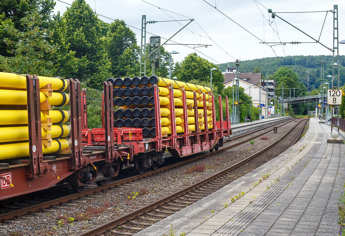 Vierachsiger Drehgestellflachwagen mit Rungen, Stirnwandklappen und Niederbindeeinrichtung, 81 80 4712 126-6 D-DB, der Gattung Sns 727, der DB Cargo AG am 20 Juni 2024 im Zugverband bei einer Zugdurchfahrt im Bahnhof Kirchen (Sieg). Hier beladen mit 36 gelb beschichteten Gasrohren bzw. HFI-längsnahtgeschweißte Stahlrohre Ø 323.9 x 12,7 (DN/NW 300 mm bzw. 12 ¾ Inch) mit gelber MAPEC® Polyethylen (HDPE)-Umhüllung), in Herstellungslänge vom 12 m. Das Metergewicht der Rohre beträgt 97,5 kg/m (ohne Umhüllung), so ist der Wagen mit ca. 45 t beladen. Der Hersteller der Stahlrohre ist die Salzgitter Mannesmann Line Pipe GmbH in Siegen (ex RW Fuchs).

In den Jahren 2001 und 2002 beschafft die DB AG vierachsige Flachwagen mit festen Rungenpaaren und niedrigen, umlegbaren Stirnborden, die mit je zwei kurzen Fallrungen gesichert werden. Die bei Grennbrier Europe Wagony Swidnica gebauten (dieser 2002) und als Sns 727 eingereihten Wagen, gleichen in vielen Komponenten den parallel beschafften Rbns 646, sind jedoch 5,91 m kürzer. Durch die reduzierte Länge und den kleineren Kurvenüberhang ließ sich die Wagenbreite um 330 mm gegenüber dem Rbns 646 vergrößern, und die Ladebreite von 2,52 m auf 2,85 m.

Wagenboden ist mit begehbaren (und nicht befahrbaren) Gitterrosten vollständig abgedeckt, die 15 hölzernen Ladeschwellen sind fest. An jeder Wagenseite befinden sich acht, innen mit Schichtholzleisten versehene Festrungenpaare (Doppelrungen), die im entlasteten Zustand oben 20 mm zur Fahrzeugmitte geneigt sind. Die in den Rungen integrierten Spannvorrichtungen verfügen über so lange Gurte, dass auch eine das G2-Profil ausnutzende Ladung gesichert werden kann. Der Sns 727 ist vorzugsweise für die Beförderung von Rohren, sowie den Transport von schweren Stahlerzeugnissen vorgesehen und überwiegend in festen Relationen im Einsatz.

TECHNISCHE DATEN:
Gattung: Sns 727
Spurweite: 1.435 mm (Normalspur)
Länge über Puffer: 20.440 mm
Drehzapfenabstand: 14.140 mm
Radsatzstand in den Drehgestellen: 1.800 mm
Ladelänge: 19.098 mm
Ladebreite: max. 2.850 mm (zwischen den Rungen)
Ladefläche: 54,4 m²
Fußbodenhöhe über SO: 1.350 mm (OK Ladeschwelle)
Rungenhöhe: 2.000 mm
Eigengewicht: ca. 26.360 kg
Zuladung bei Lastgrenze S: 63,5 t (ab Streckenklasse D); DB Netz CM 57,5 t
Max. Geschwindigkeit: 100 km/h / 120 km/h (leer)
Kleinster Gleisbogenhalbmesser: 75 m
Bauart der Bremse: KE-GP-A (LL)
Bremssohle: IB 116
Verwendungsfähigkeit: nein
