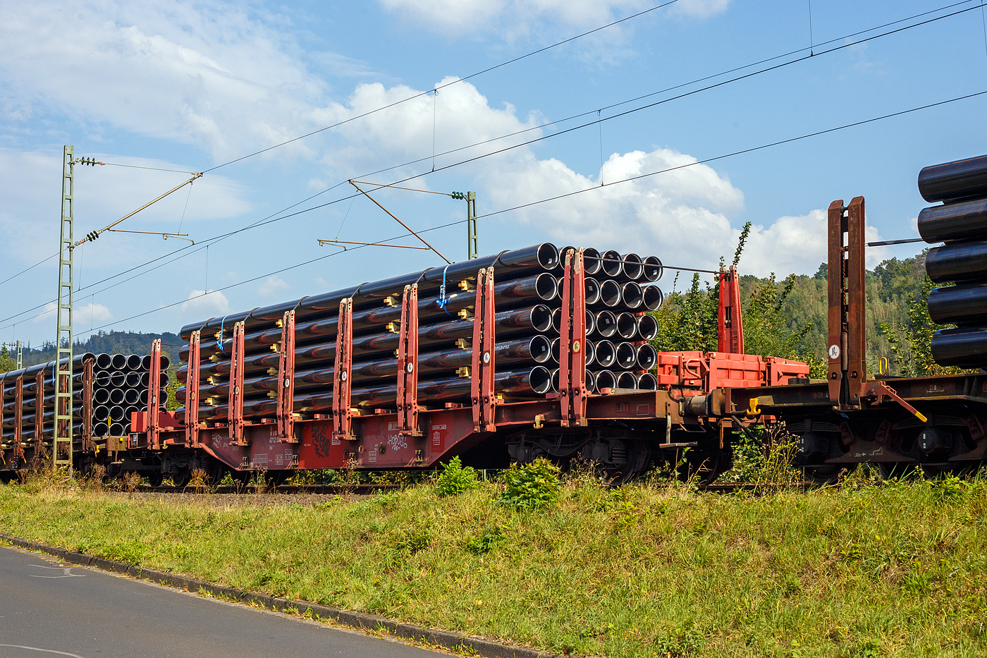 Vierachsiger Drehgestellflachwagen mit Rungen, Stirnwandklappen und Niederbindeeinrichtung, 81 80 4712 008-9 D-DB, der Gattung Sns 727, der DB Cargo AG am 19 September 2024 im Zugverband bei einer Zugdurchfahrt im Bahnhof Kirchen (Sieg). Hier beladen mit 30 HFI-längsnahtgeschweißte Stahlrohre Ø 323.9 (DN/NW 300 mm bzw. 12 ¾ Inch) in Herstellungslänge vom 12 m. Der Hersteller der Stahlrohre ist die Salzgitter Mannesmann Line Pipe GmbH in Siegen (ex RW Fuchs).

In den Jahren 2001 und 2002 beschafft die DB AG vierachsige Flachwagen mit festen Rungenpaaren und niedrigen, umlegbaren Stirnborden, die mit je zwei kurzen Fallrungen gesichert werden. Die bei Grennbrier Europe Wagony Swidnica gebauten und als Sns 727 eingereihten Wagen, gleichen in vielen Komponenten den parallel beschafften Rbns 646, sind jedoch 5,91 m kürzer. Durch die reduzierte Länge und den kleineren Kurvenüberhang ließ sich die Wagenbreite um 330 mm gegenüber dem Rbns 646 vergrößern, und die Ladebreite von 2,52 m auf 2,85 m.

Wagenboden ist mit begehbaren (und nicht befahrbaren) Gitterrosten vollständig abgedeckt, die 15 hölzernen Ladeschwellen sind fest. An jeder Wagenseite befinden sich acht, innen mit Schichtholzleisten versehene Festrungenpaare (Doppelrungen), die im entlasteten Zustand oben 20 mm zur Fahrzeugmitte geneigt sind. Die in den Rungen integrierten Spannvorrichtungen verfügen über so lange Gurte, dass auch eine das G2-Profil ausnutzende Ladung gesichert werden kann. Der Sns 727 ist vorzugsweise für die Beförderung von Rohren, sowie den Transport von schweren Stahlerzeugnissen vorgesehen und überwiegend in festen Relationen im Einsatz.

TECHNISCHE DATEN:
Gattung: Sns 727
Spurweite: 1.435 mm (Normalspur)
Länge über Puffer: 20.440 mm
Drehzapfenabstand: 14.140 mm
Radsatzstand in den Drehgestellen: 1.800 mm
Ladelänge: 19.098 mm
Ladebreite: max. 2.850 mm (zwischen den Rungen)
Ladefläche: 54,4 m²
Fußbodenhöhe über SO: 1.350 mm (OK Ladeschwelle)
Rungenhöhe: 2.000 mm
Eigengewicht: ca. 26.360 kg
Zuladung bei Lastgrenze S: 63,5 t (ab Streckenklasse D); DB Netz CM 57,5 t
Max. Geschwindigkeit: 100 km/h / 120 km/h (leer)
Kleinster Gleisbogenhalbmesser: 75 m
Bauart der Bremse: KE-GP-A (LL)
Bremssohle: IB 116
Verwendungsfähigkeit: nein