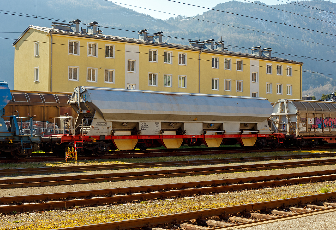 Vierachsiger gedeckter Drehgestell-Schüttgutwagen mit öffnungsfähigem Dach und dosierbarer Schwerkraftentladung, speziell für den Transport von Lebensmitteln, 31 81 0939 088-6 A-RCW der Gattung Tadnps, der Rail Cargo Austria (zur ÖBB), abgestellt am 03 April 2025 im Bahnhof Ebensee am Traunsee an der Salzkammergutbahn. Das Einsatzgebiet dieser Wagen (0939 001 – 098) ist Salz, was ja auch zu den Lebensmitteln gehört. Seine wirtschaftliche Existenz verdankt die Gemeinde Ebensee am Traunsee der Salzproduktion. In Ebensee ist die Salinen Austria AG ansässig. 

TECHNISCHE DATEN:
Spurweite: 1.435 mm (Normalspur)
Länge über Puffer: 21.640 mm
Drehzapfenabstand: 16.600 mm
Achsanzahl: 4
Achsabstand im Drehgestell: 1.800 mm
Laufraddurchmesser: 920 mm (neu)
Beladeöffnung: 16.800 x 1.200 mm
Eigengewicht: 26.560 kg
Höchstgeschwindigkeit: 100 km/h (beladen) / 120 km/h (leer)
Maximales Ladegewicht: 63,4 t ab Streckenklasse D
Kleinster bef. Gleisbogenradius: 75 m
Rauminhalt: 80,0 m³
Bremse: KE-GP-A (LL)
Intern. Verwendungsfähigkeit: RIV
Besonderheiten: Unterkante der festen Auslaufrutsche 400mm über SOK, 1.000 mm von Gleismitte, Breite 1.050 mm. Mittelentleerung deaktiviert, ein Rüttelmotor je Trichter.

Die Bedeutung der Gattungs- und Kennbuchstaben (hier Tadnps):
T - Wagen mit öffnungsfähigem Dach 
a - mit vier Radsätzen
d - mit Schwerkraftentladung, dosierbar, wahlweise zweiseitig, hochliegend
n - mit vier Radsätzen höchste Lastgrenze über 60 t
p - mit Schwerkraftentladung, dosierbar, mittig, hochliegend
s - Höchstgeschwindigkeit 100 km/h (beladen)