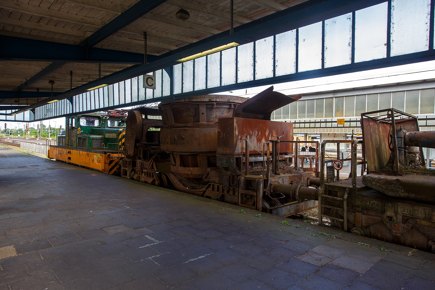 Vierachsiger Schlackenwagen Nr. 50 (Pfannenwagen zum Transport von flüssiger Schlacke) vom Hersteller BAMAG (Berlin-Anhaltische Maschinenbau Aktiengesellschaft) am 24 Juni 2025 beim Hauptbahnhof Oberhausen am Museumsbahnsteig/-gleis. Der Wagen wurde vermutlich auf der Henrichshütte in Hattingen (Ruhr) verwendet. 

Bereits an der massiven und schweren Bauweise sieht man den Fahrzeugen den Verwendungszweck Montanindustrie an. Solche Wagen sind in der Regel nur innerhalb der Stahlwerke im Einsatz, man sieht sie nicht auf den Gleisen der Staatsbahnen.

In Stahlwerken werden solche Wagen für den Transport von Schlacke verwendet. Vor allen bei der Roheisenerzeugung (Eisenverhüttung mittels Hochöfen) fällt sehr viel Schlacke an, aber auch bei der weiteren Stahlerzeugung/-verhüttung. Die flüssige und heiße Schlacke wird u.a. beim Abstich des Hochofens in die Pfanne des Wagens geleitet. Dann wird der Zug mit mehreren Schlackenwagen an die entsprechende Schlackengrube gefahren wo die noch flüssige ausgekippt wird. Nach dem erkalten wird dann die Schlacke mit Radladern o.ä. verlanden und auf die Schlackenhalde verbracht. Dies ist dann der typische Schlackensand oder auch Hüttensand genannt. Hier in der Region dem Siegerland waren viele Hochöfen in Betrieb, heute erinnern meist nur noch die Schlackenhalden daran. Unteranderem auch in Herdorf. 
