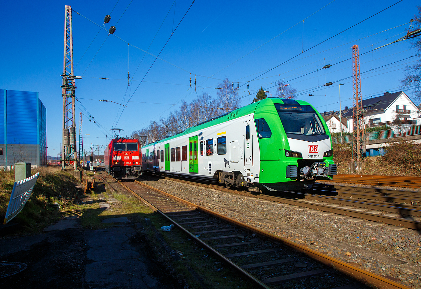 Während links auf dem Stumpfgleis die 185 359-7 der DB Cargo AG wartet, rauscht rechts der für die DB Regio AG – NRW fahrende dreiteilige Stadler FLIRT 3 XL 3427 015 (94 80 3427 015-7 D-STAP /  94 80 3827 015-3 D-STAP / 94 80 3427 515-6 D-STAP) der ZV VRR Eigenbetrieb Fahrzeuge und Infrastruktur, als RE 34 „Dortmund-Siegerland-Express“ (Dortmund - Letmathe - Siegen), von Kreuztal weiter in Richtung Siegen.

Der Stadler FLIRT 3 XL wurde 2020 von der Stadler Pankow GmbH in Berlin unter den Fabriknummern 42359 bis 42361 gebaut und an den Zweckverband Verkehrsverbund Rhein-Ruhr Eigenbetrieb Fahrzeuge und Infrastruktur geliefert. Eigentlich war dieser FLIRT 3 XL wie 9 weitere für die Bedienung der Regiobahnstrecke S 28 Kaarst - Neuss - Düsseldorf - Mettmann - Wuppertal vorgesehen, wo die Elektrifizierung bis 2020 erfolgen sollte. Da aufgrund von Verzögerungen der elektrische Betrieb voraussichtlich erst 2026 aufgenommen werden kann, wurden die inzwischen gelieferten Triebwagen u. a. von der DB Regio AG NRW eingesetzt.