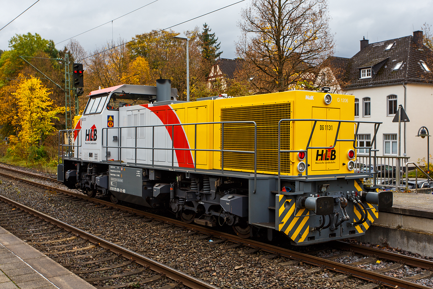 Welch seltener Gast auf der Siegstecke, auch wenn Triebzüge und -wagen der HLB hier Alltag sind, ist die Güterlok der HLB meist in und um Kassel unterwegs. Die Diesellokomotive 275 024-8, alias DG 1131 (92 80 1275 024-8 D-HEB), die Vossloh/MaK G 1206 der HLB - Hessische Landesbahn GmbH, hat am 16 Oktober 2025, auf den Weg in Richtung Köln, im Bahnhof Kirchen/Sieg Hp 0, da es eine Weichenstörung gab.

Die MaK G 1206 wurde 2001 von der VSFT - Vossloh Schienenfahrzeugtechnik GmbH in Kiel-Friedrichsort unter der Fabriknummer 1001131 gebaut und an die LC - Locomotion Capital Ltd. (London) als Mietlok geliefert. 

Lebenslauf/Stationen und Bezeichnungen:
•	Dezember 2001 - Vermietung an NE - Städtische Hafenbetriebe Neuss
•	Januar 2002 - Vermietung an StEK - Städtische Eisenbahn Krefeld 
•	Januar 2002 - Vermietung an Niederrheinische Verkehrsbetriebe AG (NIAG) 
•	Januar/Februar 2002 - Vermietung an OHE- Osthavelländische Eisenbahn AG 
•	Februar 2002 bis August 2003 - Vermietung an IL - InfraLeuna Infrastruktur- und Service GmbH, als IL 206
•	April 2003 - Verkauf an ATC - Angel Trains Cargo SA, Antwerpen (B)
•	August 2003 bis - Vermietung an RBH - RAG Bahn und Hafen GmbH als  RBH 841  
•	April bis Juni 2005 - Vermietung an MEG - Mitteldeutsche Eisenbahn GmbH  MEG 298  
•	November 2005 bis Oktober 2006 - Vermietung an MVG - Mülheimer Verkehrsgesellschaft mbH, Mülheim (Ruhr)  2  
•	November 2006 bis 2013 Vermietung an CFL - Société Nationale des Chemins de Fer Luxembourgeois bzw. CFL Cargo als 1504. Ab 2007 dann NVR-Nummer 92 82 0001 504-0 L-CFLCA. Zum 01.01.2010 aus der ATC wird die Alpha Trains Belgium NV/SA. 
•	Juni 2013 bis Dezember 2014 - Vermietung an HLB - Hessische Landesbahn GmbH  
•	31.12.2014 - Verkauf an die HLB - Hessische Landesbahn GmbH, Betreiber Bezeichnung  DG 1131 , vergabe der NVR-Nummer 92 80 1275 024-8 D-HEB. Auffällig ist das sie, trotz der längeren Einsatzdauer in Luxemburg, heute nur die UIC-Zulassung für Deutschland (D) hat. 

Die MaK G 1206 ist im schweren Rangier- und Streckendienst einsetzbar. Sie wurde 1997 zum ersten Mal gebaut und ist nach Deutschland, Österreich, der Schweiz, Luxemburg, Italien, Spanien, den Niederlanden und nach Frankreich verkauft worden. Allein 23 Lokomotiven fahren als BB 61000 bei der SNCF, davon sechs mit MTU-Motor (Die G 1206 gibt es wahlweise mit Caterpillar- oder MTU-Motor). Diese Lok hat einen Caterpillar 12 Zylinder 4-Takt Dieselmotor mit Abgasturbolader und Ladeluftkühlung vom Typ 3512B DI TA-SC mit einer Leistung von 1.500 kW bei1.800 U/min. Das Strömungsgetriebe ist ein Voith L 5r4 zU2.
