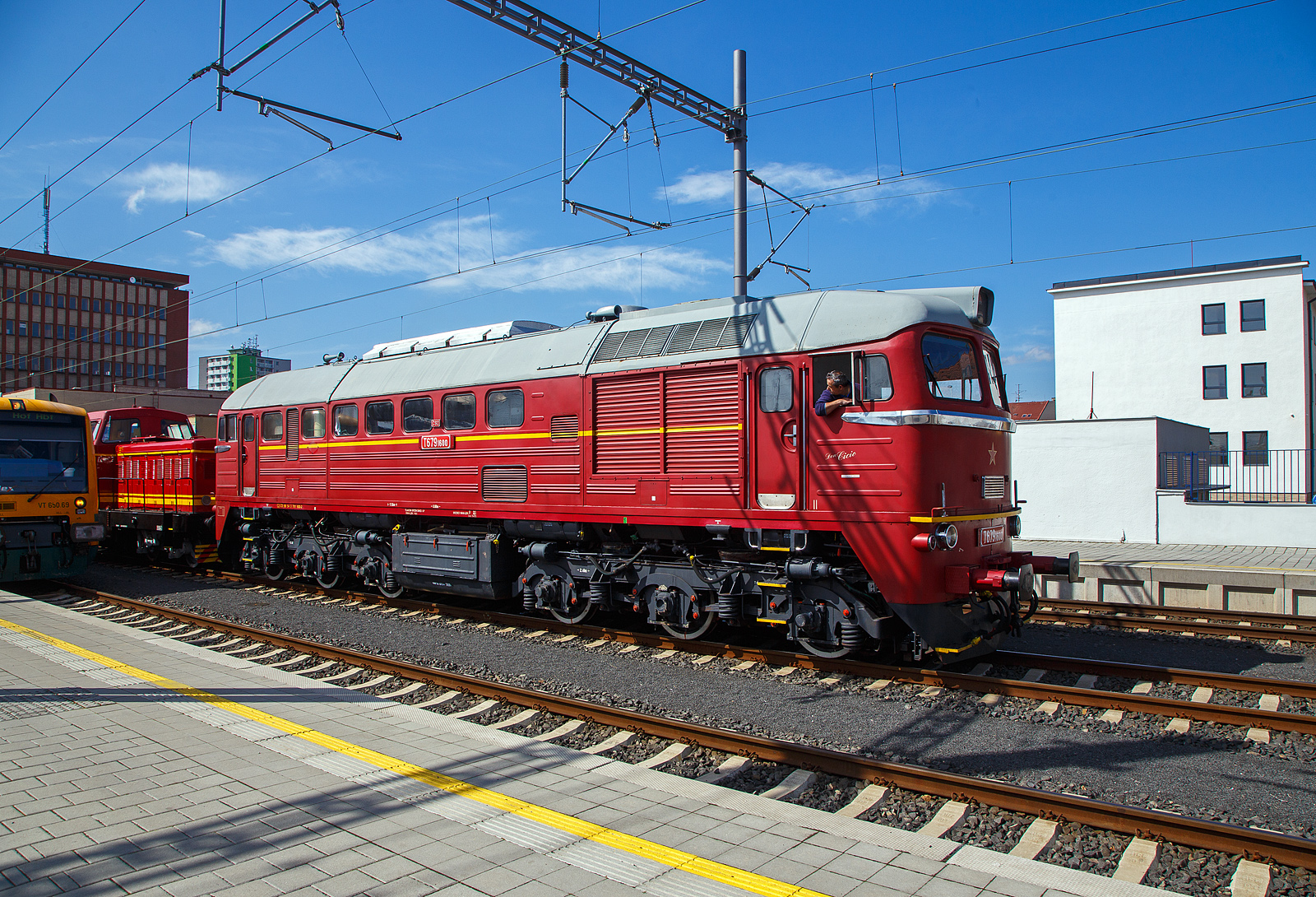 Wie in „alten Zeiten“ der ČSD in der Tschechoslowakei.....
Im Bahnhof Cheb (Eger) rangiert am 21.04.2023, die ex ČSD T679.1600 „Don Cicío“, heutige ČD 781 600-2 (CZ-ČD 90 54 3 781 600-2) mit dem Rotkäppchen („Karkulka“) T 444.030 (heute CZ- ČD 90 54 3 725 030-1) am Haken. 

Lokomotive der wurde 1979 von der Lokomotivfabrik Luhansk, deutsche Transliteration Luhanskyj Teplowosobudiwnyj Sawod (LTS), in der damaligenSowjetunion (heute Ukraine) unter der Fabriknummer 3426 gebaut. Die Herstellerbezeichnung ist LTS M62. Die für die DDR gebaute Variante (weitgehend baugleich mit dieser hier) der sowjetischen Bauart M62 sind in Deutschland bekannt als DR V 200 „Taigatrommel“, später DR 120, zuletzt DB 220.

Die ČSD-Baureihe T 679.1 (ab 1988 Baureihe 781) sind dieselelektrische Lokomotiven der ehemaligen Tschechoslowakischen Staatsbahn (ČSD) für den schweren Güterzugdienst. Wegen ihrer Herkunft erhielten die Lokomotiven den Beinamen Sergej. 

Die Lokomotiven wurden ab Mitte der 60er Jahre in der sowjetischen Lokomotivfabrik Woroschilowgrad (später Luhansk) für den Einsatz bei den Bahnverwaltungen des gesamten RGW entwickelt und produziert. Nachdem bereits die Ungarische Staatsbahn (MÁV) und die Polnischen Staatsbahnen (PKP) Lokomotiven dieses Typs beschafft hatten, entschied sich Mitte der 60er Jahre auch die ČSD für solche Lokomotiven.

1966 wurden die ersten 50 Lokomotiven an die ČSD geliefert. Bis 1979 beschaffte die ČSD insgesamt 599 Lokomotiven dieser Baureihe. 25 Lokomotiven der ersten Serie wurden breitspurig als T 679.5 für die grenzüberschreitende Strecke Bahnstrecke Uschhorod–Haniska (Sowjetunion, heute Ukraine) in Dienst gestellt. Nach der Elektrifizierung ihrer Stammstrecke in den Jahren 1973 bis 1978 wurden sie dort nicht mehr benötigt. Ein Teil dieser Lokomotiven wurde darum auf Regelspur umgespurt. Acht Lokomotiven blieben jedoch für die Bedienung der Werksanschlüsse breitspurig und erhielten ab 1988 die neue Baureihenbezeichnung 781.8. Die breitspurigen Lokomotiven wurden 1991 ausgemustert und verschrottet. 

Bereits 1987 verringerte sich der Lokomotivbestand erstmals, als neun Lokomotiven an die Ungarische Staatsbahn MÁV verkauft wurden. Nach 1990 wurden die Lokomotiven durch den zurückgehenden Güterverkehr und die fortschreitende Elektrifizierung der wichtigsten Hauptstrecken zunehmend überflüssig. 1997 endete der Einsatz der Sergejs in der Slowakei. In Tschechien waren die Lokomotiven für den schweren Güterverkehr auf der sogenannten „Podkrušnohorska magistrála“ (Strecke Chomutov–Cheb) vorerst unverzichtbar. Letztes Einsatzgebiet der Lokomotiven in Tschechien waren die schweren Kohleganzzüge von Sokolov zum Kraftwerk Arzberg in Oberfranken. Diese Verkehre endeten am 30. November 2002 mit der Stilllegung des Kraftwerkes.

Konstruktion und Technik:
Die M62 ist als schwere sechsachsige Güterzuglokomotive konstruiert. Der Rahmen ist als selbsttragender Brückenrahmen aus zwei inneren Hauptlängsträgern aus Doppel-T-Trägern und zwei äußeren Längsträgern aus U-Profilen aufgebaut, die durch Deckbleche und die Zugkästen an den Frontseiten verbunden sind. Der Lokkasten ist aus gekanteten Profilen und gesickten Blechen geschweißt. Der Rahmen der dreiachsigen Drehgestelle besteht aus zwei äußeren Längs- und zwei inneren Querträgern und dem darüber angeordneten Drehzapfenträger. Der hierauf mit dem Drehzapfenlager aufgesetzte Lokkasten ist mit einer Abstützrückstelleinrichtung abgestützt.

Herzstück dieser Lok ist der Dieselmotor, ein wassergekühlter V 12 Zylinder- Zweitakt- mit zwei Abgasturboladern und Rootsgebläse mit einem Hubraum von 149,6 Litern  vom Typ Kolomna 14 D 40. Die mechanische Leistung beträgt 1.470 kW (1.998 PS) bei einer Drehzahl von 750 U/min. Die Leistung wurde durch einen fremderregten Gleichstromgenerator für die Fahrmotoren in Gleichstrom umgewandelt. Die Leistungsregelung erfolgte durch einen magnetischen Flussregler im Erregerfeld der Erregermaschine. Die Fahrmotoren sind Reihenschlussmotoren. Deren Traktionsleistung betrug zusammen 1,270 kW (1727 PS). Um Ankerströme und Drehmoment der Fahrmotoren im oberen Geschwindigkeitsbereich wieder anzuheben, besaß die Lok zwei Shuntierungsstufen, die parallel zu den Erregerwicklungen der sechs Tatzlager-Fahrmotoren geschaltet wurden. Eine ähnliche Konstruktion verwendet die Lokfamilie der DR-Baureihe 130. Entsprechend der Auslegung als Güterzuglokomotive besitzt die M62 keine Zugheizeinrichtung. Einsätze im Reisezugdienst waren daher auf wärmere Jahreszeiten beschränkt oder erforderten den Einsatz von Heizwagen bzw. von Wagen mit Eigenheizung.

Ein besonderes Bauteil ist das Rootsgebläse, es fördert Verbrennungsluft und erzeugt eine Vorverdichtung von 0,2 bar. Das ist notwendig, weil ein Zweitakt-Motor durchgespült werden muss, er kann mit gleichzeitig offenen Einlassschlitzen und Auslassventilen nicht selbsttätig ansaugen. Nach dem Start laufen die beiden Turbolader hoch und steigern den Ladeluftdruck auf rund 1,2 bar. Der Dieselmotor hat eine Leerlaufdrehzahl von 400 U/min, aber schon bei 750 U/min seine Höchstdrehzahl. Der Motor besitzt Zylinder in V-Anordnung mit je 12,46 Litern Hubraum. Dabei sitzen die Kolben der B-Seite mit Anlenkpleueln auf den Hauptpleueln der A-Seite. Damit ändern sich die Kolbengeschwindigkeiten zwischen A- und B-Seite. Der Motor erzeugt auf beiden Zylinderbänken unterschiedlich viel Leistung. Der Kraftstoffvorrat beträgt 3.900 Liter Dieselöl.

Die Lüfter für Fahrmotoren und Traktionsgenerator sind mechanisch über Gelenkwellen vom Dieselmotor angetrieben. Der Kühlerlüfter wurde auch direkt vom Dieselmotor angetrieben, zur Steuerung ist eine Strömungskupplung dazwischengeschaltet.

Charakteristisches Merkmal der ersten Lieferserien der M62, die noch ohne Schalldämpfer geliefert wurde, war das laute Auspuffgeräusch, das ihnen in der DDR zum Spitznamen „Taigatrommel“ verhalf.  In Deutschland, Tschechien und der Slowakei sind die M62 aus dem Dienst der Staatsbahnen ausgeschieden, in allen anderen Ländern sind sie noch im Einsatz. 

TECHNISCHE DATEN:
Gebaute Anzahl: 574  Stück T 679.1 und 25 Stück T 679.5 (Breitspur)
Hersteller:  Lokomotivfabrik Lugansk
Baujahre: 1966 bis 1979
Achsformel: Co’Co’
Spurweite:  1.435 mm (1.520 mm bei T 679.5)
Länge über Puffer: 17.550 mm
Höhe: 4.493 mm
Breite: 2.950 mm
Drehzapfenabstand: 8.600 mm
Achsabstand im Drehgestell: 4.200 mm (2 x 2.100 mm)
Treibraddurchmesser:  1.050 mm
Kleinster bef. Halbmesser: 125 m
Dienstgewicht: 116 t 
Höchstgeschwindigkeit: 100 km/h
Installierte Leistung: 1.471 kW (1.998 PS)
Traktionsleistung (Leistung am Rad): 1.271 kW (1.727 PS)
Anfahrzugkraft: 260 kN
Dauerzugkraft: 200 kN
Motorentyp: Kolomna 14 D 40
Motorbauart: Zweitakt-Zwölfzylinder-V-Motor
Nenndrehzahl: 750 U/min (Leerlauf 400 U/min)
Leistungsübertragung: elektrisch
Anzahl der Fahrmotoren: 6 vom Typ ED 107
Tankinhalt: 3.900 l
Bremse: ŠKODA N-O, Dako-BS-2

Quellen: Wikipedia, atlaslokomotiv.net